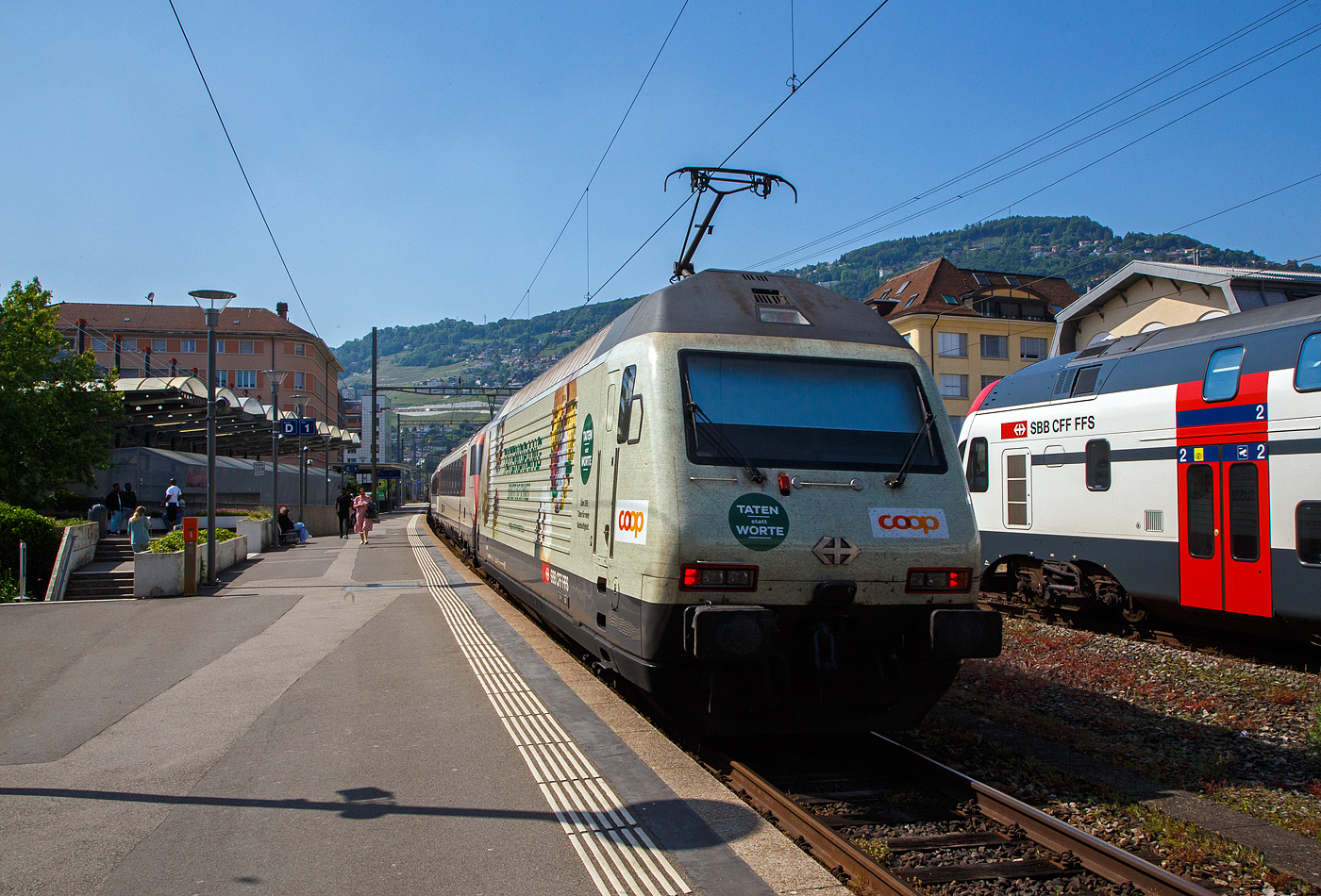 Der IR 90 von Brig nach Genève-Aéroport (Umlauf IR 1724) verlässt am 26 Mai 2023 den Bahnhof Vevey und fährt weiter in Richtung Lausanne bzw. Genf. Da der Zug recht lang war wurde im Sandwich gefahren, geführt von der SBB Re 460 069-8  Verkehrshaus  und hier im Bild am Zugschluss von der Werbe-LOK2000, der SBB Re 460 041-7  Mendrisiotto  (91 85 4 460 041-7 CH-SBB) mit der COOP Werbung.

Die Re 460 041-7 wurde 1993 von der SLM (Schweizerischen Lokomotiv- und Maschinenfabrik in Winterthur) unter der Fabriknummer 5518 gebaut, der elektrische Teil ist von der ABB (Asea Brown Boveri). Im SBB Werk Yverdon-les-Bains erfolgte 2018 die vollständige Modernisierung LOK2000, so soll sie fit für die nächsten 20 Jahre sein.

Seit 2021 trägt die Re 460 041-7 die COOP-Werbung mit der Aufschrift:
TATENDRANG 
BEWEGT DIE SCHWEIZ
TATEN statt WORTE - Über 395 Taten für mehr Nachhaltigkeit.

Modernisierungs-/Refit-Programm der LOK2000 (Re 460):
Zwischen 2015 und November 2022 unterzog die SBB alle ihrer 119 Re 460 Lokomotiven (LOK2000) einem Refit-Programm (Modernisierung) im SBB Werk Yverdon-les-Bains (VD). Dabei wurden unter anderem die auf dem GTO-(Thyristor)-Halbleiter-Technologiestand der 1990er-Jahre basierende Leistungselektronik (GTO- Traktionsumrichter) durch IGBT-Traktionsumrichter (insulated-gate bipolar transistor) der neuesten Generation von ABB ersetzt, welche die Fahrmotoren mit Strom speisen und Bremsenergie zurückgewinnen. Die SBB hat damit, in Zusammenarbeit mit der ABB, die gesamte Flotte Re 460 modernisiert und hat diese auf den neuesten Stand der Antriebstechnik gebracht. Die gesamte Flotte spart dank neuen Traktionsumrichtern und weiteren technischen Optimierungen jedes Jahr rund 30 Gigawattstunden Energie ein, das sind fünf Gigawattstunden mehr als ursprünglich erwartet. Die Energieeinsparungen entsprechen dem durchschnittlichen Stromverbrauch von 10.000 Schweizer Haushalten. Die Umrüstung auf modernste IGBT-Technologie und mit Wasser statt Öl betriebene Kühlsysteme der Umrichter ermöglicht eine Senkung des Energieverbrauchs und sorgt für einen ökologischeren und sicheren Bahnbetrieb.

Geschichte und Beschreibung:
Die SBB bestellte im Zusammenhang mit den Projekten Bahn 2000 eine erste Serie von 12 Universal-Hochgeschwindigkeitslokomotiven, noch als Re 4/4VI – 10701 bis 10712 bestellt. Diese Bestellung wurde noch vor Beginn der Konstruktionsarbeiten auf 24 erhöht. Für den alpenquerenden Güterverkehr wurde von der Eidgenossenschaft eine weitere Serie von 75 Lokomotiven (auch als 'Hupac'-Lokomotiven bekannt) in Auftrag gegeben. Die vorgegebenen Liefertermine für dieses Los waren derart kurz, dass die SLM an die Kapazitätsgrenze ihrer Werkstätte gelangte. Es wurden deshalb dreißig Lokkasten an Krauss-Maffei in München untervergeben 

Im Hinblick auf die geplante Hochgeschwindigkeitsstrecke wurden nochmals zwanzig Lokomotiven nachbestellt, was die Serie auf 119 ansteigen ließ. Die im Volksmund Lok 2000 genannte Lokomotive hat eine Höchstgeschwindigkeit von 230 km/h und eine Leistung von 6,1 MW und ist für den Schnellzugs- wie Güterverkehr ausgelegt. Um die Gesamtmasse von 84 Tonnen nicht zu überschreiten musste ein gesickter Leichtbaukasten konstruiert werden, dessen Form vom Designstudio Pininfarina entworfen wurde.

Um auf den Strecken durch die Alpen den Radverschleiß gering zu halten, haben die Lokomotive radial einstellbare Achsen erhalten. Auch auf dem Gebiet der elektrischen Ausrüstung wurde Neuland beschritten. Zwei Ebenen Steuerelektronik für das Fahrzeug und den Antrieb sind eingebaut. Über das Fahrzeugleitgerät wurden zu viele Elemente gesteuert, wie Scheibenwischer oder Signalhorn. Dies führte anfänglich zu vielen Störungen und oft blieben Lokomotiven auf der Strecke liegen. Erst die Verbesserung der Programmierung erlaubte es die Zuverlässigkeit so zu erhöhen, dass es kaum mehr zu Ausfällen führte. Als Feststellbremse wurden in den Drehgestellen Permanentmagnetschienenbremsen eingebaut. Auch hier gab es am Anfang übermäßig viele Störungen und die Lokomotiven klebten regelmäßig an den Schienen fest.

Um den Schiebedienst auf den Gebirgsstrecken weniger personalaufwendig durchzuführen, wurden mehrere Lokomotiven mit einer amerikanischen Funkfernsteuerung ausgerüstet und als Ref 460 bezeichnet. Damit konnte von der Zugspitze aus eine am Zugschluss eingesetzte Lokomotive ferngesteuert werden. Die Divisionalisierung der SBB erlaubte es nicht mehr groß davon zu profitieren, denn alle Lokomotiven wurden dem Personenverkehr zugeteilt und der Einsatz vor Güterzügen war somit beendet.

Die Re 460 blieb nicht ein Einzelstück und entwickelte sich zu einer Lokomotivfamilie. Eine erste Bestellung wurde von der BLS für acht Lokomotiven gemacht. Die BLS Re 465 hat im Gegensatz zur Re 460 vier statt zwei Stromrichter. Jeder Motor hat dadurch seine eigene Regelung um die Eigenschaften im Bergeinsatz zu verbessern. Weiter können die BLS-Lokomotiven mit allen gängigen Schweizer Lokomotiven in Vielfachsteuerung verkehren. Das erlaubte es bei der BLS den Lokomotiveinsatz flexibler zu gestalten. Die SBB bestellte ebenfalls zehn Re 465, die bei Ablieferung schon das blaue BLS-Design hatten, aber erst später von der BLS übernommen wurden. Nach Finnland konnten auch in zwei Serien Lok 2000 verkauft werden. Dort sind sie als Sr2 bezeichnet. Nach Versuchsfahrten in Norwegen im schwierigen Winterdienst bestellten die NSB die fast baugleichen Lokomotive EL18 2241 bis 2262. Eine letzte Lieferung umfasst zwei Lokomotiven für Hongkong. Sie werden an jedem Ende eines Doppelstockzuges eingesetzt. Dies sind die letzten von SLM in Winterthur gebauten Fahrzeuge. Die Re 460 ist bis auf weiteres die letzte Vollbahn-Streckenlokomotive, die komplett von schweizerischen Unternehmen konstruiert und gebaut wurde. Der Lokomotivbau in der Schweiz wurde inzwischen aus wirtschaftlichen Gründen eingestellt. Einzig Stadler Rail stellt in der Schweiz noch Lokomotiven für den Rangier- und für den Zahnradbetrieb her.

TECHNISCHE DATEN der Re 460:
Nummerierung: 	Re 460 000–118
Anzahl: 119
Baujahre: 1991–1996
Hersteller: SLM - Winterthur / ABB (Asea Brown Boveri)
Design: Pininfarina
Hersteller Lokkasten: teilweise (30 Stück) Krauss-Maffei (München)
Spurweite: 1.435 mm (Normalspur)
Achsformel: Bo'Bo'
Länge über Puffer: 18.500 mm
Höhe: 4.300 mm
Breite: 3.000 mm
Drehzapfenabstand: 11.000 mm
Achsabstand im Drehgestell:  2.800 mm
Laufraddurchmesser: 1.110 mm (neu)
Dienstgewicht: 84,0 t
Höchstgeschwindigkeit:  200 km/h (zugelassen)  / 230 km/h (Techn. möglich) 
Stundenleistung: 6.100 kW / 8.300 PS
Dauerleistung: 4.800 kW / 6.000 PS
Anfahrzugkraft: 300 kN
Dauerzugkraft: 275kN
Stromsystem: 15 kV, 16,7 Hz (über Oberleitung)
