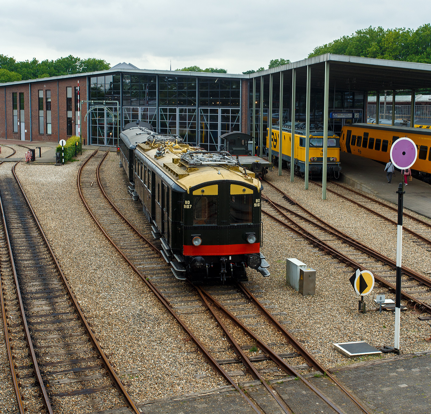 Der NS Mat ’24-Triebwagenzug (BD 9107, C 8553 und C 8104) „Blokkendozen“ (Kastendose) am 24 Juni 2025 im Het Spoorwegmuseum (bis 2005 NSM - Nederlands Spoorwegmuseum / Niederländischen Eisenbahnmuseum) in Utrecht im ehemaligen Bahnhof Maliebaanstation. Ein Eisenbahnmuseum das zum Verweilen einlädt. Hier im Vordergrund der Steuerwagen NS C 8104 (Ces) mit 88 Sitzplätzen der 3. Klasse und Durchgangsmöglichkeit, ex Triebwagen NS C 9411 (mCv).

Die NS-Baureihe Mat ’24 oder Materieel ’24 war eine (die erste) Serie von Elektrotriebzügen, die von der NS - Nederlandse Spoorwegen (Niederländischen Staatsbahnen, heute Niederländische Eisenbahnen AG) ab 1924 in großer Zahl eingesetzt wurde. Diese Züge sind unglaublich robust und schwer. nd der Tatsache, dass die Trainer wie Bausteine zusammengestellt werden können. Im Volksmund erhielten sie wegen des eckigen Äußeren und der Tatsache, dass die Wagen wie Bausteine zusammengestellt werden konnten, den Spitznamen „Blokkendozen“ (Kastendose). Ein weiterer Spitzname war „buffermaterieel“, weil sie im Unterschied zu anderen, mehr windschlüpfig aussehenden elektrischen Triebzügen mit üblicher Schraubenkupplung versehen waren. Wegen der Verbindung über Schraubenkupplung mit zwei Puffern konnten die Einheiten sehr flexibel kombiniert werden. Meist bestand ein Zug aus zwei Triebwagen und zwei oder drei antriebslosen Mittelwagen. Die lauten Geräusche der Motoren und Antriebe erinnerten manche Fahrgäste an Staubsauger, so dass auch dieser weitere Spitzname  Staubsauger  verwendet wurde. 

Ab Mitte der 1950er Jahre wurden die Mat ’24 zunehmend durch die neue Baureihe Mat ’54 ersetzt. Bei einigen Triebwagen wurden die Stromabnehmer und Motoren demontiert, sie wurden als einfache Beiwagen weiterverwendet. Da die Mat ’24 sehr robust waren, wurden einige Einheiten später auch als Postwagen oder für Dienstzwecke eingesetzt. Mehrere Wagen blieben museal erhalten.

Der Steuerwagen C 8104:
Der Steuerwagen C 8104 (Ces) wurde ursprünglich als Elektrotriebwagen C 9411 (mCv) 1928 bei NV Werkspoor in Zuilen mit einer elektrischen Installation von Heemaf in Hengelo gebaut. Er verfügte über 88 Sitzplätze der 3. Klasse und war als Spitzenverstärkung für die Hauptstrecke Amsterdam – Rotterdam vorgesehen. Durch einen Brand schwer beschädigt, wurde er 1944 zur Reparatur an Werkspoor gegeben, das inzwischen Teil der Gemeinde Utrecht geworden war. Erst nach dem Krieg im Jahr 1946 wurde C 9411 wieder in Dienst gestellt.

Der C 9411 war 1956 der erste Mat ’24-Triebwagen (Blokkendozen- Motorwagen) der in einen gezogenen Personenwagen, für den Einsatz hinter Elektrolokomotiven, umgebaut wurde und hauptsächlich als Spitzenverstärkung auf längeren Strecken innerhalb der Niederlande dienen sollte. Es erhielt daraufhin die Nummer B 5841 (Bz), wobei die 88 Sitzplätze auf Holzbänken unverändert blieben. Eine Einschränkung des Einsatzes war das Fehlen einer Toilette.

Aufgrund der Verfügbarkeit neuer und besserer Ausrüstung wurde der nunmehrige B 5841 im Jahr 1973 überflüssig. Anschließend wurde er zum Ausstellungswagen 99-31 003 umgebaut. Als solcher wurde er bis 1982 verwendet und dann für Museumszwecke reserviert.

Im Jahr 1983 begann man mit einer behutsamen Restaurierung, bei der zunächst die Innenausstattung mit Bänken und Türen eines zuvor abgerissenen „Blokkendozen“-Wagens (Kastendose-Wagens) wiederhergestellt wurde. Er erhielt erneut 88 Sitzplätze auf Holzbänken. Auch der voll ausgestattete Steuerstand wurde umgebaut. In den Jahren 1987 – 1989 erfolgte eine Generalüberholung und erhielt nun die Nummer C 8104 (Ces), da er nun mit den ursprünglichen Steuerwagen C 8101 – 8103 (Ces) identisch war. Der einzige Unterschied zwischen mCv und Ces besteht im Fehlen von Fahrmotoren und der dazugehörigen Elektroinstallation beim Ces.

Abkürzungen:
C = 3. Klasse
e = elektrischer Zwischenwagen
m = Triebwagen
s = ausgestattet mit Steuerstand
v = ausgestattet mit Steuerstand mit Balgdurchgang
z = ohne Toilette

Der dreiteilige Zug von Mat’24 des Niederländischen Eisenbahnmuseums, bestehend aus BD 9107, C 8553 und C 8104, war aufgrund einer Überholung des C 8104 und dem Fehlen der seit dem 1. April 2009 vorgeschriebenen automatischen Zugbeeinflussung ATB vorübergehend außer Betrieb. Die Überholung der Drehgestelle des C 8104 fand 2009 statt. Der Einbau der vereinfachten Version der ATB (ATBe) und deren Abnahme erfolgten im Mai und Juni 2010 bei Strukton in Zutphen. Im September wurde die Einsatzbescheinigung ausgestellt, danach fand am 9. Oktober wieder die erste Fahrt für ehrenamtliche Helfer des Eisenbahnmuseums statt.

Aufgrund größerer Wartungsarbeiten ist der Kastendosenzug aber z.Z. vorübergehend außer Betrieb.

TECHNISCHE DATEN:
Hersteller:	Werkspoor NV, Zuilen
Baujahr:1928
Typ:	Mat'24 ursprünglich '28 mC / seit 1989 Ces, Serie C 8101 – 8103 (8104)
Historischen Nummer:	ab 1928 - C 9411 / ab 1956 - B 5841 / ab 1973 - 99-31 003 / seit 1989 - C 8104
Spurweite:	1.435 mm (Normalspur)
Achsfolge:	2'2' (4 Achsen in zwei Drehgestellen)
Gewicht: 39 t
Länge über die Puffer:	19.800 mm
Höchstgeschwindigkeit: 120 km/h
Kupplung: Schraubenkupplung (UIC-Kupplung)
Betriebsfähigkeit: ja
