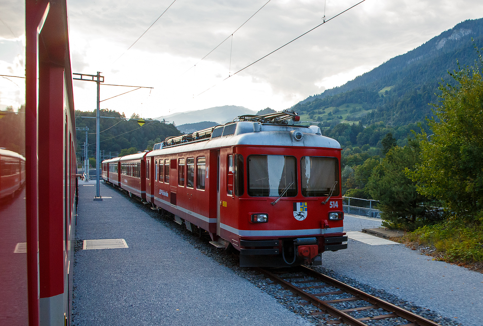 Der RhB Be 4/4 514 am 17.02.2017, mit einem Pendelzug, beim Bahnhof Reichenau-Tamins (aufgenommen aus dem Zug heraus).

Sechs dieser Elektrotriebwagen der Serie Be 4/4 mit den Betriebsnummern 511 bis 516 kommen bei der Rh�tischen Bahn (RhB) im Regionalverkehr, meist als dreiteilige Pendelz�ge (Triebwagen, Zwischenwagen B 24xx und Steuerwagen ABDt 17xx), zum Einsatz. 

Im Jahr 1971 lieferten die Unternehmen FFA (Wagenk�sten), SIG (Drehgestelle) und SAAS (elektrische Ausr�stung) die ersten vier Triebwagen (Nummern 511–14) an die RhB, seinerzeit die ersten serienm��igen Triebfahrzeuge der Schweiz mit stufenloser elektronischer Leistungsregelung (Phasenanschnittsteuerung mittels Thyristoren). Gleichzeitig stellte die RhB die dazu passenden Zwischenwagen B 2411–14 und Steuerwagen ABDt 1711–14 in Dienst, so dass vier dreiteilige Pendelz�ge gebildet werden konnten. Im Gegensatz zum �brigen RhB-Rollmaterial besitzen die Be 4/4-Pendelz�ge automatische Kupplungen und Druckluftbremsen; ein gemischter Einsatz mit anderen Fahrzeugen ist deshalb nicht m�glich. 1979 beschaffte die RhB zwei weitere praktisch baugleiche Z�ge mit den Endnummern 15 und 16. Nachdem 1988 vier zus�tzliche Zwischenwagen (B 2417–20) hinzugekommen waren, konnten auch vierteilige Z�ge verkehren. Ab 1994 durchliefen die Fahrzeuge ein umfangreiches Refit-Programm, wobei die elektrische Ausr�stung mit Ausnahme der Fahrmotoren komplett erneuert wurde.

Die gesamte Zugskomposition war von Anfang an darauf ausgelegt, einm�nnig bedient zu werden. Deshalb sind alle T�ren mit einer pneumatischen T�rschlie�ung ausgestattet, die vom F�hrerstand aus bet�tigt werden kann (seitenselektive T�rfreigabe). Die T�ren besitzen Druckknopf-Vorauswahltasten neben den T�ren. Auch besitzen sie eine T�rschlie�automatik, die beim Anfahren die T�ren selbstt�tig schlie�t und w�hrend der Fahrt geschlossen h�lt. Bei der Inneneinrichtung wurde auch darauf geachtet, dass gen�gend Haltestangen vorhanden sind, da im geplanten Einsatz durchaus mit Stehpassagieren gerechnet werden musste. Alle Achsen sind scheibengebremst. Die Drehgestelle sind mit Seitenanlenkern versehen und besitzen keine Drehzapfen. Der Triebwagen besitzt zwei zweiachsige Drehgestelle mit Einzelachsantrieb, die Achsformel lautet dementsprechend Bo’Bo’. Die Triebmotoren sind gegenl�ufig, mit entsprechend angepassten Getrieben, angeordnet. Diese – zwar aufwendigere – Anordnung hat Vorteile in der Laufruhe des Drehgestells. Die eingebaute Vielfachsteuerung ist f�r den Betrieb von bis zu drei Einheiten ausgelegt. Um ein schnelles Kuppeln und Entkuppeln zu gew�hrleisten, wurden automatische +GF+-Kupplungen in der Ausf�hrung f�r Vorortsbahnen (GFV) eingebaut, bei denen neben der mechanischen Verbindung zugleich auch die elektrischen und pneumatischen Leitungen gekuppelt werden.

Die Fahrzeuge verf�gen �ber eine Beschleunigung von 0,8 m/s�. Die zul�ssige Endgeschwindigkeit betr�gt 90 km/h. Die elektrische Bremse kann ebenfalls mit einer Verz�gerung von 0,8 m/s� den Zug bis auf eine Geschwindigkeit von 20 km/h abbremsen. Darunter schaltet sich die elektropneumatische Bremse selbstt�tig zu, um die abfallende Bremsleistung der elektrischen Bremse zu kompensieren. Die elektrische Bremse ist auch auf die Dauerbelastung ausgelegt, die bei einer Anwendung als Beharrungsbremse bei einem vollausgelasteten Zug in einem 45 ‰ Gef�lle auftritt (z.B. Davos – K�blis). Die Stundenleistung betr�gt 780 kW bei 45 km/h.

TECHNISCHE DATEN der Be 4/4:
Anzahl: 6 
Hersteller: FFA, SIG, SAAS
Baujahre: 1971 und 1979
Spurweite: 1.000 mm (Meterspur)
Achsformel: Bo’Bo’
L�nge �ber Puffer:  18,7 m (dreiteiliger Pendelzug 55,8 m)
Dienstgewicht: 44,6 t
Radsatzfahrmasse:  11,2 t
H�chstgeschwindigkeit:  90 km/h
Stundenleistung: 4 � 196 kW = 784 kW  (1.156 PS)
Beschleunigung:  0,8 m/s�
Bremsverz�gerung: 0,8 m/s�
Stromsystem:  11 kV 16,7 Hz
Anzahl der Fahrmotoren:  4
Bremse:  elektrische Widerstandsbremse
Zugbremse: elektropneumatische Druckluftbremse Bauart Oerlikon
Kupplungstyp:  +GF+-Vorortsbahnkupplung (GFV)