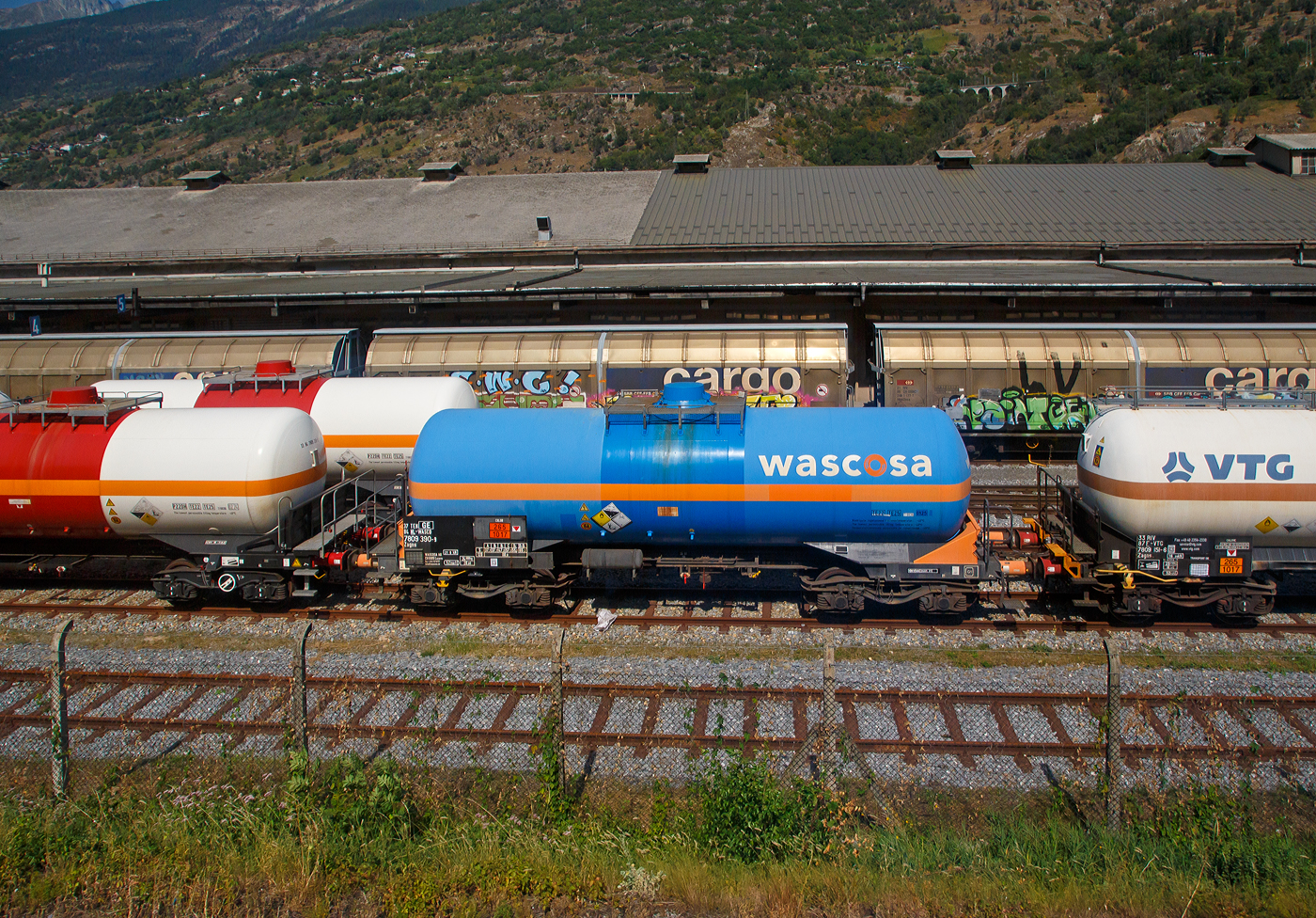 Der vierachsige Drehgestell-Druckgaskesselwagen (Flüssiggas-Kesselwagen für Chlor / Schwefeldioxid), 37 84 7809 390-9 NL-WASCO, der Gattung Zagns, der WASCOSA AG, laut Anschrift und Gefahrguttafel (265/1017) beladen mit Chlor, am 08 September 2021 abgestellt auf dem Werksgleisen des schweizerischen Chemie- und Pharmaunternehmens Lonza AG in Visp, aufgenommen aus einem Zug heraus. Oben im Hintergrund kann man gut die BLS Lötschberg-Bergstrecke erkennen,

TECHNISCHE DATEN:
Gattung: Zagns
Spurweite: 1.435 mm
Länge über Puffer : 13.455 mm
Drehzapfenabstand: 8.415 mm
Achsabstand im Drehgestell: 1.800 mm
Laufraddurchmesser: 920 mm (neu) / Radsätze BA 004 
Drehgestelle Typ:  Y25 Ls1
Höchstgeschwindigkeit: 100 km/h (beladen) / 120 km/h (leer)
Eigengewicht: 24.800 kg
Nutzlast: 65,2 ab Streckenklasse D  
Gesamtvolumen: 52.268 Liter
Behälterwerkstoff : Feinkornbaustahl (P460NL1)
Tankcode: P22DH
Sicherheitseinrichtungen: Crashpuffer, Entgleisungsdetektor, Aufkletterschutz
Kleinster befahrbarer Gleisbogen: R 35 m
Bremse: Knorr KG-GP-A (LL)
Bremssohlen: Jurid 816 M
Handbremse: Ja (20t), auf Bremserbühne
Intern. Verwendungsfähigkeit: TEN-GE

Die Bedeutung vom Tankcode:
P  = Tank für verflüssigte oder unter Druck gelöste Gase
22 = zutreffender Mindestprüfdruck in bar
D  = Tank mit obenliegenden Öffnungen ohne Öffnungen unterhalb des Flüssigkeitsspiegels
H  = luftdicht verschlossener Tank
