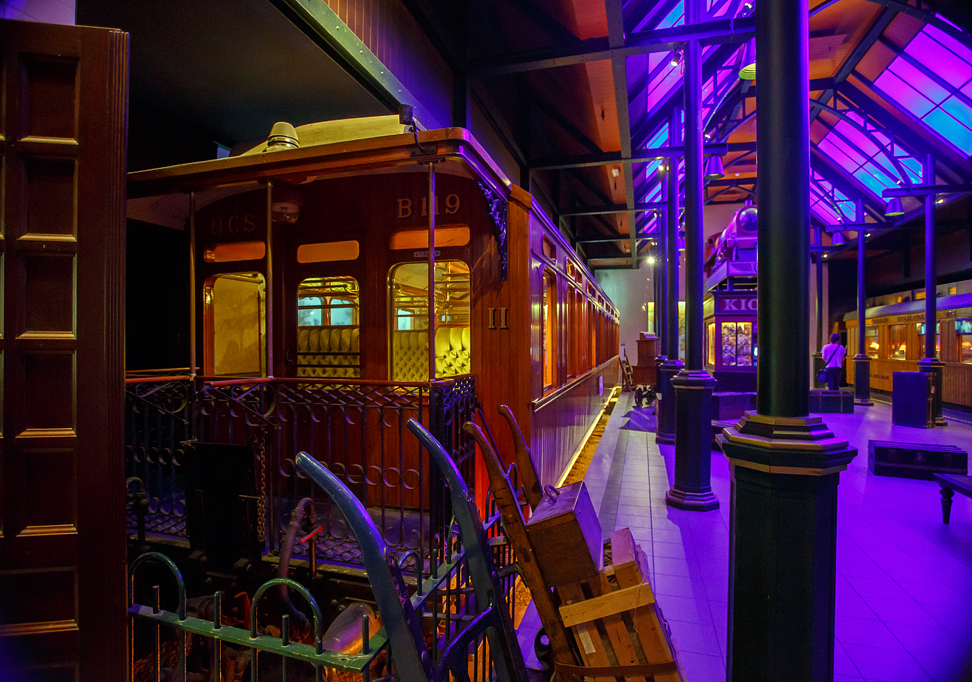 Der zweite Klasse Reisezugwagen NCS B 119, ein luxuriöser Teakholzwagen der ehemaligen NCS - Nederlandsche Centraal Spoorwegmaatschappij (Niederländische Zentralbahngesellschaft) am 24. Juni 2025 im Het Spoorwegmuseum (bis 2005 NSM - Nederlands Spoorwegmuseum / Niederländischen Eisenbahnmuseum) in Utrecht im ehemaligen Bahnhof Maliebaan. Nicht nur die Compagnie Internationale des Wagons-Lits (CIWL) für ihre Luxuszüg, wie beispielsweise dem Orient-Express, hatte solche Wagen.

Dieser äußerst luxuriösen Abteilwagen vom Typ BL8 (Serie B 111 – 127) wurde 1904 in der eigenen Werkstatt der NCS in Utrecht (Werkplaats NCS) gebaut. 

Bedingt durch den Ersten Weltkrieg wurde 1917 eine Zweckgemeinschaft der unabhängigen Eisenbahngesellschaften HSM beziehungsweise HIJSM (Hollandsche IJzeren Spoorweg-Maatschappij) und SS (Maatschappij tot Exploitatie van Staatsspoorwegen) gegründet. Da die NCS unter der Kontrolle der SS stand, wurde sie von diesem Moment an auch Teil der neuen Partnerschaft. Der Betrieb wurde am 1. Juni 1919 an die SS übertragen. Die beiden Gesellschaften errichteten einen gemeinsamen Bahnbetrieb, blieben aber rechtlich unabhängig. Dies änderte sich 1938, als HIJSM und SS vollständig fusionierten und in der AG NS (Nederlandse Spoorwegen, früher Nederlandsche Spoorwegen geschrieben) aufgingen. Das Rollmaterial wurde bereits 1921 zusammengelegt. Somit wurde ab 1924 der Wagen als NS B 1814 geführt, 1952 wurde er außer Dienst gestellt und für das Eisenbahnmuseum erhalten. Er kam 1977 vollständig restauriert als NCS B 119 dort an. Seitdem ist ein Paradewagen des Museums.

Anfang des 20. Jahrhundert war es den lokalen Eisenbahnen in den Niederladen gesetzlich verboten Waggons der 1. Klasse einzusetzen. Um doch wohlhabende Passagiere von Zeist und Baarn (einschließlich des Direktors der NCS) in passender Art zu befördern umging die NCS mit diesen als 2. Klasse Wagen klassifizierten äußerst luxuriösen Standard. Neben den teakholzgetäfelten Außenwänden ist auch der Innenraum opulent und gepflegt. Zu beiden Seiten des Mittelgangs befinden sich gepolsterte Doppelbänke mit Wendekissen. Im Winter war die plüschige Seite oben, im Sommer die kühlere, lederbezogene Seite. Lampen, Gepäckablagen, Aschenbecher, alles ist wunderschön verarbeitet und aus Kupfer gefertigt. Die Waggons wurden unter anderem auf den (Lokal-)Bahnen Utrecht–Den Dolder–Baarn und Utrecht–Bilthoven–Zeist eingesetzt. Insgesamt gab es siebzehn dieser Wagen.

TECHNISCHE DATEN:
Baujahr: 1904 (Ausmusterung 1952)
Spurweite: 1.435 mm (Normalspur)
Achsen: 4 (in 2 Drehgestellen)
Achsfolge: 2'2'
Länge über Puffer: 17.540 mm
Höchstgeschwindigkeit: 80 km/h
Sitzplätze: 56 in 8 Abteilen
