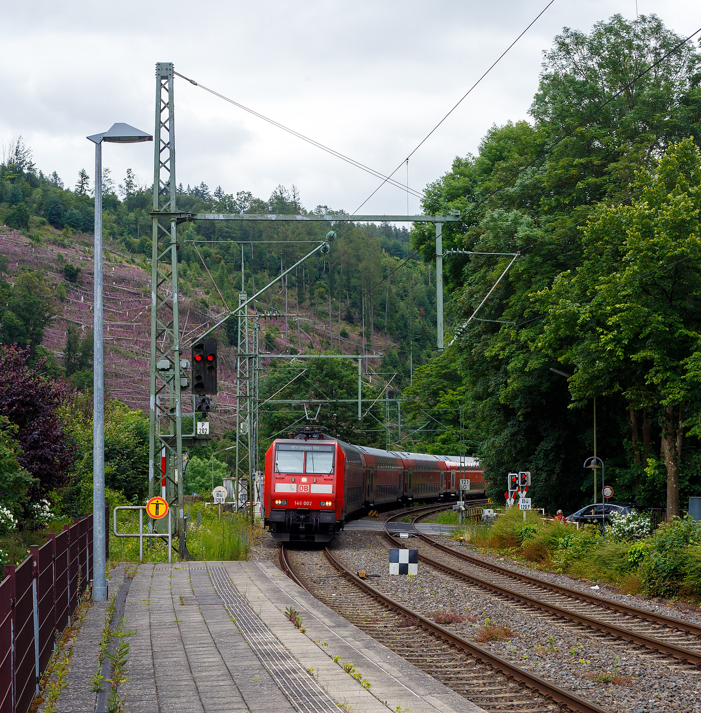 Die 146 002-1 (91 80 6146 002-1 D-DB) der DB Regio NRW passiert am 10 Juni 2024, mit dem RE 9 (rsx - Rhein-Sieg-Express) Aachen - Köln – Siegen, den Bahnübergang Bü 120,9 der Siegstecke (KBS 460) und erreicht so mit ca. 25 Minuten Verspätung den Bahnhof Kirchen/Sieg.

Die TRAXX P160 AC1 wurde 2001 von Adtranz in Kassel unter der Fabriknummer 33809 gebaut.
