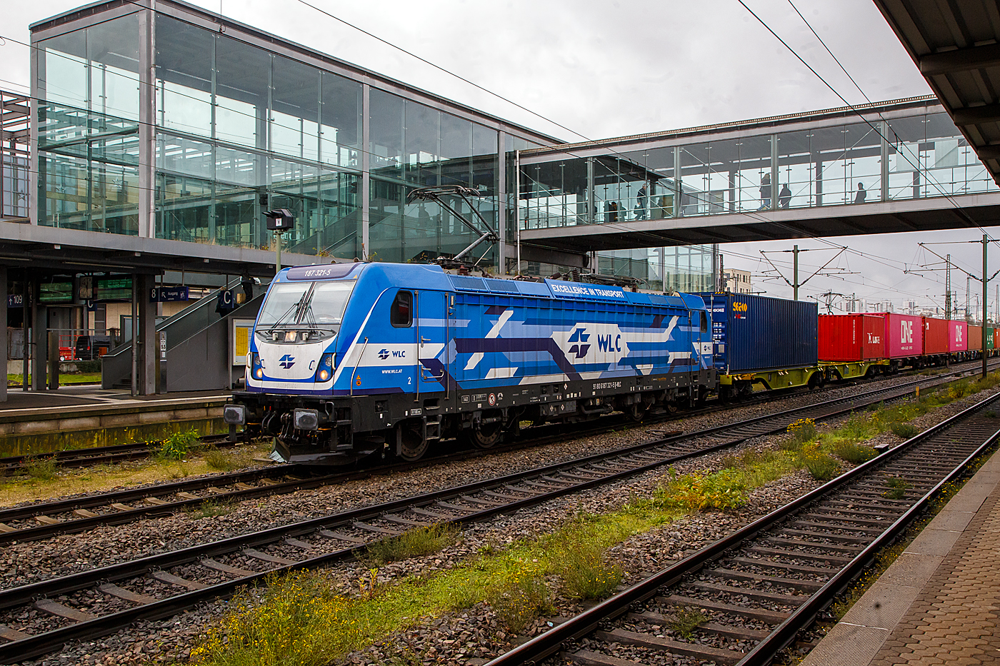 Die 187 321-5 (91 80 6187 321-5 D-WLC) der WLC - Wiener Lokalbahnen Cargo GmbH (Wien) fährt am 24.11.2022 mit einem Containerzug durch den Hauptbahnhof Regensburg.

Die Lok Bombardier TRAXX F140 AC3 LM (zugelassen für 140 km/h daher Variante F140 und nicht F 160). Sie wurde 2017 von Bombardier in Kassel unter der Fabriknummer 35229 gebaut und an die WLC - Wiener Lokalbahnen Cargo GmbH (Wien). Nach meiner Sichtung hat die Lok die Zulassung für Deutschland (D) und Österreich (A). Für Ungarn und Rumänien sind die Zulassungen noch nicht erteilt (H und RO sind durchgestrichen).

Wie die Vorgängerinnen AC1 und AC2 ist die AC3 für den Betrieb unter 15 Kilovolt bei 16,7 Hertz, sowie unter 25 Kilovolt bei 50 Hertz Wechselstrom ausgelegt, und verfügt unverändert über eine Dauerleistung von 5.600 kW ( Power Boost  von 6.000 kW) und eine Anfahrzugkraft von 300 kN. Von den Traxx 2E übernommen wurde der Maschinenraum mit Seitengang um das sogenannte Powerpack, bestehend aus Stromrichter und Hochspannungsgerüst, womit erstmals alle Varianten dasselbe Layout verwenden.

Neu ist die Kopfform der Traxx-3-Lokomotiven, im Wesentlichen ein auf dem Lokkasten aufgesetztes GFK-Modul. Zudem wurden die Lokomotiven erstmals ab Werk konstruktiv für den Einbau der Zugbeeinflussung ETCS vorbereitet. Neuerungen betreffen die verfügbaren Drehgestelle: zu den bisherigen Varianten „F140“ mit Tatzlagerantrieb und Zulassung für maximal 140 km/h, und „P160“ mit Hohlwellenantrieb und Zulassung für maximal 160 km/h, werden die Traxx-3-Lokomotiven offiziell auch als Variante „F160“ mit Tatzlagerantrieb und Zulassung für maximal 160 km/h angeboten. Es gibt sie also als TRAXX F140 AC3 und als TRAXX F160 AC3.

Gänzlich neu sind die optional verfügbaren Last-Mile-Module, die es als Last-Mile-Diesel (LMD) mit zusätzlicher Last-Mile-Battery (LMB) gibt. Das LMD besteht aus einem Dieselhilfsmotor und einem Kraftstofftank, um auch nicht-elektrifizierte Streckenabschnitte und Anschlussgleise befahren zu können. Der Dieselmotor von Deutz verfügt über einen Hubraum von 7.150 cm³, erbringt eine Leistung von 230 kW (180 kW am Rad), mit Batterieunterstützung 290 kW und erfüllt die Stage-IIIB-Abgasnorm. Im Dieselbetrieb werden alle vier Fahrmotoren betrieben, die Anfahrzugkraft beträgt dabei mit Batterieunterstützung unverändert 300 kN, ohne Batterie 260 kN. Ohne Anhängelast ist damit eine Höchstgeschwindigkeit von 60 km/h möglich, bei 2000 Tonnen Last noch 40 km/h. Der Tankinhalt von 400 Litern reicht für bis zu acht Stunden Dieselbetrieb, kurze Strecken können auch ausschließlich mit der eingebauten Batterie zurückgelegt werden. Der Übergang vom elektrischen zum Dieselbetrieb kann während der Fahrt erfolgen. Für den Rangierbetrieb ist zudem eine Funkfernsteuerung erhältlich.

Erstmals wurde der Lokkasten nicht mit glatten Seitenwänden gefertigt, sondern konstruktiv deutlich günstiger, sind die Seitenwände der AC3 vertikal gesickt und die Seitenflächen erhielten sogenannte Flex-Panels, eine Vorrichtung zum Einspannen von Planen. Diese würden die Sicken verdecken, und wären kostengünstiger als Umlackierungen oder Umbeklebungen. Die Nutzung der Flex-Panels wurde jedoch in der Schweiz umgehend untersagt.

TECHNISHE DATEN:
Hersteller: 	Bombardier Transportation
Spurweite: 	1.435 mm (Normalspur)
Achsanordnung: Bo’ Bo’
Länge über Puffer: 18.900 mm
Drehzapfenabstand: 10.440 mm
Achsabstand im Drehgestell: 2.600 mm
Treibraddurchmesser: 	1.250 mm (neu) / 1.170 mm (abgenutzt)
Höhe:  4.283 mm
Breite:  2.977 mm
Lichtraumprofil: UIC 505-1
Dienstgewicht: 87 t
Fahrmotoren: 4 Asynchronmotoren
Bremse: Elektrische Bremse (SW-GPR-E mZ)

Daten im Oberleitungsbetrieb:
Höchstgeschwindigkeit: 160 km/h
Dauerleistung: 5.600 kW 
Kurzzeitleistung  Power Boost : 6.000 kW
Anfahrzugkraft: 300 kN
Dauerzugkraft: 252 kN bei 80 km/h
Stromsystem: 15 kV 16,7 Hz~ und 25 kV 50 Hz~

Daten im Dieselbetrieb (Last-Mile):
Nenndrehzahl: 1.800 U/min
Höchstgeschwindigkeit: 60 km/h
Dauerleistung: 320 kW (Quelle WLC)
Tankinhalt:  400 l

