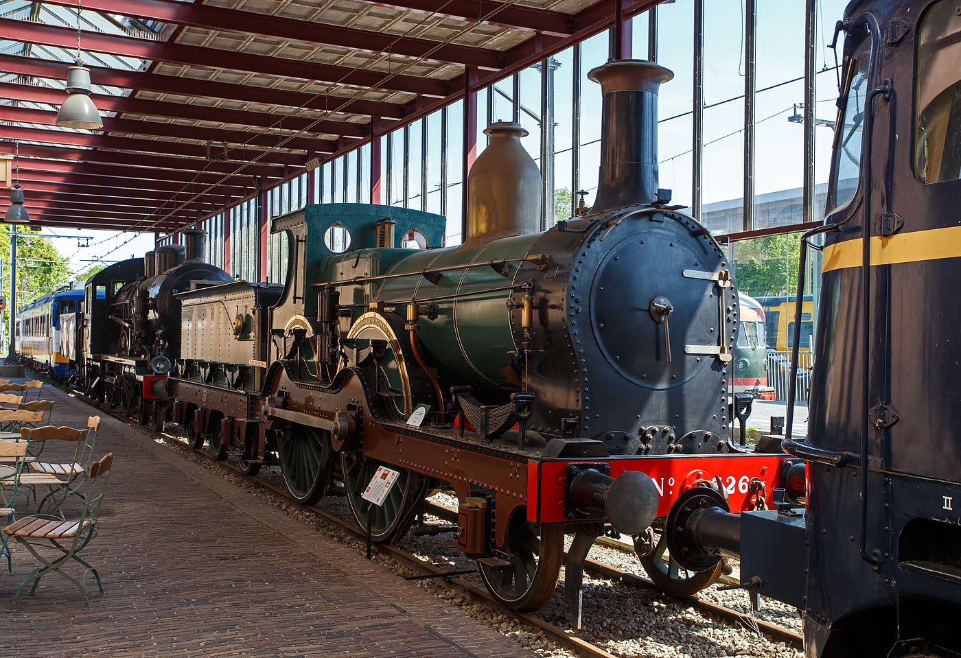 Die 1881 gebaute 1B Dampflokomotive SS 326 „Grote Groenen“ (Große Grüne), ab 1921 NS 1326 (NS-Baureihe 1300), am 29 April 2025 im Het Spoorwegmuseum (bis 2005 NSM - Nederlands Spoorwegmuseum / Niederländischen Eisenbahnmuseum) in Utrecht im Bahnhof Maliebaan.   

Die Dampflok wurde 1881 von Beyer Peacock & Co. Ltd. in Manchester (GB) unter der Fabriknummer 2101 gebaut und an die damalige SS - Maatschappij tot Exploitatie van Staatsspoorwegen (deutsch: Gesellschaft zum Betrieb von Staatseisenbahnen) geliefert. Ab 1921, nach der Zusammenlegung des Rollmaterials der SS und der NRS, wurde die Lok zur NS 1326. Die Lokomotive 1326 wurde 1939 außer Dienst gestellt und für das Eisenbahnmuseum erhalten. Am Ende des Zweiten Weltkriegs wurde sie von den zurückweichenden Deutschen Truppen in Maastricht schwer beschädigt. Im Jahr 1956 wurde sie schließlich von der Hauptwerkstatt in Tilburg in ihren Originalzustand zurückversetzt und anschließend ins Eisenbahnmuseum gebracht. Die Lokomotive 326 gilt als eines der Meisterwerke des Museums.

Die NS 1300-Serie war eine Serie von 179 Dampflokomotiven der Niederländischen Eisenbahnen (NS), die zwischen 1880 und 1895, an ihre Vorgängergesellschaften, Maatschappij tot Exploitatie van Staatsspoorwegen (SS) und Noord-Brabantsch-Duitsche Spoorweg-Maatschappij (NBDS) geliefert wurden.

Durch die Erfindung und Anwendung der kontinuierlichen Druckluftbremse (Westinghouse-Bremse) konnte die Geschwindigkeit der Züge bei gleichbleibendem Bremsweg deutlich erhöht werden. Dafür waren nun leistungsstärkere und schnellere Lokomotiven erforderlich, die die Maatschappij tot Exploitatie van Staats-Spoorwegen (SS) in diesem Lokomotiventyp vorfand. Das niederländisch-englische Design der Baureihe 301 – 479 (NS 1301 – 1479) erwies sich als sehr geeignet für den Schnellzugdienst, war aber auch im Güterverkehr nützlich. Die Lokomotiven wurden über einen Zeitraum von 15 Jahren gebaut und bildeten mit insgesamt 179 Stück die größte jemals von der SS und NS betriebene Dampflokomotiven-Baureihen. Sie fuhren auf allen wichtigen Staatsbahnstrecken im ganzen Land, einschließlich der schweren Postzüge zwischen Vlissingen und Venlo. 

Die eindrucksvollen Lokomotiven, die für die damalige Zeit in einem hellgrünen Farbton mit braunen Rahmenplatten lackiert waren, erhielten bald ihren Spitznamen „Grote Groenen“ (Große Grüne). 1919 wurde die Serie um 3 baugleiche Lokomotiven SS 476 – 478 erweitert, die von der Noord-Brabantsch – Duitsche Spoorweg-Maatschappij (NBDS 6, 7 und 11) stammten. Schließlich wurde die abweichende Verbundmaschine 701 mit einem Hoch- und einem Niederdruckzylinder weitgehend der Serie angeglichen und in 479 um nummeriert.

Bedingt durch den Ersten Weltkrieg wurde 1917 eine Zweckgemeinschaft der unabhängigen Eisenbahngesellschaften HSM (Hollandsche IJzeren Spoorweg-Maatschappij) und SS (Maatschappij tot Exploitatie van Staatsspoorwegen) gegründet. Die beiden Gesellschaften errichteten einen gemeinsamen Bahnbetrieb, blieben aber rechtlich unabhängig. Dies änderte sich 1938, als HIJSM und SS vollständig fusionierten und in der AG NS (Nederlandse Spoorwegen, früher Nederlandsche Spoorwegen geschrieben) aufgingen. Das Rollmaterial wurde bereits 1921 zusammengelegt, so wurden die Lok zur NS 1326 nummeriert. 

Die dreiachsigen Tender der SS 301-398 hatten einen Wasserinhalt von 10,3 m³. Ab der 399 wurde der Wasserinhalt der Tender durch eine Vertiefung zwischen den Rahmenplatten auf 13 m³ erhöht. Später wurde die Wasserkapazität der Tender der Linien 301–398 auf die gleiche Weise erhöht.
	
TECHNISCHE DATEN:
SS-Serie: Grote Groenen, ab 1921 NS 1300
Hersteller: Beyer Peacock & Co. Ltd. in Manchester (GB)
Gebaute Anzahl: 179
Spurweite: 1.435 mm (Normalspur)
Achsfolge: 	1 B (engl. 2-4-0), gekuppelt mit dreiachsigem Tender
Länge über Puffer: 15.395 mm
Treibraddurchmesser: 2.150 mm (neu) / 2134 mm (abgenutzt)
Laufraddurchmesser (Lok und Tender): 1.240 mm (neu) / 1.219 mm (abgenutzt)
Höhe: 4.115 mm
Höchstgeschwindigkeit: 90 km/h
Rostfläche: 2,10 m²
Gesamtheizfläche: 103 m²
Kesselüberdruck: 10,3 kg/cm²
Anzahl der Zylinder: 2 (Ø 457 mm x 660 mm Hub)
Steuerung: Stephenson
Eigengewicht: 75 t (Lok 42 t und Tender 33 t)
Anhängelast: 4.620 kg
Wasservorrat: 13 m³ (urspr. 10,3 m³)
Kohlevorrat: 4 t
