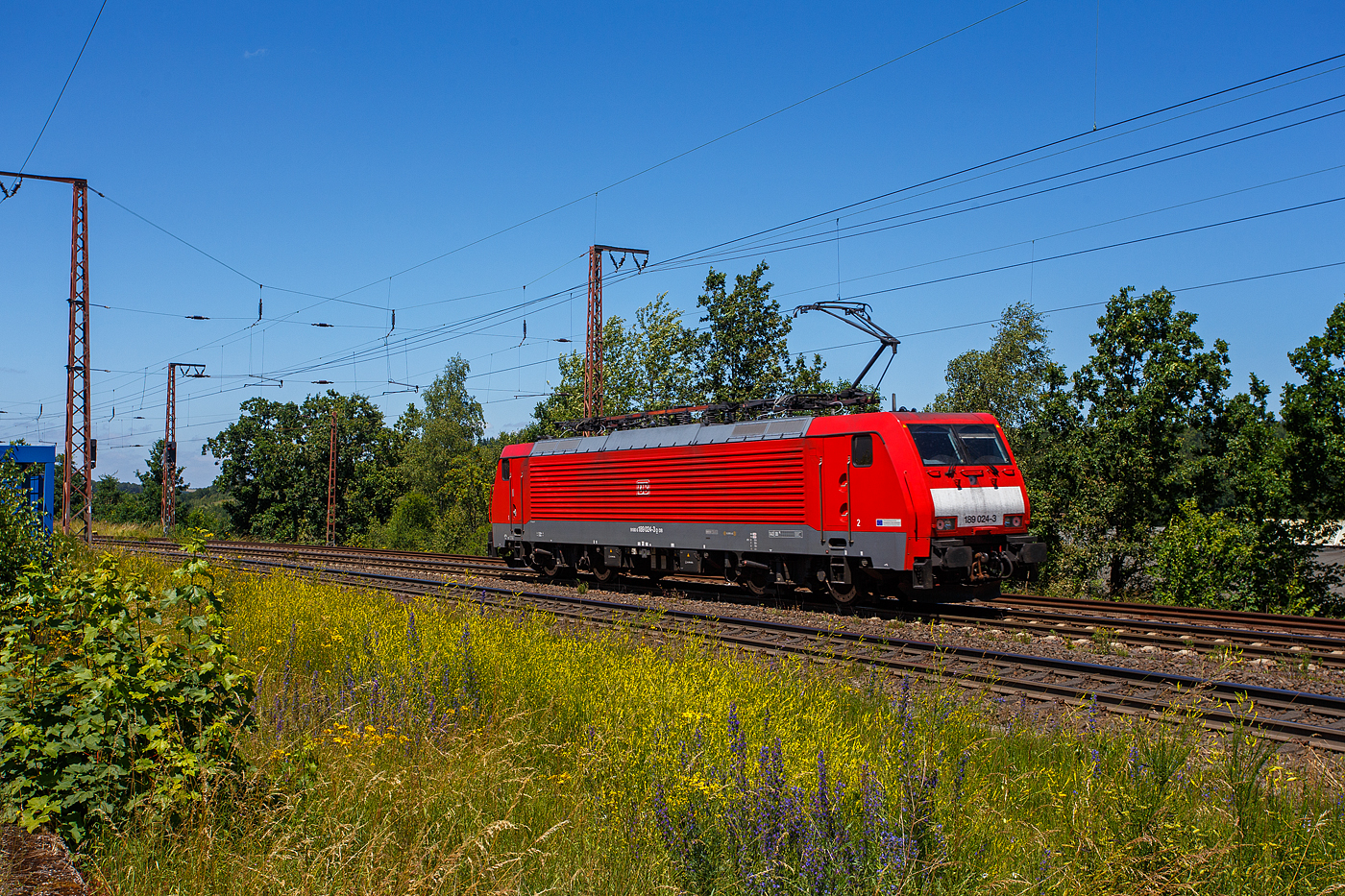 Die 189 024-3 (91 80 6189 024-3 D-DB) der DB Cargo AG rauscht am 28 Juni 2024, als Lz (Lokzug)/ auf Tfzf (Triebfahrzeugfahrt) durch Ruderdorf (Kreis Siegen) in Richtung Siegen.

Die SIEM;ENS ES 64 F4(EuroSprinter) wurde 2003 von SIEMENS in München-Allach unter der Fabriknummer 20699 gebaut und an die damalige Railion Deutschland AG (heute DB Cargo AG) in der Variante A ausgeliefert und war nur für Deutschland zugelassen. 2007 wurde sie in die Variante J umgebaut und besitzt nun die Zugbeeinflussungssysteme LZB/PZB, ETCS und ATB für
den Einsatz in Deutschland und den Niederlanden.

Die Stromabnehmerbestückung ist folgende: 
Pos. 1: D, NL (AC)
Pos. 2: NL (DC)
Pos. 3: NL (DC)
Pos. 4: D, NL (AC)

Die Elektrolokomotive ES64F4 ist eine Variante der EuroSprinter-Lokfamilie von Siemens Mobility (vormals Siemens Transportation Systems) mit Vier-Stromsystem-Ausstattung. In Deutschland ist sie vor allem als Baureihe 189 der Deutschen Bahn im Einsatz. Sie ist in allen vier in Europa üblichen Bahnstromsystemen einsetzbar. Für die verschiedenen Bahngesellschaften können die jeweils erforderlichen Zugsicherungssystem-Komponenten als „Paket“ installiert werden.

Die Lokomotiven haben eine elektrische Bremse und Scheibenbremsen. Diese sind wegen der vergleichsweise geringen zulässigen Höchstgeschwindigkeit von 140 km/h und aus Kostengründen als Radscheibenbremsen ausgeführt und nicht, wie bei Lokomotiven des Typs ES 64 U2, auf gesonderten Bremswellen angebracht. Die Konstruktion der Lok ist aber so ausgelegt, dass auch eine Version mit einer Höchstgeschwindigkeit von 230 km/h möglich ist.

Der ölgekühlte Transformator ist unterflur angeordnet, während er in der herkömmlichen Bauweise im Lok-Kasten untergebracht war. Dadurch wurde im Lokkasten ein durchgehender Mittelgang zwischen den Führerständen ermöglicht. Beiderseits des Mittelgangs befinden sich die Stromrichter-Gestelle. Je ein Stromrichtersatz versorgt die Fahrmotoren eines Drehgestelles. Er besteht aus Gleichrichtern, die die Sekundärspannung des Transformators zunächst in Gleichstrom umwandeln, sowie jeweils drei Motorstromrichtersätzen. Zur Glättung der Zwischenkreis-Gleichspannung sind Stützkondensatoren und Saugkreisdrosseln vorhanden. Die zeitlich versetzt taktenden Motorstromrichter formen den Gleichstrom in Drehstrom um und versorgen die Fahrmotoren einzeln. Dadurch können diese auch einzeln geregelt und der Reibwert Rad-Schiene optimal ausgenutzt werden.


Beim Betrieb in Gleichstrom-Netzen wird die Fahrleitungsspannung direkt in die Zwischenkreise eingespeist, wobei die Sekundärwicklungen des Trafos als Netzfilterdrossel genutzt werden.

Die Stromrichter ermöglichen zusammen mit der elektrischen Bremse auch eine Bremsstrom-Rückspeisung mit einer Bremsleistung von theoretisch 6,4 MW. Die Bremskraft ist aber aus Gründen der Entgleisungssicherheit auf 150 kN begrenzt.

TECHNISCHE DATEN:
Spurweite: 1.435 mm (Normalspur)
Achsformel: Bo’Bo’
Länge über Puffer: 19.580 mm
Drehzapfenabstand: 9.900 mm
Achsstand im Drehgestell: 2.900 mm
Treibraddurchmesser: 1.250 mm (neu)
Dienstgewicht: 87 t
Stundenleitung: 6.400 kW bei 15 kV / 25 kV AC; 6.000 kW bei 3 kV DC und 3.000 kW bis 4.200 kW bei 1,5 kV DC
Anfahrzugkraft: 300 kN
Maximale Dauerzugkraft bis 84 km/h; 270 kN
Höchstgeschwindigkeit: 140 km/h
E-Bremskraft max.: 150 kN
Stromsysteme: 15 kV, 16,7 Hz AC; 25 kV, 50 Hz AC; 1,5 kV und 3 kV DC 
Kleinster befahrbarer Gleisbogen: R = 80 m