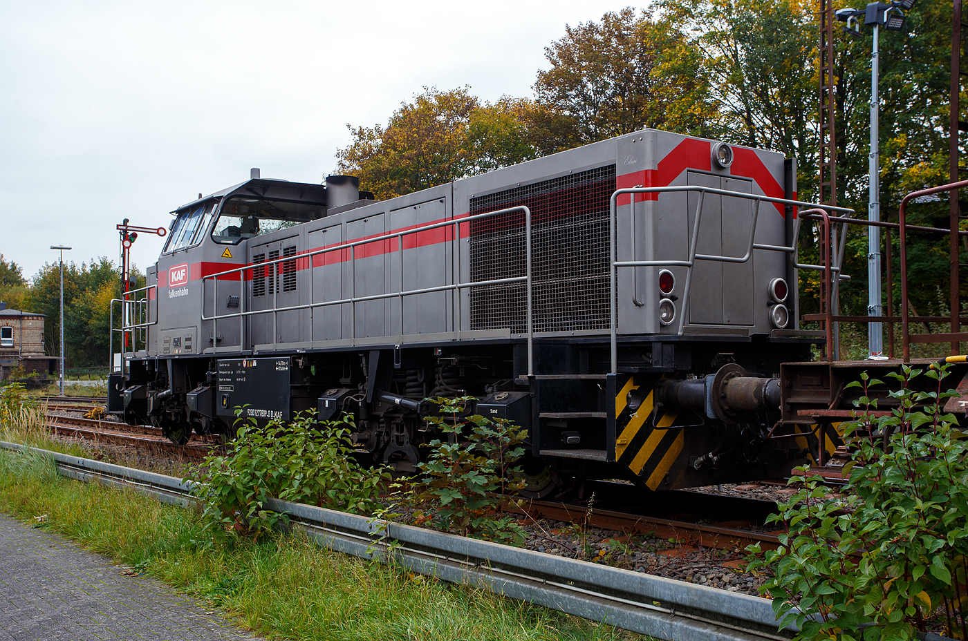 Die 277 809-0  Elmi“ (92 80 1277 809-0 D-KAF), eine Vossloh MaK G 1700 BB der KAF - Falkenhahn Bau AG (Kreuztal), steht am 12 Oktober 2025 mit einem Schotterzug im Bahnhof Herdorf. Mit dem Zug werden später die neuen Weichen 25 und 26 eingeschottert. 

Die Vossloh MaK G 1700 BB wurde 2001 von Vossloh in Kiel 2001 unter der Fabriknummer 1001113 gebaut und an die NE - Neusser Eisenbahn geliefert. Nach dem Zusammenschluss der HGK und der NE zur RheinCargo GmbH & Co. KG, fuhr sie noch als RHC 277 809-0. Anfang 2014 ging sie an die Vossloh Locomotives GmbH (92 80 1277 809-0 D-VL) und war 1 ½ Jahre als Mietlok unterwegs, bis sie im Juni 2015 an die Michael Bugdoll Bau- und Sicherungsarbeiten e. K in Dorsten ging, als diese konnte ich sie auch mal ablichten. Seit 01.01.2021 ist die Lok nun bei der KAF - Falkenhahn Bau AG (Kreuztal), hier hat sie aber ihren Namen  Elmi“ behalten. 

TECHNISCHE DATEN:
Baujahr: 2001 - 2003
gebaute Stückzahl: 6
Spurweite: 1.435 mm (Normalspur)
Achsfolge: B´B´
Länge über Puffer: 14.700 mm
Drehzapfenabstand: 7.400 mm
Achsabstand im Drehgestell: 2.400 mm
größte Breite: 3.080 mm
größte Höhe über Schienenoberkante: 4.220 mm
Raddurchmesser: 1.000 mm (neu)
kleinster befahrbarer Gleisbogen: 60 m
Dienstgewicht 87,3 t
Kraftstoffvorrat 3.500 l
Motor: MTU-12-Zylinder-Dieselmotor, vom Typ 12V 4000 R20
Leistung: 1.500 kW bei 1800 U/min
Getriebe: Voith L 5r4 zU2
Anfahrzugkraft: 249 kN
Höchstgeschwindigkeit: 100 km/h

Die Vossloh Lokomotive MaK G 1700 BB ist eine dieselhydraulische Lokomotive. Bei der Überarbeitung der Typenpalette nach der Übernahme der MaK durch Vossloh 1998 wurde im 4. Typenprogramm unter der Bezeichnung G 1700 BB der Bau einer vierachsigen Streckenlokomotive mit Mittelführerhaus vorgesehen. Tatsächlich handelte sich zunächst um eine Weiterentwicklung der G 1206. Die Maschine wurde in einigen Details an die Lokomotiven des 4. Typenprogramms angepasst. Dies betraf in erster Linie den Rahmen, der so geändert wurde, dass die neuen Standarddrehgestelle verwendet werden konnten. Dabei wurden die Rahmenenden so umgestaltet, dass die Lokomotiven die im 4. Typenprogramm üblichen Komfortaufstiege erhielten. Ebenfalls geändert wurde der Dieselmotor. Zum Einsatz kam der schon bei den G 1206 für die Dortmunder Eisenbahn verwendete MTU 12V 4000 R20 mit einer unveränderten Leistung von 1.500 kW bei 1.800 U/min. Die übrigen Komponenten der G 1700 BB blieben gegenüber der G 1206 weitgehend unverändert.

Der Dieselmotor ist ein wassergekühlter MTU 90°-V12-Zylinder-Viertakt-Dieselmotor mit Common-Rail-Einspritzung, OHV-Ventilsteuerung, Registeraufladung mit Ladeluftkühlung. Der Hubraum beträgt 57.199 cm³ (57,2 Liter), die Zylinder haben eine Bohrung von Ø 170 mm × 210 mm Hub. Die Motorabmessungen (LxBxH) sind 2.670 x 1.696 x 2.001 mm, das Gewicht (trocken) beträgt 7.700 kg.

Die ersten beiden Lokomotiven dieses Typs (die KSW Lok 42 und diese hier) wurden im Jahr 2001 ausgeliefert. Ende 2002 bis Anfang 2003 folgten weitere vier Lokomotiven aus Vorratsbauten. Nach diesen sechs Lokomotiven wurde der Bau der G 1700 BB zugunsten der technisch sehr ähnlichen und bereits weiter verbreiteten G 1206 wieder eingestellt.

So ist der Nachfolger die G 1700-2 BB keine Weiteentwicklung der G 1700 BB, sondern um eine komplette Neuentwicklung. 
