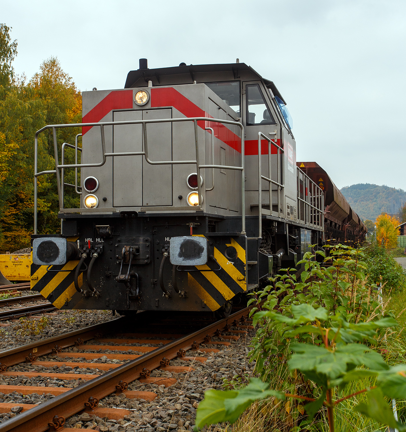 Die 277 809-0  Elmi“ (92 80 1277 809-0 D-KAF), eine Vossloh MaK G 1700 BB der KAF - Falkenhahn Bau AG (Kreuztal), steht am 12 Oktober 2025 mit einem Schotterzug im Bahnhof Herdorf. Mit dem Zug werden später die neuen Weichen 25 und 26 eingeschottert. 

Die Vossloh MaK G 1700 BB wurde 2001 von Vossloh in Kiel 2001 unter der Fabriknummer 1001113 gebaut und an die NE - Neusser Eisenbahn geliefert. Nach dem Zusammenschluss der HGK und der NE zur RheinCargo GmbH & Co. KG, fuhr sie noch als RHC 277 809-0. Anfang 2014 ging sie an die Vossloh Locomotives GmbH (92 80 1277 809-0 D-VL) und war 1 ½ Jahre als Mietlok unterwegs, bis sie im Juni 2015 an die Michael Bugdoll Bau- und Sicherungsarbeiten e. K in Dorsten ging, als diese konnte ich sie auch mal ablichten. Seit 01.01.2021 ist die Lok nun bei der KAF - Falkenhahn Bau AG (Kreuztal), hier hat sie aber ihren Namen  Elmi“ behalten. 

TECHNISCHE DATEN:
Baujahr: 2001 - 2003
gebaute Stückzahl: 6
Spurweite: 1.435 mm (Normalspur)
Achsfolge: B´B´
Länge über Puffer: 14.700 mm
Drehzapfenabstand: 7.400 mm
Achsabstand im Drehgestell: 2.400 mm
größte Breite: 3.080 mm
größte Höhe über Schienenoberkante: 4.220 mm
Raddurchmesser: 1.000 mm (neu)
kleinster befahrbarer Gleisbogen: 60 m
Dienstgewicht 87,3 t
Kraftstoffvorrat 3.500 l
Motor: MTU-12-Zylinder-Dieselmotor, vom Typ 12V 4000 R20
Leistung: 1.500 kW bei 1800 U/min
Getriebe: Voith L 5r4 zU2
Anfahrzugkraft: 249 kN
Höchstgeschwindigkeit: 100 km/h

Die Vossloh Lokomotive MaK G 1700 BB ist eine dieselhydraulische Lokomotive. Bei der Überarbeitung der Typenpalette nach der Übernahme der MaK durch Vossloh 1998 wurde im 4. Typenprogramm unter der Bezeichnung G 1700 BB der Bau einer vierachsigen Streckenlokomotive mit Mittelführerhaus vorgesehen. Tatsächlich handelte sich zunächst um eine Weiterentwicklung der G 1206. Die Maschine wurde in einigen Details an die Lokomotiven des 4. Typenprogramms angepasst. Dies betraf in erster Linie den Rahmen, der so geändert wurde, dass die neuen Standarddrehgestelle verwendet werden konnten. Dabei wurden die Rahmenenden so umgestaltet, dass die Lokomotiven die im 4. Typenprogramm üblichen Komfortaufstiege erhielten. Ebenfalls geändert wurde der Dieselmotor. Zum Einsatz kam der schon bei den G 1206 für die Dortmunder Eisenbahn verwendete MTU 12V 4000 R20 mit einer unveränderten Leistung von 1.500 kW bei 1.800 U/min. Die übrigen Komponenten der G 1700 BB blieben gegenüber der G 1206 weitgehend unverändert.

Der Dieselmotor ist ein wassergekühlter MTU 90°-V12-Zylinder-Viertakt-Dieselmotor mit Common-Rail-Einspritzung, OHV-Ventilsteuerung, Registeraufladung mit Ladeluftkühlung. Der Hubraum beträgt 57.199 cm³ (57,2 Liter), die Zylinder haben eine Bohrung von Ø 170 mm × 210 mm Hub. Die Motorabmessungen (LxBxH) sind 2.670 x 1.696 x 2.001 mm, das Gewicht (trocken) beträgt 7.700 kg.

Die ersten beiden Lokomotiven dieses Typs (die KSW Lok 42 und diese hier) wurden im Jahr 2001 ausgeliefert. Ende 2002 bis Anfang 2003 folgten weitere vier Lokomotiven aus Vorratsbauten. Nach diesen sechs Lokomotiven wurde der Bau der G 1700 BB zugunsten der technisch sehr ähnlichen und bereits weiter verbreiteten G 1206 wieder eingestellt.

So ist der Nachfolger die G 1700-2 BB keine Weiteentwicklung der G 1700 BB, sondern um eine komplette Neuentwicklung. 