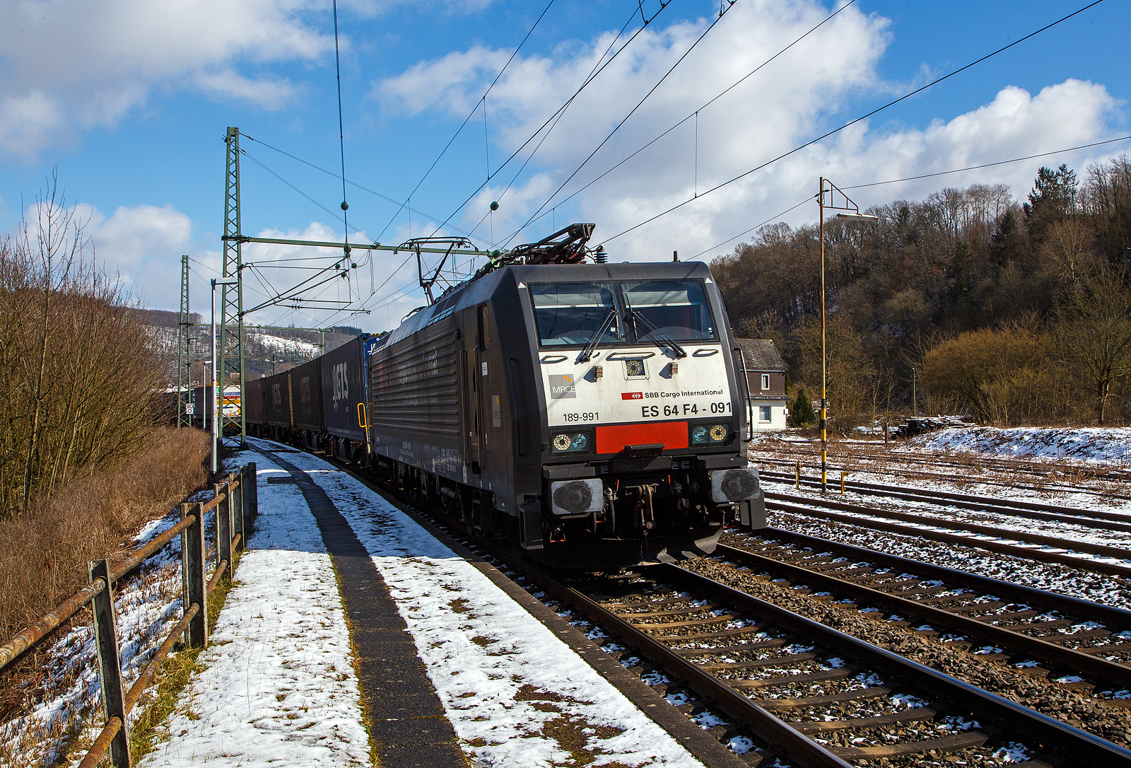 Die an die SBB Cargo International AG vermietete MRCE Dispolok ES 64 F4 - 091 bzw. 189-991 / LZB 189 991-3 (91 80 6189 991-3 D-DISPO, Class 189-VE) fährt am 15.03.2023, mit einem KLV-Zug auf der Siegstrecke (KBS 460) durch Scheuerfeld (Sieg) in Richtung Köln.

Die SIEMENS EuroSprinter wurde 2004 von SIEMENS in München-Allach unter der Fabriknummer 20739 gebaut.

Die BR 189 (Siemens ES64F4) hat eine Vier-Stromsystem-Ausstattung. Sie ist in allen vier in Europa üblichen Bahnstromsystemen einsetzbar. Diese hier hat die Variante E und besitzt die Zugbeeinflussungssysteme LZB/PZB, ETCS, SCMT, ZUB, INTEGRA und ATB für den Einsatz in Deutschland, Österreich, Schweiz, Italien, Niederlande, Slowenien und Rumänien.

Die Stromabnehmerbestückung ist folgende:
Pos. 1: CH, FR (AC), LU (AC), BE (AC)
Pos. 2: IT, SI, HR (DC)
Pos. 3: NL (DC), CZ (DC), FR (DC), SK, LU (DC)
Pos. 4: DE, AT, NL (AC), DK, CZ (AC), HR (AC), HU, RO
