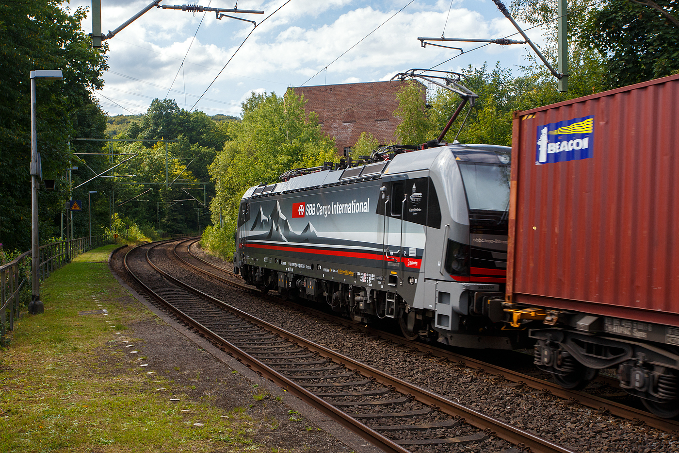 Die an die SBB Cargo International AG vermietete mit XLoad ausgestattete SIEMENS Vectron 193 542  Kapellbrücke Luzern  (91 80 6193 542-8 D-SIEAG) der SüdLeasing GmbH, Stuttgart (eingestellt in Deutschland durch Siemens) fährt am 21 August 2025, mit einem KLV-Zug, durch Scheuerfeld/Sieg in Richtung Köln.

Die Multisystemlokomotive Siemens Vectron MS wurde 2024 von Siemens Mobilitiy in München-Allach unter der Fabriknummer 23559 gebaut und am 19.09.2024 ausgeliefert. Sie wurde in der Variante A40-1a ausgeführt und hat so die Zulassung für Deutschland, Österreich, die Schweiz, Italien, die Niederlande und Belgien (D / A / CH / I / NL / B). Sie verfügt über eine Leistung von 6,4 MW (160 km/h) und ist neben den nationalen Zugsicherungssystemen mit dem Europäischen Zugsicherungssystem (ETCS BL3) ausgestattet. Zudem ist sie mit der neuen Ausrüstungspaket XLoad ausgestattet.

Das neue XLoad Ausrüstungspaket für Vectron:
XLoad ist ein Ausrüstungspaket für Vectron, welches künftig mitbestellt, aber auch bei bereits ausgelieferten Vectron Loks nachgerüstet werden kann. Das Feature verbessert die Reibwertausnutzung und ermöglicht dadurch höhere Anhängelasten. Zudem reduzieren die Fahreigenschaften, die das Feature bewirken, den Verschleiß von Rad und Schiene.

Aktuell sind die Schweizer Vectron-Lokomotiven (SBB Cargo und BLS Cargo) in der Regel in Doppeltraktion unterwegs. Die Steigungen und Rampen der Schweizer Berge sind vor allem bei schlechten Witterungsbedingungen nicht ohne. Eine Lokomotive muss auch bei geringerem Schlupf genügend Traktion auf die Schienen bringen, um alle Güter sicher und zuverlässig ans Ziel zu bringen. Ein effizienter Weg aus dieser «Misere» ist die für Vectron entwickelte Zusatz-Funktion «XLoad». Den erfolgreichen Beweis trat eine SIEMENS Testlokomotive im Frühjahr 2022 bei der SBB Cargo International und bei der BLS Cargo eindrücklich an.

Für SBB Cargo International bewies die Test-Lokomotive am Bözberg und für BLS Cargo an der Nordrampe des Lötschbergs ihre enorme Zugkraft.
Vectron meisterte im Frühjahr 2022 die lange 12‰-Steigung des Bözbergs mit einer Anhängerlast von 2.000 Tonnen bravourös. Bei den nächtlichen Testfahrten zeigte sich eindrücklich die enorme Zugkraft der Lokomotive.

Am Lötschberg wurden bei der BLS Cargo steigungsmäßig noch ein paar Promille draufgepackt. Mit 1.020 Tonnen im Gepäck bewältigte die Vectron-Lokomotive mit XLoad-Feature die 27‰-Steigung der Nordrampe ebenfalls meisterlich. Und auch diverse Anfahrtsversuche absolvierte der mit dem XLoad-Feature aufgerüstete Vectron problemlos.

So bestellte die SüdLeasing GmbH (Stuttgart) im Auftrag der SBB Cargo International jüngst 20 Vectron Lokomotiven mit XLoad bei SIEMENS.