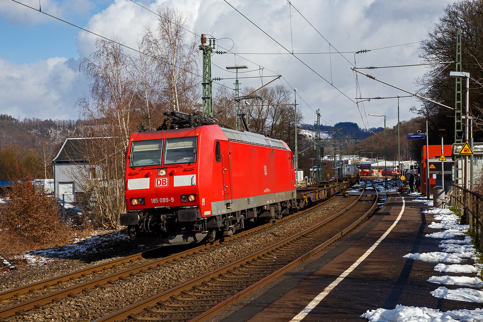 Die auch f�r die Schweiz zugelassene 185 099-9 (91 80 6185 099-9 D-DB) der DB Cargo AG f�hrt am 15.03.2023, mit einem KLV-Zug auf der Siegstrecke (KBS 460) durch Scheuerfeld (Sieg) in Richtung K�ln.

Die TRAXX F140 AC1 wurde 2002 von der Bombardier in Kassel unter der Fabriknummer 33521 gebaut. Sie hat die Zulassung f�r Deutschland und die Schweiz, man kann es auch an den vier DSA-200 Einholm-Stromabnehmer erkennen. Au�en sind jeweils die f�r das Schweizernetz bestimmten Stromabnehmer mit einer 500 mm schmaleren Wippenbreite von 1.450 mm und innen die DB-Netz bestimmten mit einer Wippenbreite von 1.950 mm.
