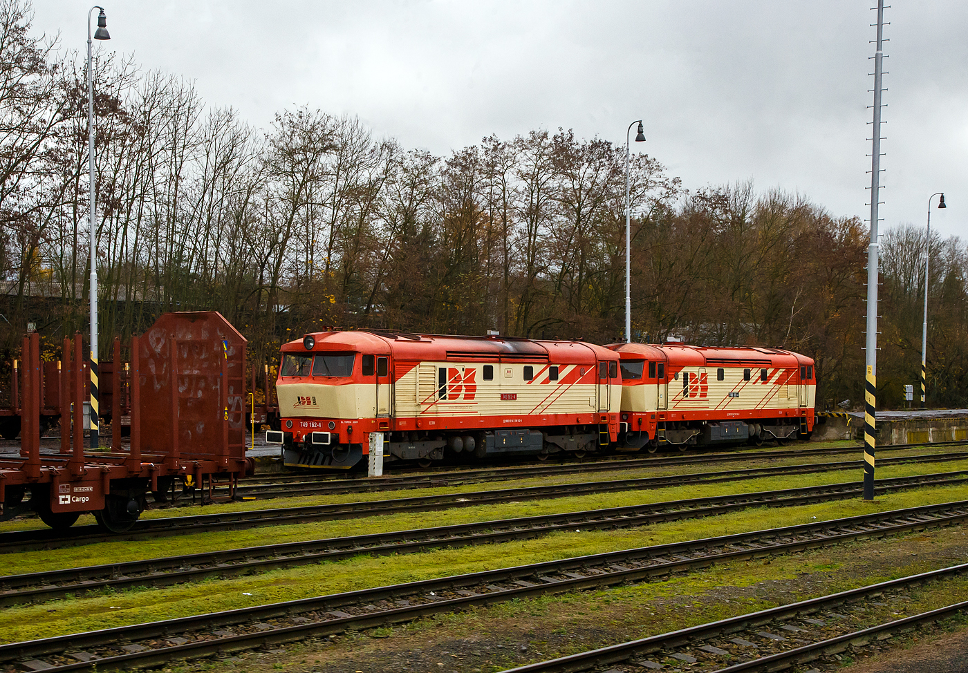 Die beiden „Zamračenás“ (Finstergesichter) 749.162-4 und 749.181-4 (CZ – IDSC 92 54 2 749 162-4 und CZ – IDSC 92 54 2 749 181-4) der IDS Cargo  a.s. (Olomouc / Olmütz) sind am 24.11.2022 beim Bahnhof Domažlice (Taus) abgestellt.

Die 749 162-4 wurde 1969 von ČKD Praha (Českomoravská-Kolben-Daněk, Prag) unter der Fabriknummer 7359 gebaut und als ČSD T 478.1162 an die Československé státní dráhy (Tschechoslowakischen Staatsbahnen) geliefert, 1988 erfolgte die Umzeichnung in ČSD 751 162-9, nach der Auflösung der Tschechoslowakei zum 31. Dezember 1992, blieb sie in Tschechien und wurde zum 01.01.1993 zur ČD751 162-9, im Jahr 1994 wurde sie zur ČD 749 162-4 umgebaut und im Mai 2012 wurde sie an die IDS Cargo  a.s. in Olomouc (Olmütz) verkauft.

Die 749 181-4 wurde 1970 von ČKD Praha unter der Fabriknummer 7673  gebaut und als ČSD T 478.1181 geliefert, ab 1988 ČSD 751 181-9, ab 1993 ČD 751 181-9, im Jahr 1995 umbau zur ČD 749 181-4, im Mai 2012 Verkauf an IDS Cargo  .

Die Lokomotiven der Baureihe 749 sind Diesellokomotiven mit elektrischer Kraftübertragung, die durch Rekonstruktion/ Modernisierung aus der ČD Baureihen 751 und 752 (ex ČSD-Baureihe T478.1 und .2) entstanden ist. Zwischen 1992 und 1996 wund insgesamt 60 Lokomotiven umgebaut. Kernstück des Umbaus der Loks war der Einbau einer elektrischen Zugheizung (Heizgenerator TA415), anstelle des Dampferzeugers PG 500, damit diese Lokomotiven weiterhin im Personenverkehr eingesetzt werden konnten.

Nach dem Ende des Übergangs von der Dampf- zur Motortraktion in den frühen 80er Jahren des letzten Jahrhunderts beschloss die ČSD, die bis dahin übliche Beheizung von Personenkraftwagen mit Dampfheizung zu beenden. Von einer Motorlokomotive gezogene Züge sollten nur elektrisch beheizt werden. Die Dampfheizung der Eisenbahn war (damals) schon technisch anspruchsvoll, vor allem was die Wartung anbelangte. Auch der Dieselverbrauch, der allgegenwärtige austretende Dampf und die Notwendigkeit Wasser nachzufüllen waren unbefriedigend. Kernstück des Umbaus von Lokomotiven der Baureihe 751 (T478.1) war der Ersatz des Dampferzeugers PG 500 durch einen Heizgenerator TA415, damit diese Lokomotiven weiterhin im Personenverkehr eingesetzt werden konnten. Maschinen der Baureihe 752 (T478.2), die für den Güterverkehr bestimmt waren, hatten anstelle eines Generators ein Vorschaltgerät eingebaut. Außerdem wurde sie durch eine moderne Elektroheizung ersetzt. Früher ab 1991 wurden jüngere   Brejlovec  (Taucherbrillen) der ursprünglichen BR 753 (ČSD T478.3) auf ähnliche Weise auf die BR 750 umgebaut.

Die Umrüstung der Lokomotiven der Baureihen 751 und 752 auf elektrische Beheizung der Zuggarnituren erfolgte nur bei den ČD. In der Slowakei wurden Umbauten dieser Baureihen nicht vorgenommen, da die jüngeren und leistungsstärkeren Maschinen 750 und 754 für die Personenbeförderung ausreichten.

Im Jahr 2022 besitzt das staatliche Verkehrsunternehmen ČD insgesamt acht Lokomotiven. Seit 2011 wurden zudem einige stillgelegte 749er Lokomotiven an private Transportunternehmen verkauft. Die überwiegende Mehrheit von ihnen wurde umfangreichen Hauptreparaturen unterzogen und wird entweder als historische Fahrzeuge oder für den Transport verschiedener (hauptsächlich Güter-) Züge im gesamten Gebiet der Tschechischen Republik eingesetzt. Zu diesen gehören auch diese 749.162-4 und 749.181-4 der IDS Cargo  a.s. (Olomouc / Olmütz).

TECHNISCHE DATEN:
Hersteller: ČKD Praha (Prag) 
Umbau durch: ČD und ŽOS
Anzahl der Umbauten: 60 
Baujahre/Umbaujahre: 1966 bis1971/ 1992 bis 1995
Spurweite: 1.435  mm (Normalspur)
Achsformel: Bo' Bo'
Länge über Puffer: 16.500  mm
Drehzapfenabstand: 9.000 mm
Achsabstand im Drehgestell: 2.400 mm
Maximale Breite:  2.940 mm
Maximale Höhe:  4.103 mm
Treibraddurchmesser: 1.000 mm (neu) / 920 mm (abgenutzt)
Dienstgewicht: 75 t
Höchstgeschwindigkeit: 100 km/h
Installierte Leistung: 1.104 kW (1.500 PS)
Leistung am Rad: 4 x 245 kW = 980 kW
Anfahrzugkraft: 180 kN
Dauerzugkraft: 120 kN
Dieselmotor: Sechszylinder-Viertakt-Dieselmotor mit Turboaufladung und Ladeluftkühlung vom Typ ČKD K 6 S 310 DR
Fahrmotor : 4 Stück vom Typ TE 005 mit 245 kW Leistung 
Leistungsübertragung: elektrisch

Quellen: Wikipedia, atlaslokomotiv.net

Beschreibung der ursprünglichen Baureihe 751/752 siehe 
http://hellertal.startbilder.de/bild/slowenien~unternehmen~ssk-cargo/799903/wir-erreichen-am-24112022-mit-dem.html
