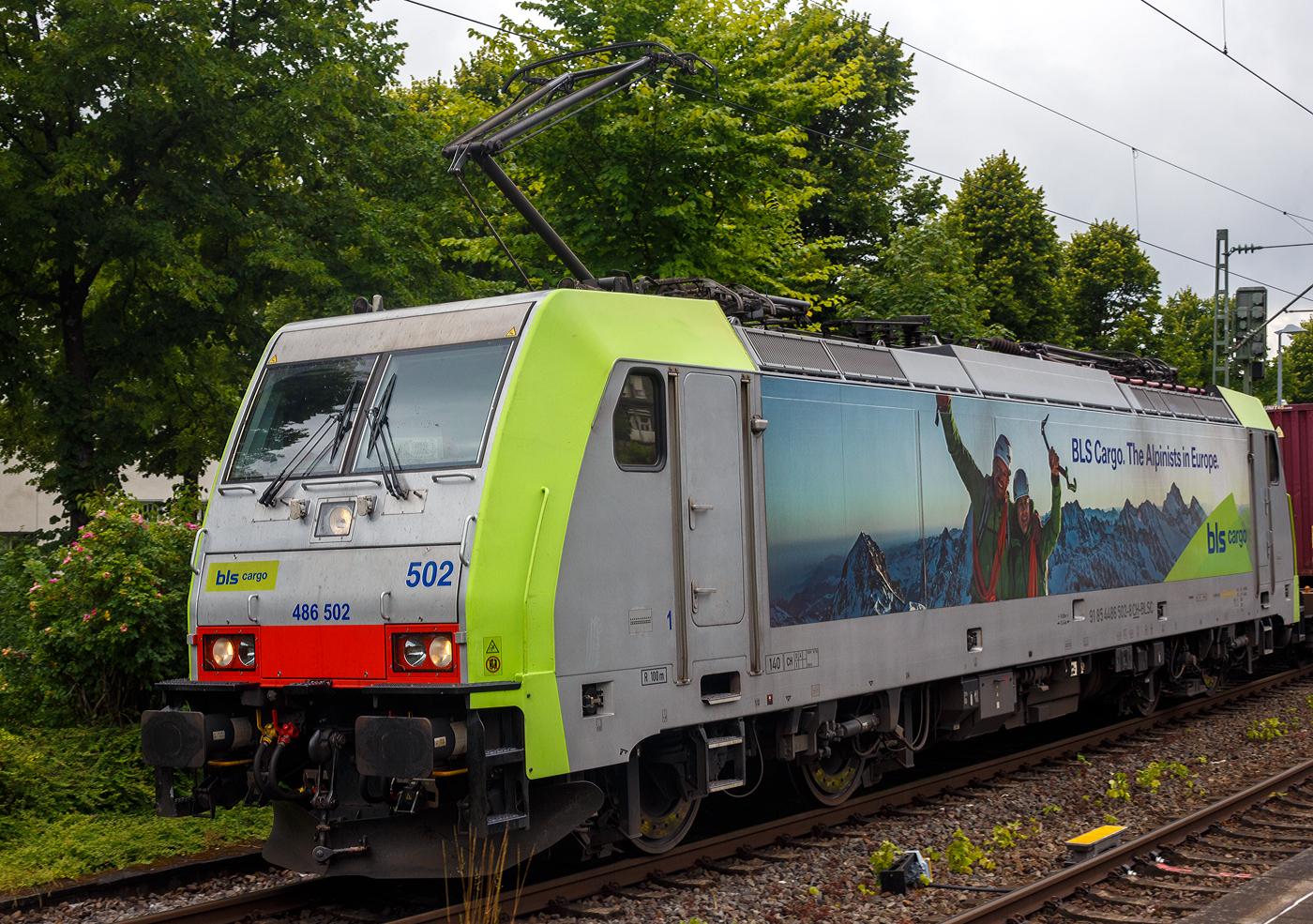 Die BLS Cargo 502, Re 486 502-8/E 486 502 SF  The Alpinists in Europa  (91 85 4486 502-8CH-BLSC) f�hrt am 07 Juli 2025 mit einem HUPAC KLV-Zug durch Kirchen (Sieg) in Richtung K�ln.

Nochmals einen lieben Gru� an den netten Lokf�hrer zur�ck.

Die TRAXX F140 MS wurde 2008 von Bombardier in Kassel unter der Fabriknummer 34401 gebaut und an die BLS Cargo AG (Bern) geliefert. Die Loks sind nur f�r die Schweiz, Deutschland, �sterreich und Italien zugelassen.

Der Erfolg im G�terverkehr veranlasste die BLS zehn weitere TRAXX zu bestellen im Gegensatz zur ersten Serie TRAXX F140 AC1 mit der Bezeichnung Re 485 001 bis 485 020, die nur unter Wechselstrom fahren k�nnen, k�nnen die TRAXX F140 MS Re 486 501 bis 486 510 auch unter 3.000 Volt Gleichstrom eingesetzt werden. Bombardier hatte seit der ersten Lieferung Verbesserungen vorgenommen. Dabei wurde der Lokomotivkasten optimiert und die Traktionsausr�stung mit moderneren Komponenten versehen. Eine Nachbeschaffung w�re noch m�glich gewesen, h�tte aber dazu gef�hrt, dass die Lokomotiven nicht auf dem neuesten Stand waren und nicht unter der Gleichstromfahrleitung eingesetzt werden konnten. Die eingebauten Zugbeeinflussungssysteme erlauben den Einsatz in Deutschland, �sterreich, der Schweiz und Italien (DACHI). Anf�nglich waren die Lokomotiven in der Schweiz nur f�r den Einsatz auf Strecken mit konventioneller Zugbeinflussung und nicht auf ETCS Level 2 Strecken zugelassen. Die Re 486 k�nnen unter sich und mit den Re 485 und Lokomotiven der Baureihe 185/186 in Vielfachsteuerung eingesetzt werden. Mittlerweile nach Umbauten durch die BLS, k�nnen die Loks nun auch mit Re 465, sowie mit Siemens Vectron der BR 193 bzw. Re 475 in Mehrfachtraktion gefahren werden.

TECHNISCHE DATEN:
Spurweite: 1.435 mm (Normalspur)
Achsformel: Bo’Bo’
L�nge �ber Puffer: 18.900 mm
H�he: 4.385 mm
Breite: 2.978 mm
Drehzapfenabstand: 10.400 mm
Achsabstand im Drehgestell: 2.600 mm
Dienstmasse: 85 t
H�chstgeschwindigkeit:  140 km/h
Dauerleistung: 5.600 kW
Dauerzugkraft: 300 kN
Treibraddurchmesser: 1.250 mm
Stromsysteme: 15 kV 16,7 Hz, 25 kV 50 Hz Wechselstrom sowie 3 kV und 1,5 kV Gleichstrom
Antrieb: Tatzlager
