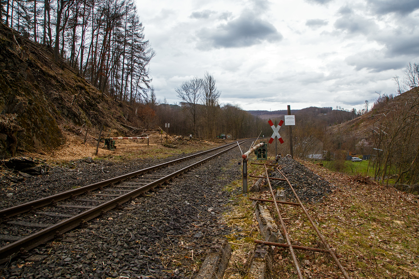 Die Hellertalbahn (KBS 462 / Strecke 2651) bei km 87,8 (bei Herdorf-Sassenroth) am 18.03.2023: Auch wenn hier mindestens bis zum kleinen Fahrplanwechsel im Juni 2023, wegen dem Felsstutz am 23.12.2022, kein Zug zwischen Betzdorf und dem Hp K�nigsstollen (Herdorf) f�hrt, ist und wird die Strecke nun gut freigeschnitten.

Hier die ehemalige Anrufschranke, heute ist der Bahn�bergang st�ndig gelschlossen. Hinten bei km 87,9 gab es fr�her auch eine Anschlussstelle (Anst bzw. Gleisanschluss) zur ehem. Fa. Kr�mer / bzw. zum Hollertszug Herdorf. Hier kann man noch gut Reste davon erkennen. Bis 1987 war der Abschnitt Betzdorf–Herdorf noch zweigleisig. 
