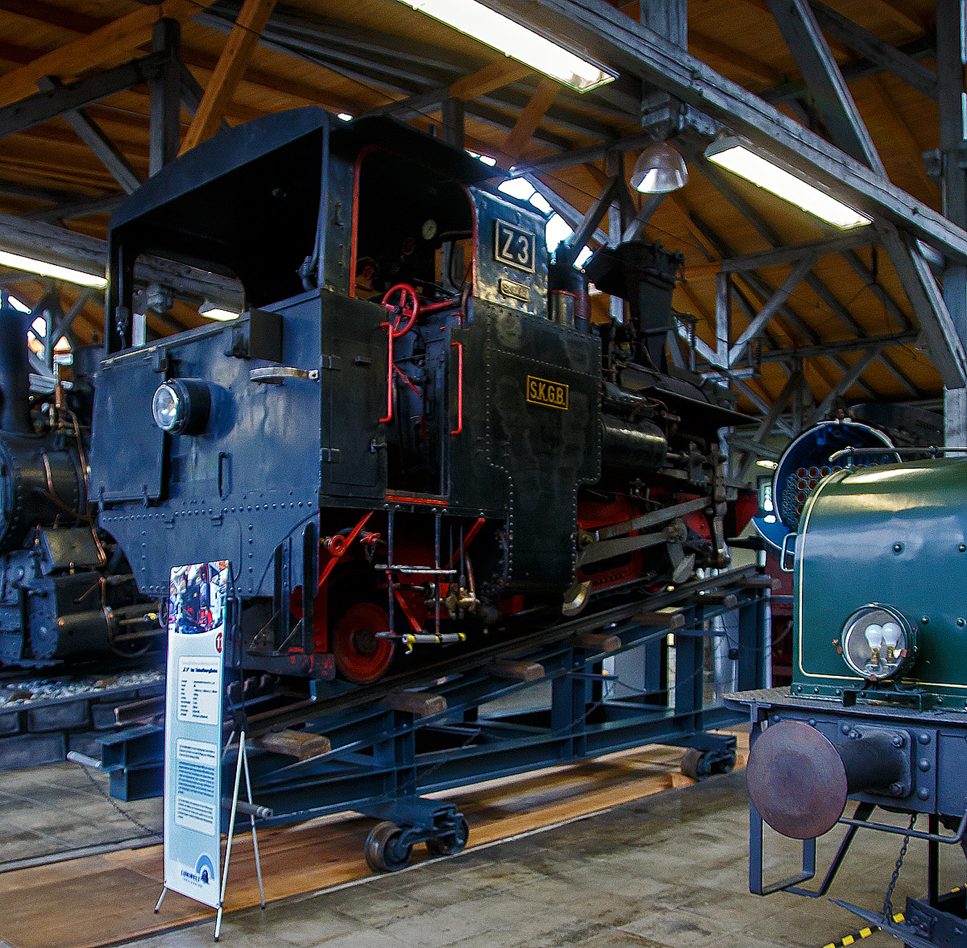 Die kohlegefeuerte Zahnraddampflokomotive SKGLB Z3 „Erika“ der Schafbergbahn, ex SKGB 999.103 „Erika“, ex BB� Z3, ex �BB 999.103 „Erika“ am 11.09.2022 in der Lokwelt Freilassing.

Die Lok wurde 1893 von der Lokomotivfabrik Krauss & Comp. In Linz unter der Fabriknummer 2746 gebaut und an die Salzkammergut-Localbahn-Actiengesellschaft (SKGLB) f�r die Zahnradbahn auf den Schafberg geliefert. Die Lok ist Eigentum der Salzkammergutbahn GmbH und wurde 2007 als Leihgabe in die „Lokwelt Freilassing“ abgegeben.

Die Dampflokomotiven SKGLB Z sind eine Schmalspur-Zahnrad-Tenderlokomotivreihe der Bauart Abt (H 2/3), von denen urspr�nglich sechs Loks Krauss in Linz (abgeleitet der Bauart H 2/3 der Schweizerischen Lokomotiv- und Maschinenfabrik Winterthur) f�r die Schafbergbahn der Salzkammergut-Lokalbahn (SKGLB) gebaut wurden. Eine weitgehend baugleiche Serie von Loks wurde 1896/1900 von der Schneebergbahn-Gesellschaft (SchBB) beschafft. Von den sp�ter zu den �sterreichischen Bundesbahnen geh�renden Lokomotiven sind heute noch vier St�ck betriebsf�hig. Die Maschinen sind aufgrund der Steigung stark geneigt, damit der Kessel w�hrend der Fahrt in der Ebene liegt. Die Kesselneigung ist der einzige nennenswerte Unterschied zwischen den beiden Baureihen und betr�gt bei den am Schafberg eingesetzten Maschinen 170 ‰, bei den Lokomotiven der Schneebergbahn 120 ‰. Die Lokomotiven besitzen einen Au�enrahmen, der im Bereich der Nachlaufachse zu einem Innenrahmen verengt wird.

Der Antrieb erfolgt von einem obenliegenden und relativ kurzhubigen Zylinder (System Brown) �ber einen Balancierhebel und Treibstangen auf die beiden gekuppelten Zahnradachsen. Die Leistung betr�gt ungef�hr 200 PS. Die Steuerung erfolgt �ber eine innenliegende Exzentersteuerung System Gooch. Es werden lediglich die beiden Zahnr�der angetrieben, die R�der sind lediglich lose mitdrehend und dienen ausschlie�lich der F�hrung im Gleis. Deshalb m�ssen auch die ebenen Streckenabschnitte mit Zahnstangen ausger�stet sein.

Die Lokomotiven werden mit Kohle gefeuert. 1954/55 erhielten die Maschinen einen Giesl-Ejektor mit Mikrofunkenf�nger. Der Wasserkasten fasst 1,2 m�. Zus�tzlich werden ca. 300 Liter zur K�hlung der Zylinder bei der Talfahrt mitgef�hrt.

Gebremst wird �ber eine Gegendruckbremse Bauart Riggenbach sowie eine Rillen-Bandbremse. In den 1960er Jahren wurden die Lokomotiven mit einer bei �berschreitung der H�chstgeschwindigkeit automatisch ausl�senden Notbremse in Form einer als Bandbremse ausgef�hrten Druckluftbremse ausger�stet. Da jedoch auf den kleinen Lokomotiven kein Platz f�r einen Druckluftpumpe und einen Luftbeh�lter war, wurden Druckluftflaschen an den F�hrerhaus-R�ckw�nden montiert.

TECHNISCHE DATEN:
Gebaute Anzahl: 6 (Schafbergbahn) / 5 (Schneebergbahn)
Hersteller:  Krauss & Comp./Linz
Baujahre: 1893, 1896–1900
Spurweite:  1.000 mm (Meterspur)
Achsformel: 2zz1'  n2t
L�nge �ber Puffer:  4.545 mm
H�he: 3.300 m
Eigengewicht: 14,5 t
H�chstgeschwindigkeit: 12 km/h
Zahnrad-Teilkreis-� (Treibrad): 573 mm
Laufraddurchmesser vorn: 706 mm
Laufraddurchmesser hinten: 520 mm
Zahnradsystem:  Abt
Steuerungsart: Exzentersteuerung
Zylinder: 2 x � 320 mm x 600 mm Hub
Kessel�berdruck: 14,0 bar
Leistung (ca.): 150 kW (200 PS)
Anzahl der Heizrohre: 150
Heizrohrl�nge: 2.000 mm
Rostfl�che: 0,9 m�
Wasservorrat: 1,2 m�
Kohlevorrat: 0,6 t
Lokbremse: Rillenband-, Riggenbach-Gegendruckbremse
Max. Steigung: 255‰ (Schafbergbahn), 197‰ (Schneebergbahn)
Besonderheiten:  Giesl-Ejektor

Die Schafbergbahn ist eine meterspurige reine Zahnradbahn (System Abt) in �sterreich. Sie verkehrt zwischen St. Wolfgang am Wolfgangsee  (542 m �.M.) und dem Schafberg (1.782 m �.M.). Die Talstation liegt in Ober�sterreich, die Bergstation im Bundesland Salzburg. Die Bahn ist mit einer Zahnstange nach System Abt ausgestattet und �berwindet bei einer maximalen Steigung von 255 ‰ einen H�henunterschied von 1.190 Metern. Der Antrieb erfolgt ausschlie�lich durch die Zahnr�der, daher sind auch waagrechte und wenig geneigte Gleise mit einer Zahnstange ausger�stet. Die Strecke ist nicht elektrifiziert und wird von Dampf- und Dieselloks befahren. Von den historischen Originalmaschinen der Type SKGLB Z (Baujahre 1893/1894) sind noch drei Exemplare, bei der Schafbergbahn vorhanden, diese kommen im Zuge eines eigenen Nostalgiefahrplanes zum Einsatz. Mit ihnen betr�gt die Fahrzeit zum Gipfel eine Stunde statt 35 Minuten.

Die Schafbergbahn wurde 1932 an das �sterreichische Verkehrsb�ro verkauft. 1938 ging sie an die Deutsche Reichsbahn und somit nach dem Zweiten Weltkrieg an die �BB �ber. Seit 2006 betreibt die Salzkammergutbahn GmbH (SKGB), eine Tochterfirma der Salzburg AG, die Schafbergbahn und die Wolfgangseeschifffahrt.
