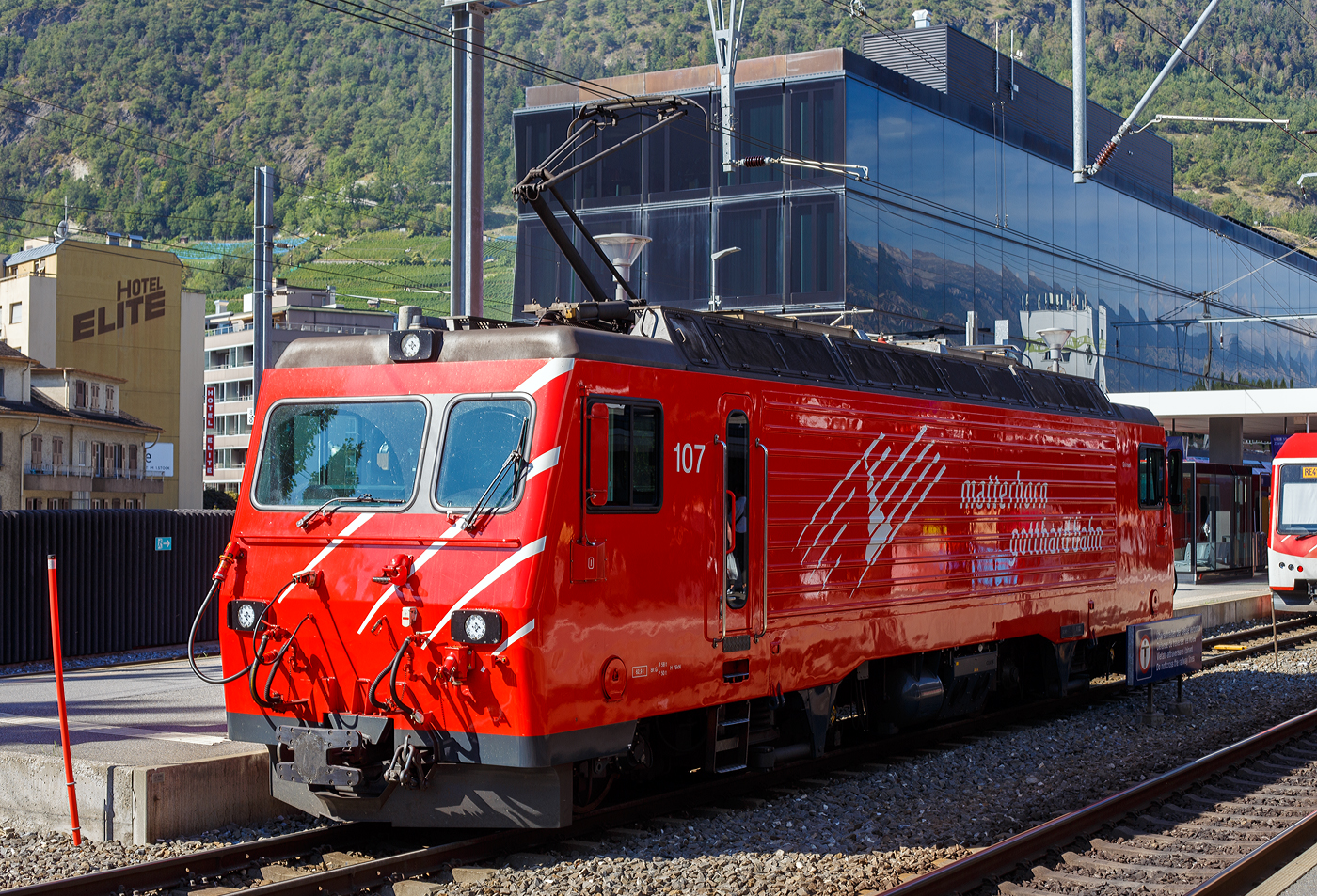 Die MGB HGe 4/4 II 107 „Grimsel“ erreicht am 11 September 2022 als Lz (solo) den Bahnhof Visp.

Die HGe 4/4 II 103 „Grimsel“ wurde 1990von der SLM (Schweizerische Lokomotiv- und Maschinenfabrik) in Winterthur unter der Fabriknummer 5393 gebaut und an die FO (Furka-Oberalp-Bahn) geliefert. Der elektrische Teil ist von BBC. 

Die HGe 4/4 II ist eine schmalspurige (1.000 mm) gemischte Zahnrad- und Adhäsions-Lokomotive. Eine erste Serie von fünf Lokomotiven wurde gemeinsam von der Furka-Oberalp-Bahn (FO) sowie von der SBB für die Brünigbahn, die heute zur Zentralbahn (zb) gehört, beschafft. Da sich dieser Lokomotivtyp bewährte, wurden weitere elf Lokomotiven bestellt, und schließlich gab auch noch die Brig-Visp-Zermatt-Bahn (BVZ) fünf Loks in Auftrag.

Die HGe 4/4 II bespannt vor allem schwere Personenzüge, zum Teil im Pendelzugbetrieb. Bei der Zentralbahn bespannte sie bis 2012 alle Schnellzüge von Meiringen nach Luzern, bei der Matterhorn Gotthard Bahn die Züge des Glacier-Express. Weiter führen die Loks Pendelzüge Brig–Visp–Zermatt und seit der Eröffnung des Tunnels nach Engelberg Pendelzüge Luzern–Engelberg. Außerdem werden aushilfsweise Autopendelzüge durch den Furkatunnel geführt. Schließlich gehören neben weiteren Personenzügen auch diverse Güterzüge Visp–Zermatt sowie bis 2013 Disentis–Sedrun (NEAT-Baustelle) zum Aufgabengebiet.

Konstruktion:
Der Lokomotivkasten ist ein Stahlblechkasten mit gesickten Seitenwänden. Die asymmetrische Frontscheibe aus beheizbarem Verbundglas verbessert die Sicht für den Lokomotivführer. Die drei Dachelemente sind aus Aluminium. Die Pufferkräfte werden über Verstrebungen auf den ganzen Kasten übertragen, weshalb auf seitliche Maschinenraumöffnungen verzichtet werden musste. Der gesamte Kasten hat ein Gesamtgewicht von nur 5,9 Tonnen. Er kann ohne bleibende Deformation eine zentrale Druckkraft von 1000 kN aufnehmen.

Die Drehgestelle sind als geschweißte Hohlträgerkonstruktion mit zwei Längsträgern und einem kräftigen mittleren Querträger sowie zwei Kopftraversen ausgeführt. Sie haben einen Achsstand von 2980 mm, und die Flexicoil-Federn stützen den Kasten auf die seitlich an die Längsträger angeschweißten Federwannen. Die Zug- und Druckkräfte werden durch seitlich angeordnete Stangen mit Sphärolastiklagern übertragen. Wegen des kurzen Achsstands sind die Fahrmotoren oberhalb des Drehgestellrahmens angebracht.
Für den Antrieb wurde erstmals der Differentialantrieb eingebaut, der es ermöglicht, im Zahnstangenbetrieb auch einen Anteil der Zugkraft über den Adhäsionsantrieb aufzubringen. Dies setzt wiederum eine Schlupfbegrenzung im Differentialgetriebe voraus, um ein Schleudern oder Gleiten der Räder zu verhindern. Da die zweilamellige Abtzahnstange (System Abt) der FO nicht die gesamte Zugkraft aufnehmen kann, ist die Mithilfe des Adhäsionsantriebs notwendig; dieser übernimmt einen Drittel der Zugkraft. Hätte sich der Antrieb nicht bewährt, wäre es zumindest am Brünig mit der Riggenbachzahnstange möglich gewesen, auf einen abkuppelbaren Adhäsionsantrieb zu wechseln. Dies war aber nicht notwendig, da das Differentialgetriebe zur vollen Zufriedenheit funktionierte.

Bremssysteme:
Dank der elektrischen Rekuperationsbremse ist eine gleichmäßige Beharrungsbremse bei der Talfahrt möglich.
Daneben ist eine normale automatische Druckluftbremse eingebaut, welche auch als Bremssystem I bezeichnet und im Regelbetrieb zum Halten des Zuges verwendet wird. Sie ist als Klotzbremse ausgeführt.
Weiterhin ist noch das Bremssystem II installiert, welches für Zahnradbahnen vorgeschrieben ist und es ermöglichen soll, den Zug nur mit Hilfe der Lokomotive im Zahnstangenabschnitt zum Halten zu bringen, wenn das erste Bremssystem ausfallen sollte. Dieses ist als federspeichergestütztes Bandbremssystem ausgelegt, welches direkt auf das Zahnrad wirkt. Bei Einsatz dieser Bremse treten enorme Kräfte auf, welche nur unter Kontrolle sind, wenn die Anhängelast bei der Talfahrt nicht zu groß ist.
Schließlich ist eine direkt wirkende Rangierbremse vorhanden, die sich der Bremsklötze des Bremssystems I bedient.
Die Lokomotive hat keine Handbremse, sondern wird mit Federspeicherbremsen gesichert.

TECHNISCHE DATEN der HGe 4/4 II der FO und BVZ (heute MGB), 
die Daten der  zb (Zentralbahn), ex SBB Brünigbahn weichen ab:
Spurweite: 1.000 mm
Achsformel: Bo'Bo'
Dienstgewicht: 64 t 
Achslast: 16 t
Länge über Puffer: 14'.776 mm 
Höchstgeschwindigkeit Adhäsion: 100 km/h
Höchstgeschwindigkeit Zahnrad: 40 km/h
Stromsystem: 11 kV 16.7 Hz
Anzahl der Motoren: 4
Adhäsions-Antrieb: Gelenkwelle
Antrieb Zahnrad: Differentialantrieb
Zahnradsystem: 	Abt (zweilamellig)
Stundenleistung: 1.932 kW
Dauerleistung: 1.875 kW
Anfahrzugkraft: 230 kN (Adhäsion) / 280 kN (Zahnrad)
Anzahl Bremssysteme: 4
Bremsen: Rekuperation, Klotz, Federspeicher, Bandbremse
Anhängelast: 130 t (125 ‰)
