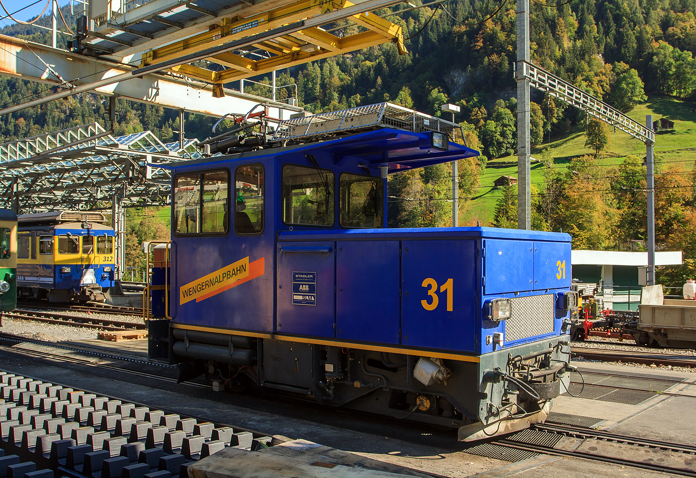 Die moderne elektrische Zahnradlokomotive WAB He 2/2 – 31am 02.10.2011 abgestellt im Bahnhof Lauterbrunnen.

Die Gleichstrom-Elektro-Zahnradlokomotive wurde 1995 von Stadler Rail AG / SLM gebaut, der elektrische Teil ist von ABB.

Die WAB He 2/2 31–32 sind zwei elektrische Zahnradlokomotiven der schweizerischen Wengernalpbahn, kurz WAB. Ursprünglich war geplant, diese im Jahre 1995 beschafften Lokomotiven, als endgültigen Ersatz für die letzten sich im Einsatz befindenden He 2/2 51–65 aus den Jahren 1909 bis 1929 zu verwenden, mit Stand 2020 sind aber einzelne dieser zwischenzeitlich über 100-jährigen Lokomotiven immer noch täglich im Rangierdienst im Bahnhof Lauterbrunnen im Einsatz.

Die He 2/2 31–32 besitzen einen geschweißten Stahlrahmen, welcher in marineblau angestrichen ist. Der Führerstand ist geschlossen und hat eine Stirnwandtür zur talseitigen Rangierplattform. Beide Loks haben in beide Fahrtrichtungen Führertische, können aber auch funkferngesteuert werden. Die 5,75 m langen und 16,0 t schweren Loks haben die Achsformel 2zz. Auf beiden Laufachsen befindet sich ein angetriebenes Zahnrad. Die Lokomotiven haben eine Rekuperationsbremse. Da sie 22 km/h Höchstgeschwindigkeit bewältigen können, können sie mit allen Triebwagen mithalten und somit auch während des laufenden Hochbetriebes verkehren. Als Triebmotoren haben sie Drehstrommotoren und erreichen eine Stundenleistung von 460 kW. Es sind die ersten Zahnradfahrzeuge mit Drehstrom-Umrichterantrieb.

Die He 2/2 31 und 32 sind in Lauterbrunnen stationiert und kommen hauptsächlich auf dem Streckenabschnitt Lauterbrunnen–Wengen zum Einsatz. Vornehmlich verkehren die Lokomotiven mit Güter-, Arbeits-, Bau- und Schneeräumzügen. Bei Bedarf auch mit Personenwagen, um so größere Fahrgastanstürme bewältigen zu können.

TECHNISCH DATEN:
Baujahre: 1995
Hersteller:  Stadler Rail, SLM, ABB
Nummerierung: 31 und 32
Achsfolge:  2zz
Spurweite: 800 mm
Zahnradsystem:  Riggenbach-Pauli
Länge über Puffer : 5.750 mm
Höhe: 3.730 mm
Breite: 2.200 mm
Achsstand: 3.250 mm
Zahnradteilkreis-Ø: 637 mm
Laufraddurchmesser: 728 mm (neu)
Dienstgewicht: 16 t
Leistung: 460 kW
Stundenzugkraft: 120 kN
Zul. Höchstgeschwindigkeit: 22 km/h (Bergfahrt) / 14 km/h (Talfahrt)
Übersetzung:  1:15,65
Stromsystem: 1.500 V DC
Anzahl der Fahrmotoren: 2
Max. Neigung : 250 ‰