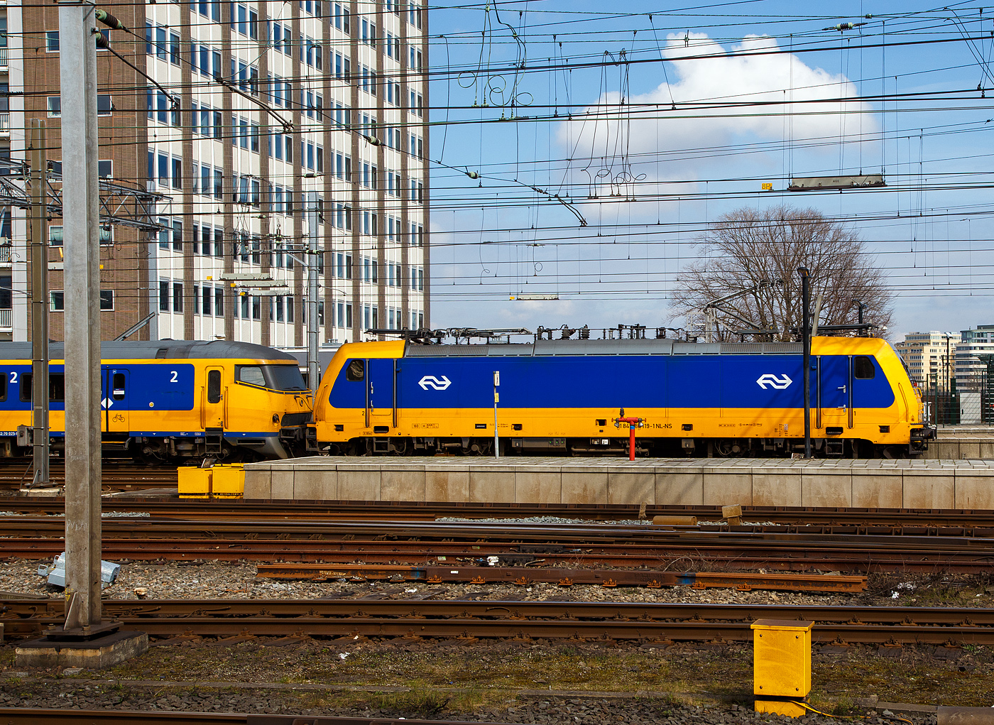 Die NS 186 119 (91 84 1186 119-1 NL-NS) erreicht am 31 M�rz 2018 mit einem IC (InterCity) den Bahnhof Amsterdam Centraal. Am Zugschluss war noch eine weitere 186er. 

Die Bombardier TRAXX F140 MS wurde 2007 von Bombardier in Kassel unter der Fabriknummer 34323 gebaut und an die ATC - Angel Trains Cargo, seit 2008 war sie dann an die NS Hispeed bzw. NS - Nederlandse Spoorwegen N.V. vermietet. Sie hat die Zulassungen f�r Deutschland, �sterreich, Belgien und die Niederlande. Aktuell (seit 2024) ist die Lok an die SNCB - Soci�t� Nationale des Chemins de Fer Belges als 2869 vermietet und tr�gt die UiC Nummer 91 84 1186 119-1 NL-B. 

Die NS-Baureihe 186 wurden von Bombardier Transportation zwischen 2006 und 2014 gebaut. Die Lokomotiven werden zum Ziehen von Personenz�gen verwendet, fr�her f�r NS Hispeed und jetzt f�r NS International. Sie sind eine Multi-Systems-Variante des TRAXX, einer Vierfach-Spannungslokomotive, die auf den meisten europ�ischen Elektrifizierungssystemen arbeiten kann: 1,5/3,0 kV DC und 15/25 kV AC.

Die BR besteht aus zwei Chargen, die erste im Jahr 2008 eingef�hrte Bauloks. Die zweite Charge wurde 2014 eingef�hrt. Die ersten 12 Lokomotiven wurden 2005 von der Hochgeschwindigkeitsallianz (HSA) bei Alpha Trains bestellt. Die Bombardier Transportation in Kassel baute und �ber Alpha Trains angemietet wurden. Diese kamen ab 2008/2009 auf den Verbindungen der HSL-Zuid zwischen Amsterdam und Breda zu Einsatz. Diese Z�ge haben eine H�chstgeschwindigkeit von 160 km/h. Diese Lokomotiven mit den Z�gen sollte nur eine tempor�re Ma�nahme sein, bis die Hochgeschwindigkeitstriebz�ge Fyra V250 (AnsaldoBreda V250) in Betrieb genommen wurden. Die V250 traten 2012 in Dienst, wurde aber Anfang 2013, wegen zahlreicher M�ngel, au�er Betrieb genommen und an den Hersteller zur�ckgegeben. Die italienische Trenitalia kaufte 2017 17 von den 19 Einheiten, die dort nun als ETR 700 im Einsatz sind. 

Aus diesem Grund waren die NS TRAXX-Lokomotiven noch bis 2024 im Einsatz.
