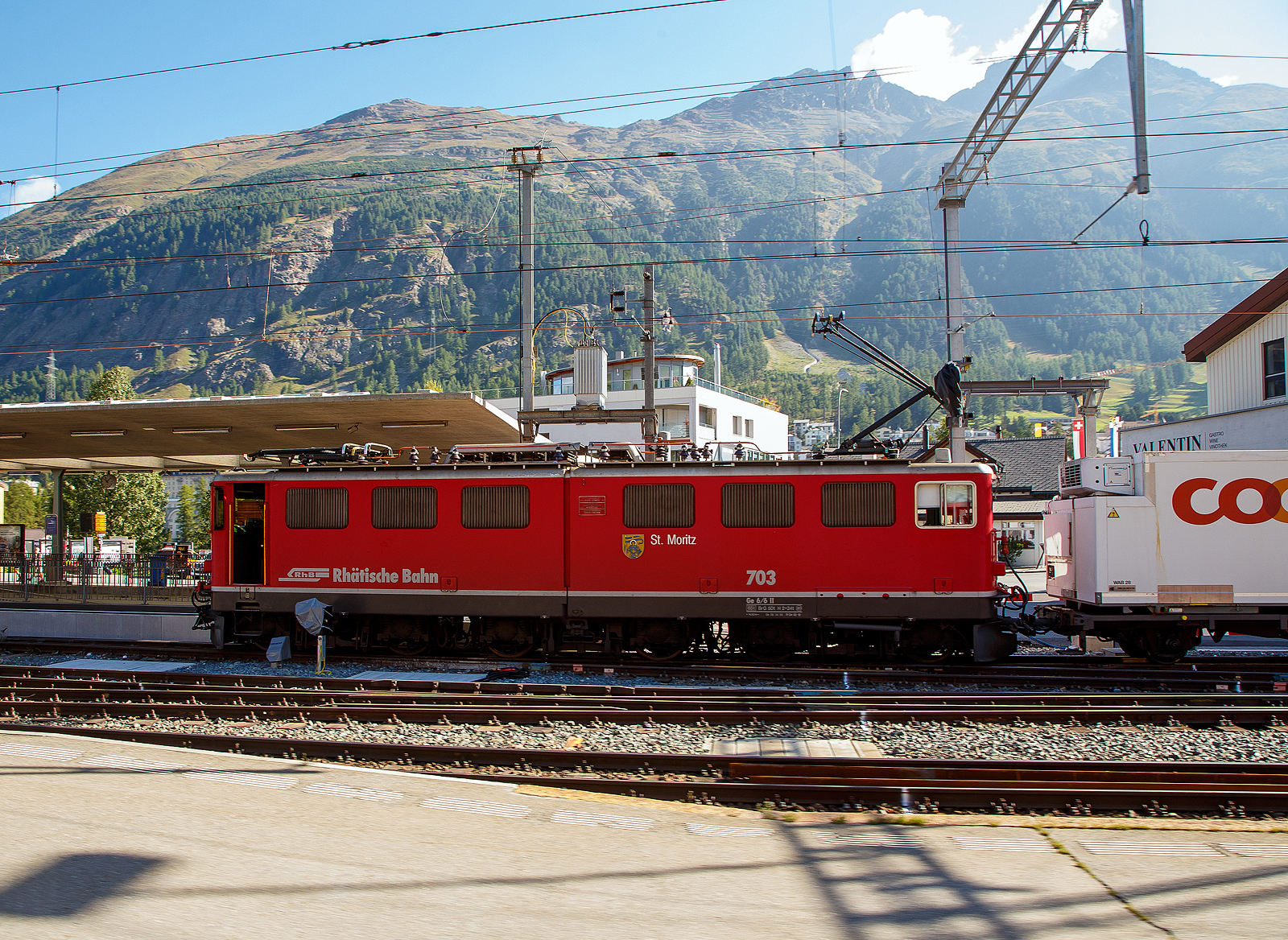 Die RhB Ge 6/6 II - 703 „St. Moritz“ steht am 06.09.2021 mit einem G�terzug im Bahnhof Samedan. Leider ist die RhB Ge 6/6 II – 703 auch schon Geschichte, sie wurde am 14. Juni 2022 in Chur abgebrochen (verschrottet). Auch zwei weitere (701 und 704) wurden bereits abgebrochen, die anderen vier Loks sind ausrangiert und wurden abgestellt. Nur die 707 „Scuol“ ist als historische Lok vorgesehen und z.Z. in Samedan abgestellt.

Die Ge 6/6 II ist/war eine schwere Elektrolokomotive der Rh�tischen Bahn (RhB). Die sechsachsigen Maschinen (Achsformel Bo'Bo'Bo') wurden meistens im G�terzugdienst eingesetzt.

Zur Verst�rkung des Lokomotivparks bestellte die RhB Mitte der 50er Jahre des vergangenen Jahrhunderts bei der schweizerischen Industrie eine leistungsstarke sechsachsige Gelenklokomotive. Zahlreiche Komponenten dieser Fahrzeuge mit geteiltem Lokomotivkasten wurden von der Ge 4/4 I �bernommen. Mitte 1958 erfolgte die Auslieferung der ersten beiden Prototypen. Die folgende Serie von f�nf weiteren Fahrzeugen wurde 1965, mit leicht ge�nderter Front ohne �bergangst�r, ausgef�hrt. Diese wurde bei den beiden Prototypen 1968/69 zugeschwei�t. Ein Umbau der Front entsprechend der Serie 703 - 707 erfolgte jedoch erst Ende der 80er Jahre. Ab 1985 wurden die ersten Maschinen umlackiert und trugen seitdem eine rote Lackierung. 1998 erfolgte, wie zuvor schon bei den Ge 4/4 I, ein Austausch der Scherenstromabnehmer durch moderne Einholmstromabnehmer.

�ber weite Jahre wurden diese Fahrzeuge haupts�chlich vor den Schnellz�gen zwischen Chur und St. Moritz eingesetzt. Diese Aufgabe haben inzwischen die modernen Umrichterlokomotiven Ge 4/4 III �bernommen. So sieht man sie heute meistens im G�terzugdienst.

Technisch entsprechen die Maschinen dem damaligen Stand: (Niederspannungs-) Stufenschalter und Einphasen-Reihenschlussmotoren. Die �u�eren beiden Drehgestelle und die Fahrmotoren k�nnen mit den Ge 4/4 I ausgetauscht werden. Das Kastengelenk zwischen den beiden Lokh�lften erlaubt nur vertikale Bewegungen. 

TECHNISCHE DATEN:
Bezeichnung: Ge 6/6 II
Betriebsnummern: 701 – 707
Anzahl Fahrzeuge: 7
Baujahre: 1958 (701 und 702), 1965 (703 bis 707)
Hersteller Kasten und Drehgestelle: SLM
Hersteller Elektrik: BBC, MFO

Spurweite: 1.000 mm
Achsanordnung: Bo'Bo'Bo'
L�nge �ber Puffer: 14.500 mm
Breite: 2.650 mm
Drehzapfenabstand: 8.600 mm (Der �u�eren Drehgestelle)
Gesamtradstand: 11.100 mm
Achsabstand im Drehgestell: 2.500 mm
Triebraddurchmesser (neu): 1.070 mm
Dienstgewicht:65,0 t
H�chstgeschwindigkeit: 80 km/h
Anh�ngelast: bei 45 ‰ 205 t / bei 35 ‰ 280 t
Fahrleitungsspannung: 11 kV, AC 16,7 Hz
Anzahl Fahrmotoren: 6 St�ck (Typ 8SW570)
Max. Leistung am Rad: 1.776 kW (2.414 PS)
Max. Zugkraft am Rad: 213,9 kN
Dauerzugkraft am Rad: 135,4 kN
Getriebe�bersetzung: 1 : 5,437
