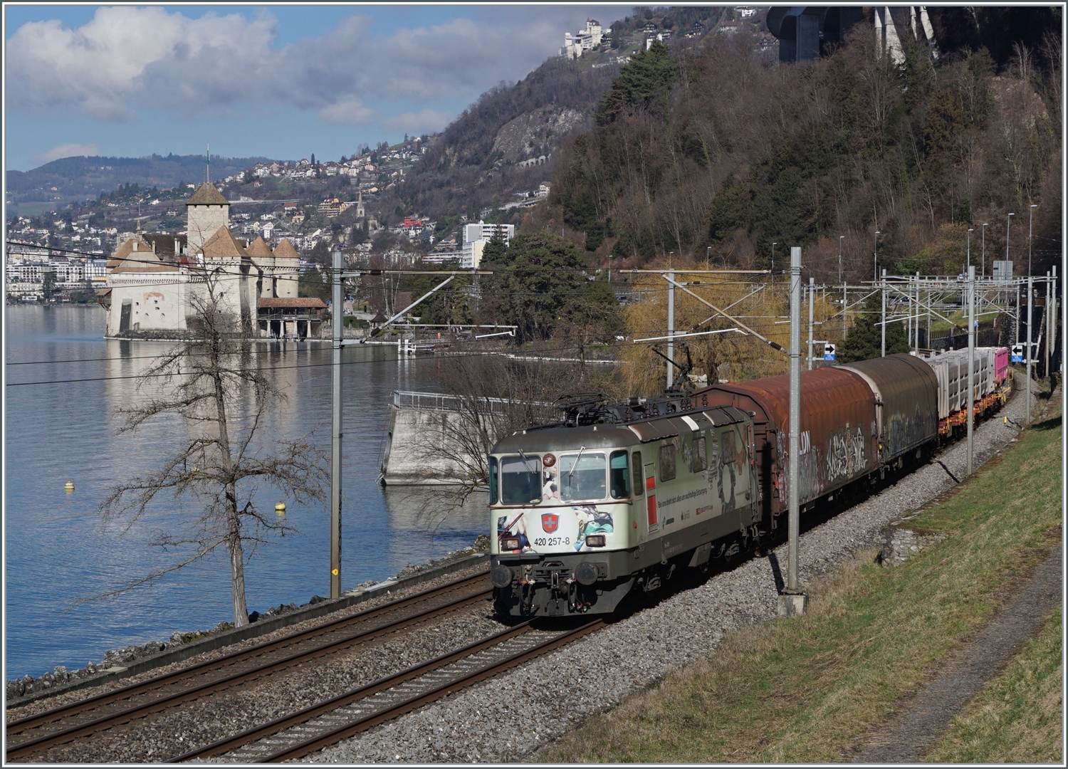 Die SBB Re 4/4 II 11275 (Re 420 257-8) mit einem Werbeanstrich ist mit einem Güterzug Richtung Wallis kurz vor Villeneuve unterwegs. Im Hintergrund das Château de Chillon.

13. Februar 2024