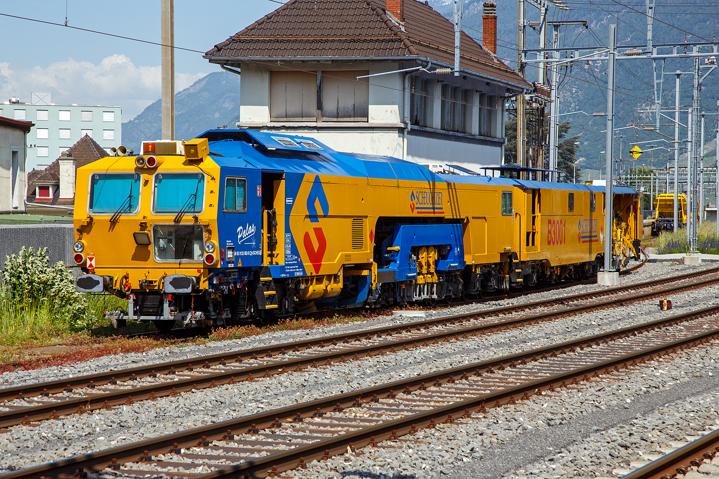 Die SCHEUCHZER B 3001 Hochleistungsstopfmaschine (Dreikopf) mit integriertem Gleisstabilisator, Flankenverdichtung und Kehranh�nger, 99 85 9123 002-9 CH-SCHEU (ex VTmaas 80 81 00 03 198-8), ein Plasser & Theurer Dynamic Stopfexpress 09-3X mit Kehranh�nger der Scheuchzer SA, ist am 26. Mai 2023 beim Bahnhof Martigny abgestellt.

Die Dynamic 09-3X sind kontinuierlich arbeitende Nivellier-, Hebe-, Richt- und Drei-Schwellen-Stopfmaschinen mit integrierter dynamischer Gleisstabilisation. Sie erm�glichen das Stopfen von drei Schwellen in einem Arbeitsgang. Dadurch wird eine hohe Arbeitsgeschwindigkeit erzielt. Diese Maschinen sind jedoch nicht f�r den Bereich von Weichen geeignet. Bei der Stopfung wird der Schotter unter der Schwelle verdichtet, wodurch ein stabiles Schwellenauflager entsteht. Diese Maschine ist zudem mit Kehranh�nger, zur Reinigung der Schwellenoberfl�che, ausgestattet.

TECHNISCHE DATEN:
Spurweite: 1.435 mm
Achsanzahl: 11
Achsfolge Fahrantrieb (Hydrodyn.): Bo´2´2´+ Bo´2´+1´ (4 Achsen angetr.)
Achsfolge  Arbeitsantrieb (Hydrodyn.): Bo´ Bo´2´+ Bo´ Bo´+1´ (8 Achsen angetr.)
L�nge �ber Puffer: 49.740 mm
Drehzapfenabstand: 12.545 / 3.265 / 5.000 / 11.800 / 9.000 mm
Gesamtgewicht: 167 t
Achslast: 20 t
H�chstgeschwindigkeit (eigen/geschleppt):100 km/h 
Motorleistung: 440 kW und 370 kW (Deutz Dieselmotoren mit Partikelfilter)
Kleinster befahrbarer Gleisbogen: R 120 m
Bremse: KE-GP (K)
Bremssohlen: J 838
Bremsgewichte: G = 100 t / P = 112 t
Tankvolumen (Diesel): 4.000 l
Tankvolumen (Hydraulik�l): 1.300 und 800 l
Tankvolumen (Wasser): 3.900 l (f�r Staubniederbek�mpfungsanlage)

Quelle: Scheuchzer SA
