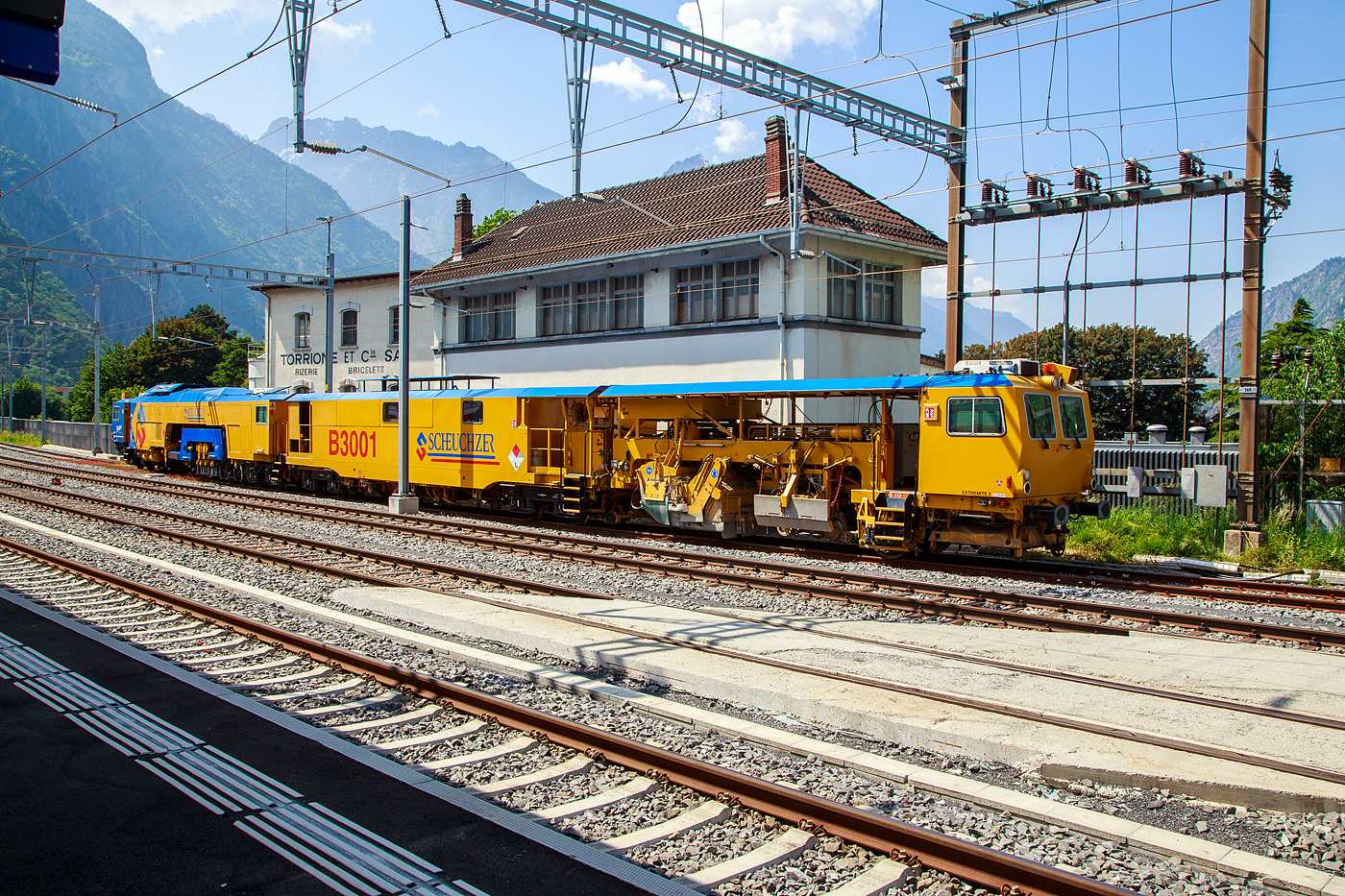 Die SCHEUCHZER B 3001 Hochleistungsstopfmaschine (Dreikopf) mit integriertem Gleisstabilisator, Flankenverdichtung und Kehranh�nger, 99 85 9123 002-9 CH-SCHEU (ex VTmaas 80 81 00 03 198-8), ein Plasser & Theurer Dynamic Stopfexpress 09-3X mit Kehranh�nger der Scheuchzer SA, ist am 26. Mai 2023 beim Bahnhof Martigny abgestellt.

Die Dynamic 09-3X sind kontinuierlich arbeitende Nivellier-, Hebe-, Richt- und Drei-Schwellen-Stopfmaschinen mit integrierter dynamischer Gleisstabilisation. Sie erm�glichen das Stopfen von drei Schwellen in einem Arbeitsgang. Dadurch wird eine hohe Arbeitsgeschwindigkeit erzielt. Diese Maschinen sind jedoch nicht f�r den Bereich von Weichen geeignet. Bei der Stopfung wird der Schotter unter der Schwelle verdichtet, wodurch ein stabiles Schwellenauflager entsteht. Diese Maschine ist zudem mit Kehranh�nger, zur Reinigung der Schwellenoberfl�che, ausgestattet.

TECHNISCHE DATEN:
Spurweite: 1.435 mm
Achsanzahl: 11
Achsfolge Fahrantrieb (Hydrodyn.): Bo´2´2´+ Bo´2´+1´ (4 Achsen angetr.)
Achsfolge  Arbeitsantrieb (Hydrodyn.): Bo´ Bo´2´+ Bo´ Bo´+1´ (8 Achsen angetr.)
L�nge �ber Puffer: 49.740 mm
Drehzapfenabstand: 12.545 / 3.265 / 5.000 / 11.800 / 9.000 mm
Gesamtgewicht: 167 t
Achslast: 20 t
H�chstgeschwindigkeit (eigen/geschleppt):100 km/h 
Motorleistung: 440 kW und 370 kW (Deutz Dieselmotoren mit Partikelfilter)
Kleinster befahrbarer Gleisbogen: R 120 m
Bremse: KE-GP (K)
Bremssohlen: J 838
Bremsgewichte: G = 100 t / P = 112 t
Tankvolumen (Diesel): 4.000 l
Tankvolumen (Hydraulik�l): 1.300 und 800 l
Tankvolumen (Wasser): 3.900 l (f�r Staubniederbek�mpfungsanlage)

Quelle: Scheuchzer SA
