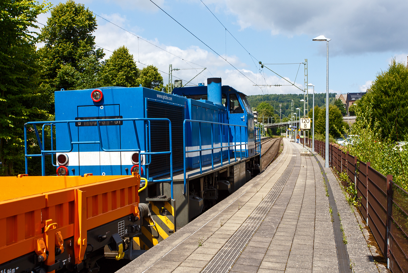 Die SPITZKE G 1206-SR-01 / 275 846-4 (92 80 1275 846-4 D-SLG) der SPITZKE SE (Großbeeren), ex XR 01 der SPITZKE RIEBEL GLEISLOGISTIK, ex V 200 001 der Xaver Riebel Gleisbau, fährt am 17 Juli 2025, mit einem Flachwagen-Güterzug (vierachsige Flachwagen mit Stahlfußboden, Seiten- und Stirnwänden der Gattung Res), durch Kirchen (Sieg) in Richtung Siegen.

Die MaK G 1206 wurde 2003 von Vossloh unter der Fabriknummer 1001382 gebaut und an die Xaver Riebel Gleisbau als V 200 001 geliefert.
Lebenslauf
18.03.2003 Auslieferung an Xaver Riebel Gleisbau GmbH & Co. KG, Buchloe  V 200 001  
09.12.2008 SRG - SPITZKE RIEBEL GLEISLOGISTIK GmbH, Buchloe  XR 01  (NVR-Nummer: 92 80 1275 846-4 D-XR)
Ab 01.07.2015 SPITZKE SE, Großbeeren  XR 01 (92 80 1275 846-4 D-SLG), später Umzeichnung in  G 1206-SR-01   

Die MaK G 1206 ist im schweren Rangier- und Streckendienst einsetzbar. Sie wurde 1997 zum ersten Mal gebaut und ist nach Deutschland, Österreich, der Schweiz, Luxemburg, Italien, Spanien, den Niederlanden und nach Frankreich verkauft worden. Allein 23 Lokomotiven fahren als BB 61000 bei der SNCF, davon sechs mit MTU-Motor (Die G 1206 gibt es wahlweise mit Caterpillar- oder MTU-Motor). Eine Weiterentwicklung der MaK 1206 ist die Vossloh G 1700 BB. 

Im Zuge der fortschreitenden Liberalisierung des Schienenverkehrs in Deutschland zeichnete sich Ende der 1990er Jahre ein zunehmender Bedarf an streckentauglichen Diesellokomotiven. Bei zahlreichen Bahnen bestanden damals Überlegungen, Verkehrsleistungen über das eigene Netz hinaus auf Gleisen der DB AG eigenständig zu erbringen, was in den folgenden Jahren auch vielfältig realisiert wurde.

Mit der G 1206 stand zwar im Prinzip schon eine für diese Einsätze geeignete Maschine zur Verfügung, jedoch gab es an der Maschine noch Verbesserungspotential, das nun genutzt wurde. Inzwischen standen in der benötigten Leistungsklasse neu entwickelten Motoren zur Verfügung, die mit 12 statt 16 Zylindern auskommen. Statt des in den Lokomotiven für die Dortmunder Eisenbahn verwendeten neuen MTU-Motors entschied man sich für die kommende Serienproduktion aber für einen technisch ähnlichen Motor von Caterpillar, den 3512B. Im Zuge der Anpassung der Lok an diesen Motor erhielt sie geringfügig breitere Motor- und höhere Getriebehauben, wodurch sich diese Loks schon äußerlich von ihren Vorgängern unterscheiden.

Ebenfalls überarbeitet wurde das Fahrwerk. Hier kamen weiterentwickelte Drehgestelle mit Lenkerführung für eine Höchstgeschwindigkeit von 100 km/h zum Einsatz. Die Radsätze werden bei diesen Drehgestellen nicht mehr von einer Gleitplattenführung sondern von verschleißfreien Lenkern geführt. Damit konnte nicht nur das Laufverhalten verbessert und damit die Höchstgeschwindigkeit gesteigert, sondern auch die Führung von Drehgestell und Radsatz weitgehend verschleißfrei ausgeführt werden. Für den Antrieb wurden nicht mehr die Radsatzgetriebe aus eigener Fertigung verwendet, sondern welche von ZF mit einer für die Höchstgeschwindigkeit besser geeigneten Übersetzung.

TECHNISCHE DATEN der G 1206:
Spurweite: 1.435 mm (Normalspur)
Antriebart: dieselhydraulisch
Achsfolge: B'B' 
Länge über Puffer: 14.700 mm
Drehzapfenabstand: 7.200 mm
Achsabstand im Drehgestell: 2.400 mm
größte Breite: 3.080 mm
Höhe über Schienenoberkante: 4.220 mm
Raddurchmesser neu: 1.000 mm
Motor: Caterpillar 12 Zylinder 4-Takt Dieselmotor mit Abgasturbolader und Ladeluftkühlung vom Typ 3512B DI TA-SC
Leistung: 1.500 kW bei1.800 U/min
Strömungsgetriebe: Voith L 5r4 zU2
Anfahrzugkraft: 267 kN
Höchstgeschwindigkeit: 100 km/h
max. Schleppgeschwindigkeit: 80 km/h
kleinste Dauerfahrgeschwindigkeit: 10 km/h
kleinster befahrbarer Gleisbogen:	60 m
Dienstgewicht: 87,3 t
mittlere Achslast: 21,8 t
Kraftstoffvorrat: 3.150 l
