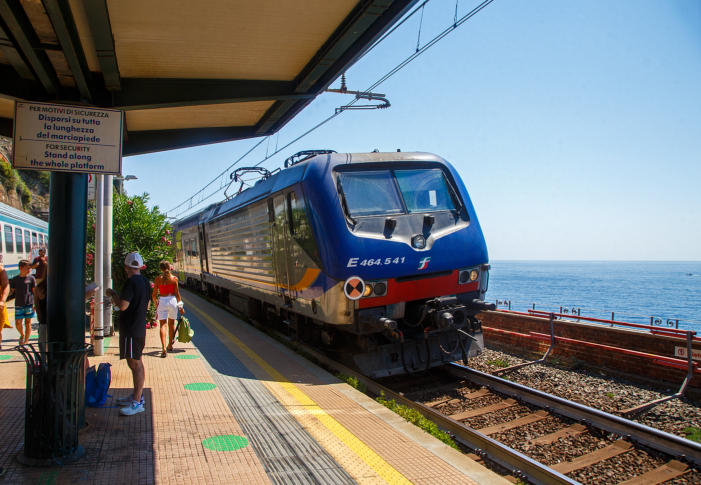 Die Trenitalia E.464.541 erreicht mit dem Cinque Terre Express (Regionale La Spezia Centrale – Levanto) am 21.07.2022 den Cinque Terre Bahnhof Corniglia.

Corniglia hat zwar diesen Bahnhof an der Bahnstrecke Pisa–Genua, aber Corniglia ist das einzige Dorf der Cinque Terre (5 Dörfer) das nicht direkt am Meer und so ist man nicht direkt vom Bahnhof im Ort. Sondern der Ort ist auf einem Bergvorsprung in etwa 100 m Höhe, umgeben von drei großen Weinbergflächen und einer steilen Klippe zum Meer. So müsste man hier vom viel tiefer gelegenen Bahnhof aus über die Lardarina, eine lange Ziegelsteintreppe, laufen. 

Wer wie wir aber die Cinque Terre Card Treno (Zugkarte) hat, könnte sich aber auch mit den Minibusen des Cinque Terre Parks (im Preis der Cinque Terre Treno Card eingeschlossen) die über 1 km lange Strecke hinauf fahren lassen. Aber die Busse waren uns einfach zu voll. Mit der Karte hat man auch Zutritt zu den beiden gebührenpflichtigen Wanderwegen des Cinque Terre Parks.
