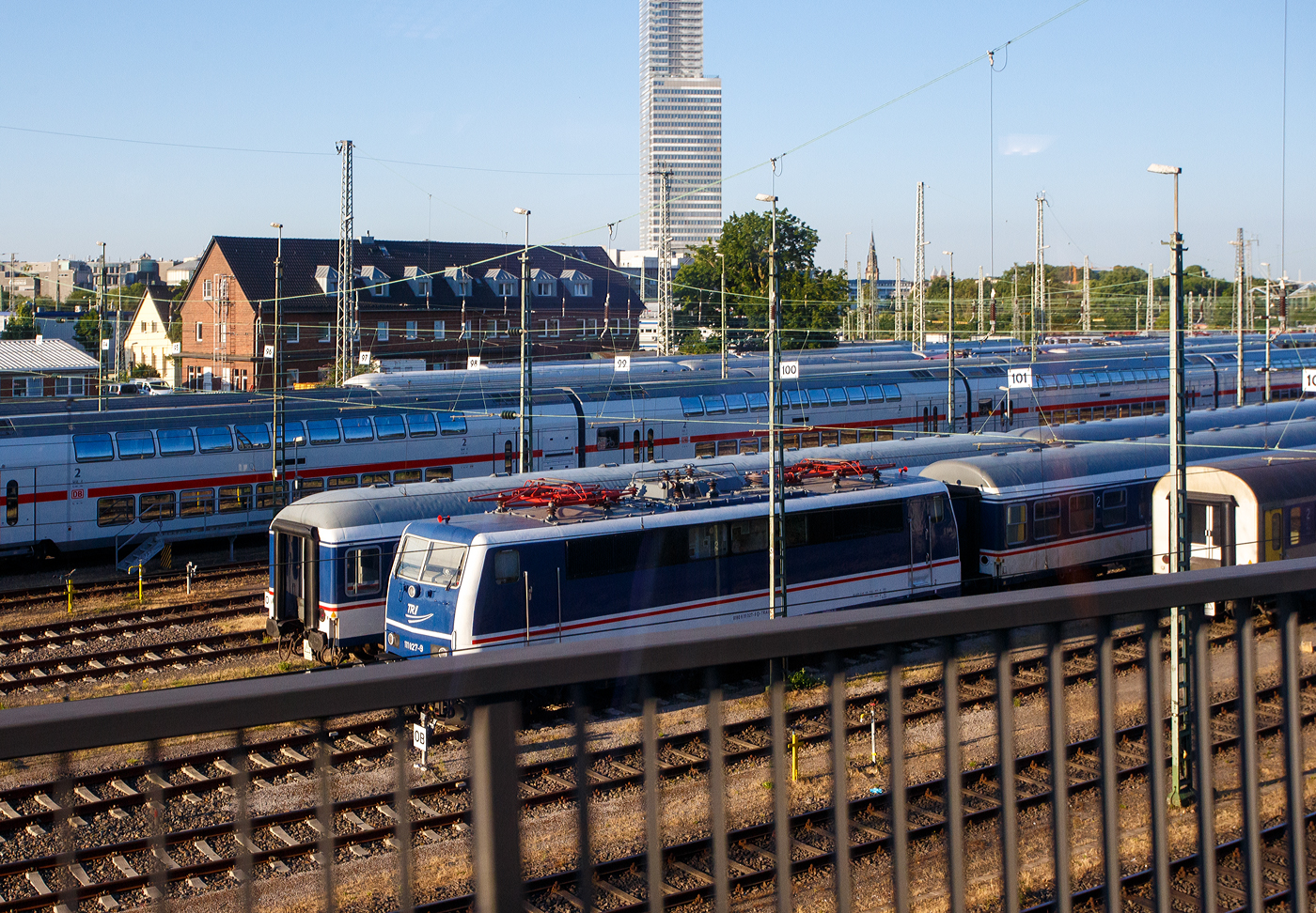 Die TRI 111 027-9 (91 80 6111 027-9 D-TRAIN) der TRI Train Rental GbR (Eckental-Eschenau) in National Express Lackierung steht am 01 Juli 2025 beim DB Betriebsbahnhof Köln (Gladbacher Wall).

Die Lok wurde 1976 von Krauss-Maffei in München-Allach unter der Fabriknummer 19764 gebaut und als 111 027-9 an die Deutsche Bundesbahn geliefert. Der elektrische Teil ist von Siemens. 2023 wurde sie von der DB Regio AG an die TRI Train Rental GbR verkauft. Sie besitzt eine Konventionelle-Wendezug-Steuerung (36-poliges Kabel), eine Zeitmultiplexe-Wendezug-Steuerung (UIC-Kabel) und eine Zeitmultiplexe-Doppeltraktions-Steuerung (UIC-Kabel).

Vielleicht liegt es an der Lackierung, aber wenn ich hier nicht deutlich die Nummer hätte lesen können, dann wäre ich nicht gleich auf eine 111er gekommen.

Die TRI Train Rental GmbH ist ein deutsches Eisenbahnverkehrsunternehmen, welches sich der Erhaltung historischer Schienenfahrzeuge widmet. Über ihr eigentliches Ziel, die betriebsfähige Aufarbeitung eines Triebzugs der Baureihe 403 hinaus, hat sich TRI zu einem Dienstleister für Sonder-, Ersatz- und Notverkehre entwickelt. Im Dezember 2018 begann die TRI mit Fahrten des Verkehrsvertrages Sonderzüge NRW.