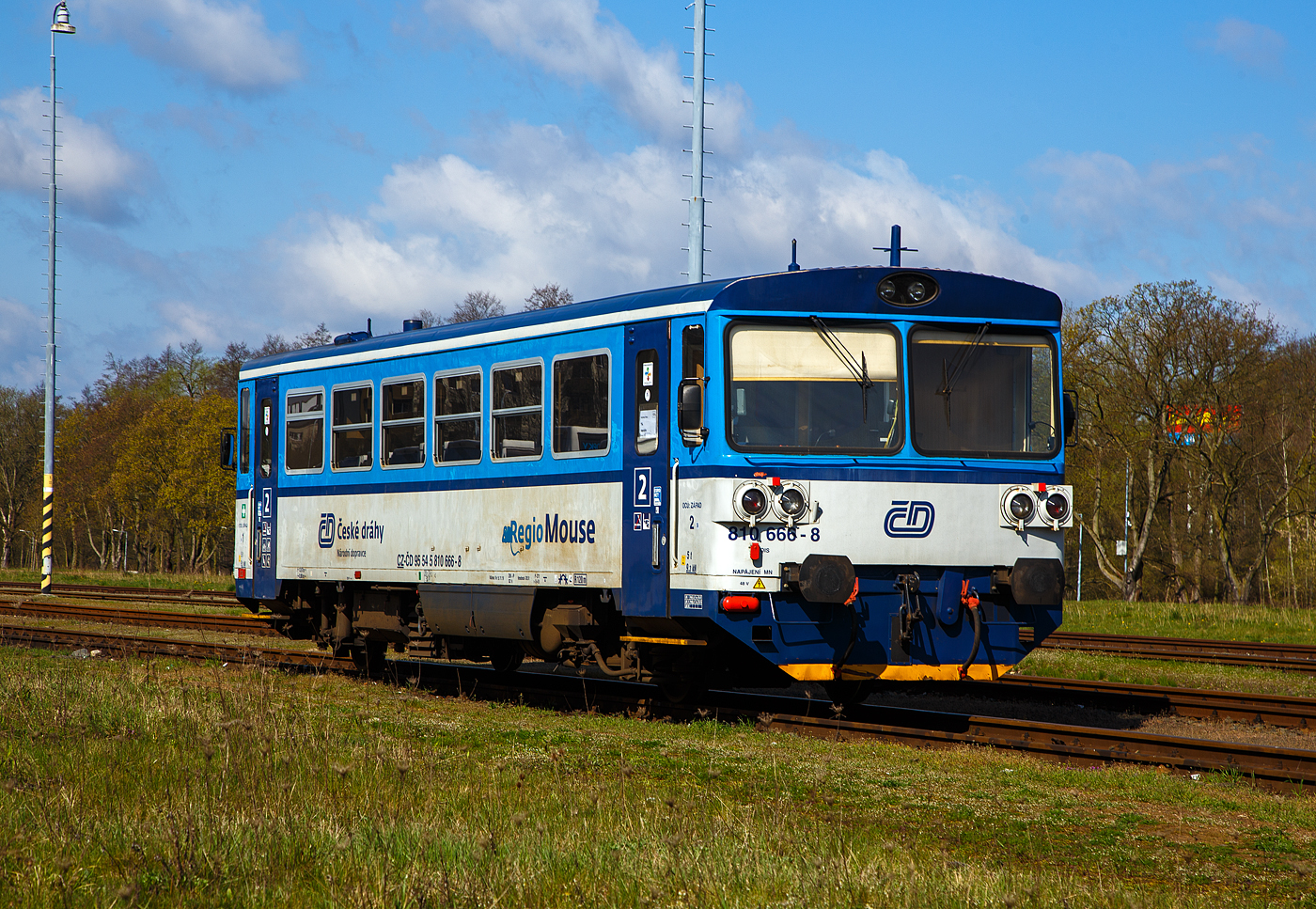 Die zur „RegioMouse“ modernisierte “Chc�p�k”  (Brotb�chse) bzw. der zweiachsige Dieseltriebwagen ČD 810 666-8 (CZ-ČD 95 54 5 810 666-8), ex ČSD M 152.0566, ist am 19.04.2023 beim Bahnhof Karlovy Vary doln� n�dra�� (Karlsbad unterer Bahnhof) abgestellt.

Der Dieseltriebwagen wurde 1982 von Vag�nka Stud�nka unter der Fabriknummer  87866  f�r die damalige ČSD Československ� st�tn� dr�hy (Tschechoslowakischen Staatsbahnen als ČSD M 152.0666 gebaut.

Die zweiachsige Dieseltriebwagen f�r den Regionalverkehr wurden als Baureihen M 152.0 (ab 1988: Baureihe 810) f�r die Tschechoslowakischen Staatsbahnen (ČSD) gebaut. Die Fahrzeuge bilden die dritte Generation zweiachsiger Triebwagen der ČSD. Die seit 2018 einer zweiten Modernisierung unterzogenen Fahrzeuge der ČD-Baureihen 809 und 810 werden als „RegioMouse“ vermarktet.

Ab 1975 wurden bei Vagonka Tatra in Stud�nka (heute �koda Vagonka a.s.) in sieben Bauserien 680 zweiachsige Dieseltriebwagen f�r die ČSD als Baureihe M 152.0 gebaut. Nahezu baugleiche Fahrzeuge wurden an die Ungarischen Staatsbahnen (M�V), als Bzmot, geliefert. Passend zu den Triebwagen wurden entsprechende Beiwagen vom Typ Blm geliefert, welche in Aufbau und Aussehen identisch mit den Triebwagen sind. Jedem Triebwagen konnten zwei Beiwagen beigegeben werden. Aufgrund der eckigen Aufbauten erhielten die Triebwagen von deutschen Eisenbahnfreunden den Spitznamen „Brotb�chse“.

Zwischen 1987 und 1990 f�hrten die ČSD EDV-gerechte Triebfahrzeugnummern ein. In der �bergangszeit wurden die EDV-Nummern zus�tzlich zu den alten Gussschildern mit Klebeziffern angebracht. Die Triebwagen erhielten die Reihenbezeichnung 810, die Beiwagen 010. Beide Nachfolgeunternehmen der ČSD behielten den Nummernplan bei, allerdings wurden freiz�gig einsetzbare Beiwagen 2009 auch nummernm��ig in den Reisezugwagenpark aufgenommen.

Nach der Teilung der Tschechoslowakei in die Nachfolgestaaten Tschechien und Slowakei am 1. Januar 1993 wurden Trieb- und Beiwagen auf die neugegr�ndeten Staatsbahnen ČD und �SR aufgeteilt. In der Slowakei geh�ren die Fahrzeuge heute zum Bestand des Nachfolgeunternehmens �elezničn� spoločnosť Slovensko (ZSSK).

Technische Merkmale:
Die Triebwagen haben keine Vielfachsteuerung, passende Steuerwagen existieren nicht. Deshalb muss bei mehrteiligen Einheiten jeder Triebwagen mit einem Triebfahrzeugf�hrer besetzt sein. Die Triebwagen m�ssen, wenn sie mit entsprechenden Beiwagen verkehren,  an Endbahnh�fen stets an die jeweilige Zugspitze umgesetzt werden.

Aufbau des Triebwagens:
Der Triebwagen ist eine Leichtbaukonstruktion. Der Wagenkasten besteht aus gewalzten und abgekanteten Stahlprofilen, die mit Stahlblech verkleidet sind. Innen ist das Gerippe mit Spanplatten, die mit Sprelacart �berzogen sind, verkleidet. Der Fu�boden besteht aus wasserbest�ndigem Sperrholz von 15 Millimetern Dicke und ist mit einer zwei Millimeter starken Schicht aus PVC beklebt. An jedem Ende des Wagenkastens befindet sich ein vom F�hrerstand abgetrennter Einstiegsraum, der auf beiden Seiten jeweils eine vom F�hrerstand schlie�bare pneumatische Schiebet�r besitzt.

Das Fahrgastabteil besitzt 56 Sitzpl�tze in der Anordnung 3+2 mit Mittelgang, die urspr�nglich schaumgummigepolstert waren. Zus�tzlich bietet ein Wagen etwa 40 Stehpl�tze. Der Fahrgastraum hat auf jeder Seite sechs Fenster mit der lichten Weite von 1316 � 841 mm, deren oberer Teil klappbar ist. Gro�e Frontscheiben mit Scheibenheizung, Scheibenwischern und Sonnenschutzblende erm�glichen eine gute Streckenbeobachtung. Durch die Anordnung einer zus�tzlichen Trennwand fielen die F�hrerst�nde sehr kurz aus. Um eine befriedigende Sitzposition f�r den Triebwagenf�hrer zu erm�glichen, musste die Trennwand im Bereich seines Sitzes ausgeschnitten werden. Der Ausschnitt ist mit einer in den Einstiegsraum reichenden Blechabdeckung verschlossen.

Die Beiwagen entsprechen im Aufbau den Triebwagen, abgesehen von der fehlenden Antriebsanlage. An Stelle der F�hrerst�nde ist an den Wagenenden eine durchgehende Sitzbank vorhanden.

Laufwerk und Antriebsanlage:
Gef�hrt wird das Fahrzeug von zwei einachsigen Drehgestellen, von denen eines �ber eine Gelenkwelle angetrieben wird. Damit sind beide Rads�tze im Bogen radial einstellbar. Die Drehgestelle st�tzen sich mit Schraubenfeder auf den Achslagern ab. Die Aufh�ngungen sind mit dem Wagenkasten �ber Gummibl�cke verbunden. Auf der Treibachse, die beidseitig gesandet werden kann, sitzt das Wendegetriebe zur Umsteuerung der Fahrtrichtung. Bei den Triebwagen sind beide Rads�tze mit einer Spurkranzschmiereinrichtung ausger�stet.

Als Antriebsanlage ist ein nicht aufgeladener Dieselmotor vom Typ LIAZ ML 634 unterflur eingebaut. Dieser besitzt sechs Zylinder in Reihe mit Direkteinspritzung und ist mit dem Getriebe vom Typ Praga 2M 70 direkt verbunden. Die gesamte Antriebsanlage besteht bis auf das Achswendegetriebe aus Komponenten, die vom Omnibus Karosa �M 11 �bernommen wurden. 

Die Antriebsanlage und die Hilfseinrichtungen wie Wasserk�hlung, �lw�rmetauscher, Batterie, Kraftstoffbeh�lter und Warmwasserheizung sind unterflur angeordnet. Deshalb d�rfen die Triebwagen Ablaufberge nicht befahren. Die Hilfsmaschinen, ein Wechselstromgenerator und ein Kompressor f�r die Druckluft der pneumatischen Bremse, werden �ber Gelenkwelle und Keilriemen vom Dieselmotor angetrieben. Der Dieselmotor ist wassergek�hlt, zus�tzlich ist ein L�fter mit hydrostatischem Antrieb vorhanden. Dieser wird in Abh�ngigkeit von der Motordrehzahl und der K�hlwassertemperatur automatisch geregelt.

�brige Einrichtungen:
Die Triebwagen sind mit indirekter Bremse und direkter Bremse nach dem System DAKO ausger�stet. Gesteuert wird diese mit dem F�hrerbremsventil �koda N – 0. Au�erdem ist eine Handbremse, die in beiden F�hrerst�nden bedient werden kann, vorhanden. In beiden Einstiegsr�umen und dem Fahrgastraum befinden sich Notbremsh�hne.

Beheizt wird das Fahrgastabteil des Triebwagens durch Warmluft. Hierzu wird das K�hlwasser aus dem Motorkreislauf einem W�rmetauscher zugef�hrt, der unter den Sitzen angebracht ist. Bei nichtarbeitendem Dieselmotor wird ein Vorw�rmger�t verwendet. Der F�hrerstand wird mit einer Warmwasserheizung beheizt. Die Beiwagen werden elektrisch beheizt. Bel�ftet wird das Abteil der Reisenden �ber Dachl�fter. Die Beleuchtung des Fahrgastabteiles �bernimmt der Wechselstromgenerator. Durch die Ausr�stung der Trieb- und Beiwagen mit Seitenpuffern und Schraubenkupplung ist es m�glich, die Fahrzeuge mit anderen Fahrzeugen zu kuppeln. Daher k�nnen die Triebwagen vereinzelte G�tertransporte auf Nebenbahnen durchf�hren. Die Schraubenkupplungen entsprechen der bei Dieseltriebwagen der ČSD �blichen leichten Ausf�hrung, die damit ausger�steten Wagen d�rfen in Regelz�gen nur am Schluss eingestellt werden.

Umbauten in Tschechien  (der ČD): 
1994 begann der Umbau von 28 Einheiten f�r den schaffnerlosen Betrieb. Dabei wurde die Inneneinrichtung ge�ndert. 1996 wurden diese Einheiten in die ČD-Baureihe 809 umgezeichnet.

Von 2005 bis 2012 wurden die Fahrzeuge der ČD durch die Firma Pars Nova (geh�rt zu �koda) grundlegend modernisiert und umgebaut. Dabei entstanden zweiteilige Einheiten, die jeweils aus einem Triebwagen und einem teilweise niederflurigen Steuerwagen bestehen. Ein Teil der Triebz�ge wurde als dreiteilige Einheit mit zwei Triebwagen und einem dazwischen eingestellten Beiwagen zusammengestellt. Bei den Wagen, die einen zwischen den Rads�tzen abgesenkten Wagenboden erhielten, wurden die Einstiege von den Enden in Wagenmitte verlegt.

Im Februar 2018 wurde als letzte Modernisierung die Baureihe 816 von GW Train Regio vorgestellt.

Einsatz:
Die Fahrzeuge besitzen eine Zulassung f�r den Verkehr nach Deutschland und �sterreich. Im grenz�berschreitenden Nahverkehr geh�rten sie auf den Grenzbahnh�fen Zittau, Ebersbach (Sachs), Bad Schandau, Johanngeorgenstadt, Furth im Wald und Bayerisch Eisenstein zum t�glichen Bild. 

Trotz des Umbauprogrammes existieren nach wie vor einige Fahrzeuge, die sich bis auf eine Teilmodernisierung des Fahrgastraumes mit neuer Bestuhlung noch weitgehend im Originalzustand befinden. Sie kommen weiterhin auf Strecken mit geringem Verkehrsaufkommen planm��ig zum Einsatz. Bei den ČSD war es �blich, Beiwagen von Verbrennungsmotortriebwagen auch als lokbespannte Reisez�ge einzusetzen. Die Nachfolger behielten diese Betriebsweise bei.

TECHNISCHE DATEN :
Hersteller: ČKD Vag�nka in Stud�nka (heute �koda Vagonka a.s.)
Spurweite: 1.435 mm (Normalspur)
Achsformel: 1'A' 
L�nge �ber Puffer: 13.970 mm
H�he: 3.500 mm
Achsabstand: 8.000 mm
Dienstgewicht: 20 t
Radsatzfahrmasse: 10 t
H�chstgeschwindigkeit: 80 km/h
Installierte Leistung: 155 kW (bei 1.950 U/min)
Anfahrzugkraft: 29 kN 
Motorbauart: Sechszylinder-Reihendieselunterflurmotor
Motorentyp: LIAZ ML 634
Motorhubraum: 11,946 Liter (Zylinder-� 130 mm / Kolbenhub 150 mm)
Nenndrehzahl: 2.150 U/min (Leerlaufdrehzahl 600 U/min)
Kompressionsverh�ltnis: 12,5 : 1
Getriebe: Praga 2M70
Leistungs�bertragung: hydromechanisch
Sitzpl�tze: 55
Tankinhalt: 300 l
Fu�bodenh�he: 570 mm (Niederflurteil)
Kleinster befahrbarer Gleisbogen: R 100 m

Quellen: Wikipedia, atlaslokomotiv.net