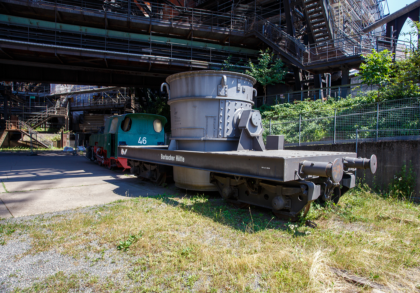 Ein vierachsiger normalspuriger offener Roheisenpfannenwagen der Burbacher H�tte hinter der Normalspur-Dampflokomotive 46, einer Jung Hochofenlok niedriger Bauart, der V�lklinger H�tte (ehem. R�chling'schen Eisen- und Stahlwerke GmbH in V�lklingen/Saar, ab 1982 ARBED-Saarstahl GmbH, ab 1986 Saarstahl V�lklingen GmbH), ausgestellt als Denkmal am Gel�nde V�lklinger H�tte, hier am 01 Juli 2025 am Gel�nde V�lklinger H�tte als Denkmal. Heutiger Eigent�mer ist die Initiative V�lklinger H�tte e.V..

1971 fusionierten die Burbacher und V�lklinger H�tte, und ab 1975 wurde die Stahlproduktion in der Burbacher H�tte eingestellt. Das Bild zeigt einen offenen Pfannenwagen, mit dem das fl�ssige und hei�e Roheisen aus dem Hochofen aufgefangen wird, und dann zur Weiterverarbeitung mittels Werkseisenbahn zur Weiterverarbeitung in das angrenzende Stahl- und Walzwerk weitertransportiert wurde. Da die Entfernungen gering waren, ben�tigte man keine mit Schamott ausgemauerten Torpedopfannenwagen. Ob der Wagen hier auf der V�lklinger H�tte ist mit nicht klar, aber da er erheblich h�her ist als die Lok, so vermute ich das er hier keinen Einsatz fand.