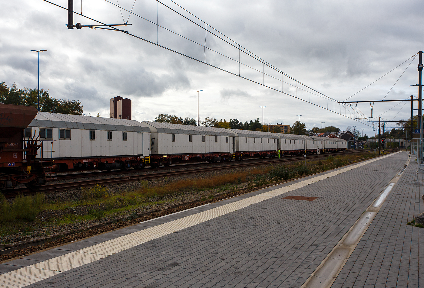 Ein Wohnzug des belgischen Infrastrukturunternehmens INFRABEL steht am 21 Oktober 2025 in Ans.

Die SNCB verf�gt �ber 7 dieser Wohn-/Schlafz�ge f�r schnelle Interventionen, in denen 20 bis 25 Personen autark leben k�nnen. Ein Zug besteht aus 8 vierachsigen Wagen sowie einem zweiachsigen Gbs-G�terwagen als Energiewagen. Der setzt sich aus f�nf Schlafwaggons, einem K�chen- und Speisewagen, einem B�ro- und Lagerwagen, einem Sanit�rwagen, sowie dem Energiewagen zusammen. Jeder Waggon verf�gt �ber eine eigene Wasserversorgung, einen Abwassertank, ein Heizsystem mit Heiz�l und einen Brandmelder. Elektrisch wird der gesamte Zug von dem Energiewagen versorgt, es kann zwischen fester Einspeisung (vom Abstellgleis) oder Versorgung �ber den im Energiewagen vorhandenen Generator gew�hlt werden. Der Speise- und B�robereich sind zudem mit einer Klimaanlage sowie den notwendigen TV- und Internetanschl�ssen ausgestattet. Siehe auch: http://warsco.eu/de/projekte/leeftrein-infrabel

Gebaut wurden die Aufbauten mit der Inneneinrichtung von der belgischen Firma Warsco NV (Gent), einem Containerbauer f�r tempor�re und permanente R�ume. Auch wenn es den Wagen von au�en nicht ansieht, so sind sie von innen sehr professionell eingerichtet. Bei den Untergestellen der 8 vierachsigen Wagen handelt es sich um 19,9 m langen Wagen der ehemaligen Gattung Res - Type 3514D1 (noch angeschrieben). Da den Wagen aber die Borde und Rungen beraubt wurden und daran noch �nderungen vorgenommen wurden, so d�rften sie eigentlich mit mehr „Res“ hei�en. Die Wagen sind hintereinander gekuppelt und �ber Faltenbalg-�berg�nge verbunden. Es handelt sich hierbei um Ma�anfertigungen, bei denen wir das Lichtraumprofil einhalten mussten, da die Z�ge durch Tunnel passen m�ssen.

Ja, man h�tte auch Containerwagen mit aufgesetzten Standard Wohn-Containern verwenden k�nnen, aber dann w�re das Lichtraumprofil gr��er und so nicht f�r jede Strecke verwendbar. 