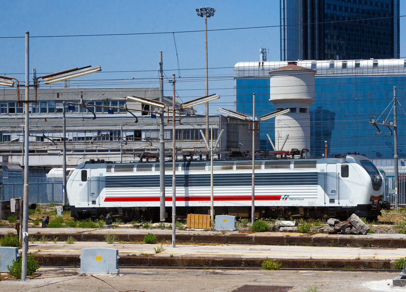 Eine Trenitalia E.403 (91 83 2402 0xx-8 I-TI), in weiß-grau-roter IC-Lackierung, ist am 16.07.2022 beim Bahnhof Napoli Centrale abgestellt. Die Aufnahme konnte ich aus einem ausfahrenden IC machen.

Die Trenitalia / FS E.403 baut auf die FS E.402B auf, war auch ursprünglich als E.402 C vorgesehen, haben aber einen anderen elektrischen und elektronischen Teil als die E.402B. 24 Loks wurden von AnsaldoBreda zwischen 2005 bis 2008 gebaut. 

Anfang der 2000er Jahre entwickelte Trenitalia Pläne zur Ausweitung seines Güterverkehrs auf das europäische Festland, insbesondere auf dem Korridor Italien-Österreich-Deutschland sowie der Schweiz. 
Eine neue Lokomotive musste konzipiert werden, damit die Pläne Wirklichkeit werden konnten, und wurde ursprünglich als E.402C bezeichnet. Es war eine Weiterentwicklung der E.402B-Lokomotive mit zusätzlicher Ausrüstung für den Betrieb in diesen Ländern und wesentlich anderen Hembot-Drehgestellen. Die Loks waren für den Einsatz vor schnellen Güterzügen vorgesehen und hatten ursprünglich auch vier Einholm-Stromabnehmer für Oberleitungen-Spannungen von 1,5 kV DC, 3 kV DC, 15 kV ~ 16 2/3 Hz und 25 kV ~ 50 Hz. 

Das Programm erlitt große Schläge: Als AnsaldoBreda diese Lokomotivenserie exklusiv für Trenitalia auf einer nicht standardmäßigen Plattform (im Gegensatz zu den Lokomotiven der TRAXX und EuroSprinter/Vectron, die sich Standardkomponenten teilen) baute, explodierten die Kosten. Die Lokomotive wurde verkleinert, indem die 1,5-kV- und 15-kV-Teile sowie die französischen, deutschen und österreichischen Sicherheitssysteme entfernt wurden. Stattdessen übernahm Trenitalia 51% der Anteile an TXLogistik und beantragte die Zulassung seiner E.412- Lokomotiven in Österreich und Deutschland. Die (eingeschränkte) österreichische und deutsche Zulassung wurde 2006 erteilt, wobei TXLogistik Lokführer die Züge in Österreich und Deutschland fahren.


Die Lokomotive sollte nun in schnellen Güterzügen eingesetzt werden, die teilweise auf den neuen Hochgeschwindigkeitsstrecken verkehren. Bis Februar 2010 verkehrte jedoch noch kein Güterzug auf den HS-Strecken und die E.403 waren noch nicht im Linienverkehr. In den ersten Monaten des Jahres 2010 beschloss die Trenitalia, diese Lokomotiven der Passagierabteilung zuzuordnen und erst 2012 erfolgte die endgültige Zulassung der Loks.

Aus der Mehrsystemlokomotive wurde eine rein italienische Zweisystemlokomotive für 3 kV Gleich- und 25 kV 50 Hz~ Wechselstrom. Die Baureihe E.403 kann so unter 3.000 V Gleichstromspannung, dem hauptsächlichen italienischen Bahnnetz, aber auch auf den italienischen Schnellfahrstrecken mit 25 kV, 50 Hz Wechselstrom fahren. Fernerhin kann sie unter 1.500 V Gleichstrom betrieben werden, dann hat sie aber nur die halbe Leistung. Die Lokomotiven verfügen über eine elektrische regenerative und rheostatische Bremse, sowie eine mechanische Scheibenbremse mit zwei Scheiben pro Achse. Die Loks haben auch ein variables Übersetzungsverhältnis von 45/71 oder 33/92. 

TECHNISCHE DATEN:
Hersteller: AnsaldoBreda
Gebaute Anzahl: 24 
Baujahre: 2005-2008 (Ineinssetzung 2012)
Spurweite:  1435 mm (Normalspur)
Achsformel: Bo'Bo'
Länge: 19.900 mm
Drehzapfenabstand: 10.450 mm
Achsabstand im Drehgestell: 2.750 mm
Treibraddurchmesser:  1.110 mm (neu)
Dienstgewicht: 86 t
Höchstgeschwindigkeit: 180 km/h
Übersetzungsverhältnis: variabel 45/71 oder 33/92
Stundenleistung: 6.000 kW
Dauerleistung: 5.600 kW (7.500 PS)
Anfahrzugkraft: 315 kN
Dauerzugkraft: 265 kN
Stromsysteme: 3000 V DC und 25 kV - 50 Hz AC 