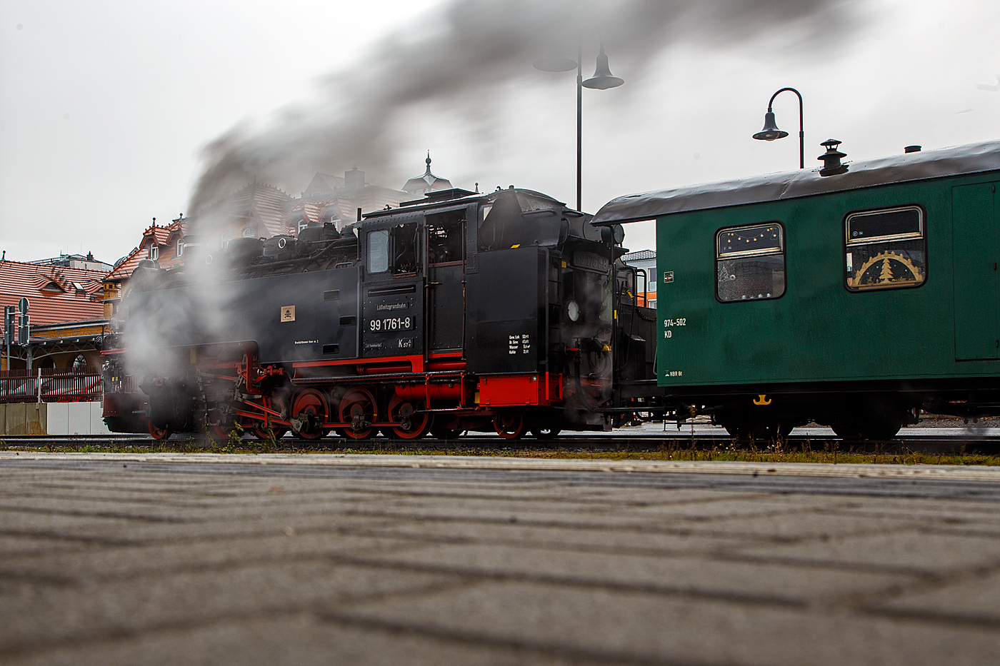 Es qualmt und dampft...
Die (s�chsische) VII K – Altbau 99 1761-8 steht am 07.12.2022  in Radebeul Ost, mit dem L��nitzdackel (L��nitzgrundbahn) . nun wieder zur Abfahrt nach Radeburg via Moritzburg bereit.

Die 750 mm-schmalspurige Dampflok der Altbau-Baureihe 99.73-76 wurde 1933 von der BMAG - Berliner Maschinenbau-Actien-Gesellschaft vormals L. Schwartzkopff in Berlin unter der Fabriknummer 10152 gebaut und als 99 761 an die DRG - Deutsche Reichsbahn-Gesellschaft geliefert.

Weitere Lebenslauf und Nummerierungen:
1933 bis 1970 - DRG / DRB / DR 99 761 
1970-1992 - DR 99 1761-8 
1992-1994 - DR 099 734-6 
1994-2004 - DB 099 734-6 
2004-2007 - BVO 99 1761-8 (Busverkehr Ober- und Westerzgebirge Bahn GmbH)
seit 2007- SDG 99 1761-8 (S�chsische Dampfeisenbahn Gesellschaft mbH)
Im Jahr 1964 bekam sie im Raw Cottbus einen Neubaukessel (Baujahr 1964, Fabriknummer 15).

Die 5-fach-gekuppelten Lokomotiven der Baureihe 99.73–76 waren Einheitslokomotiven der Gattung K 57.9  der Deutschen Reichsbahn f�r die s�chsischen Schmalspurbahnen. Zusammen mit der Nachfolgebauart Baureihe 99.77–79 stellen die Lokomotiven die st�rksten Schmalspurlokomotiven f�r 750 mm-Spurweite in Deutschland dar.

Obwohl mit der f�nffach gekuppelten Baureihe 99.67–71 schon eine recht leistungsf�hige Lokomotive f�r den Betrieb auf den Gebirgsstrecken im Erzgebirge vorhanden war, bestand auch weiterhin Bedarf an einer besonders leistungsstarken Bauart. So gelang es der neu gegr�ndeten Reichsbahndirektion Dresden, die Beschaffung einer Einheitslokomotive f�r 750 mm-Spur durchzusetzen. Das Vereinheitlichungsb�ro der Deutschen Lokomotiv-Vereinigung in Berlin-Tegel erarbeitete den Entwurf f�r die Konstruktion.

Die erste Serie von 13 Lokomotiven fertigte die S�chsische Maschinenfabrik vormals Richard Hartmann in Chemnitz. Laut Liefervereinbarung sollte die S�chsische Maschinenfabrik noch weitere Loks liefern, durch den Konkurs und die Liquidation des Unternehmens 1930 ging dieser Auftrag an die Berliner Maschinenbau AG vormals Schwartzkopff (BMAG) �ber. 1928 wurden sieben und 1933 noch weitere zw�lf Lokomotiven von der BMAG geliefert. Die damals hochmodernen Lokomotiven entsprachen in ihrer Konstruktion den regelspurigen Einheitslokomotiven. Die Lokomotiven erf�llten die Erwartungen. Mit Vorspann war es nun m�glich, auch �berlange Schmalspurz�ge mit bis zu 56 Achsen bergw�rts zu bef�rdern.

1945 mussten zehn Lokomotiven als Reparationsleistung an die Sowjetunion abgegeben werden. Zudem erhielten die Loks dort auch einige, bauliche �nderungen. Die hintere Laufachse wurde entfernt, und sie wurden alle auf �lfeuerung umgebaut und mit Schlepptendern ausger�stet. Zwischen 1975 und 1979 wurden alle Maschinen der UdSSR ausgemustert. Es waren die Loks 733, 736, 737, 744, 748, 751, 752, 753, 755 und 756. Demgegen�ber stand eine enorme Zunahme der Verkehrsleistung auf den Schmalspurbahnen im Erzgebirge durch den neu aufgenommenen Uran-Bergbau der SDAG Wismut. Um dem daraus resultierenden Lokomotivmangel abzuhelfen, entstand ab 1952 eine �hnliche Nachfolgebauart beim VEB Lokomotivbau Karl Marx in Babelsberg als Baureihe 99.77–79.

Ende der 1960er Jahre mussten wegen Sch�den an den Kesseln die ersten Lokomotiven ausgemustert werden. Zehn Lokomotiven erhielten neue, geschwei�te Kessel und wurden auch weiterhin auf ihren Stammstrecken eingesetzt. Die 99 1760 wurde 1992 auf �lhauptfeuerung umgebaut.

Technische Merkmale:
Die f�nffach gekuppelten Lokomotiven haben einen Barrenrahmen und verf�gen �ber in Bisselgestellen gelagerte Laufachsen. Als Treibachse dient die fest gelagerte dritte Achse, welche anfangs geschw�chte Spurkr�nze aufwies. Nach 1945 wurden die Spurkr�nze dann v�llig entfernt, um die Bogenl�ufigkeit weiter zu verbessern. Die zweite und die f�nfte Kuppelachse waren seitenverschiebbar. Der feste Achsstand betrug anfangs 3.000 Millimeter, wurde dann aber sp�ter auf 4.000 Millimeter verl�ngert. Wie f�r alle Einheitslokomotiven typisch, wurden die Lokomotiven 99 731 bis 99 750 mit Kolbenspeisepumpe und einen quer �ber der Rauchkammer eingebauten Knorr-Oberfl�chenvorw�rmer geliefert. Die 99 751 bis 99 762 wurden dagegen mit Abdampfinjektor Bauart Friedmann geliefert, sp�ter jedoch ebenfalls auf Knorr-Vorw�rmer umgebaut. Die zweite Kesselspeisevorrichtung ist eine saugende Dampfstrahlpumpe. Der Langkessel bestand aus zwei Sch�ssen.

Wegen der damals noch teilweise gebr�uchlichen Heberleinbremse erhielten die Lokomotiven ab Werk auch die daf�r erforderliche Ausr�stung mit Rollenf�hrungen und Haspel. Die Lokomotive selbst bekam eine Knorr-Druckluftbremse, welche �ber die Saugluftbremse f�r den Wagenzug angesteuert wird. Als die ersten Lokomotiven 1928 ausgeliefert wurden, war schon geplant, die veraltete Trichterkupplung durch die Scharfenbergkupplung abzul�sen. So erhielten die ersten Lokomotiven zun�chst Trichterkupplungen. Diese wurden sp�ter problemlos gegen die neuen Kupplungen getauscht.

TECHNISCHE DATEN:
Bauart:  1’E1’ h2t
Gattung:  K 57.9
Spurweite:  750 mm
L�nge �ber Kupplung:  10.540 mm
H�he:  3.570 mm
Fester Radstand:  4.000 mm
Gesamtradstand:  7.600 mm
Kleinster befahrbarer Radius:  50m
Leergewicht:  44,3 t
Dienstgewicht:  56,7 t
Reibungsmasse:  46,1 t
H�chstgeschwindigkeit:  30 km/h
Indizierte Leistung:  600 PSi, 441 kW
Anfahrzugkraft:  83,35 kN
Steuerungsart:  Heusinger
Zylinderanzahl:  2
Kessel�berdruck:  14 bar
Wasservorrat:  5,80 m�
Brennstoffvorrat:  2,5 t Kohle
Lokbremse:  Knorr-Druckluftbremse, urspr�nglich saugluftgesteuert, mit Zusatzbremse
Zugbremse:  K�rting-Saugluftbremse, anfangs Heberleinbremse, heute Knorr-Druckluftbremse
Zugheizung:  Dampf
Kupplungstyp:  Scharfenbergkupplung