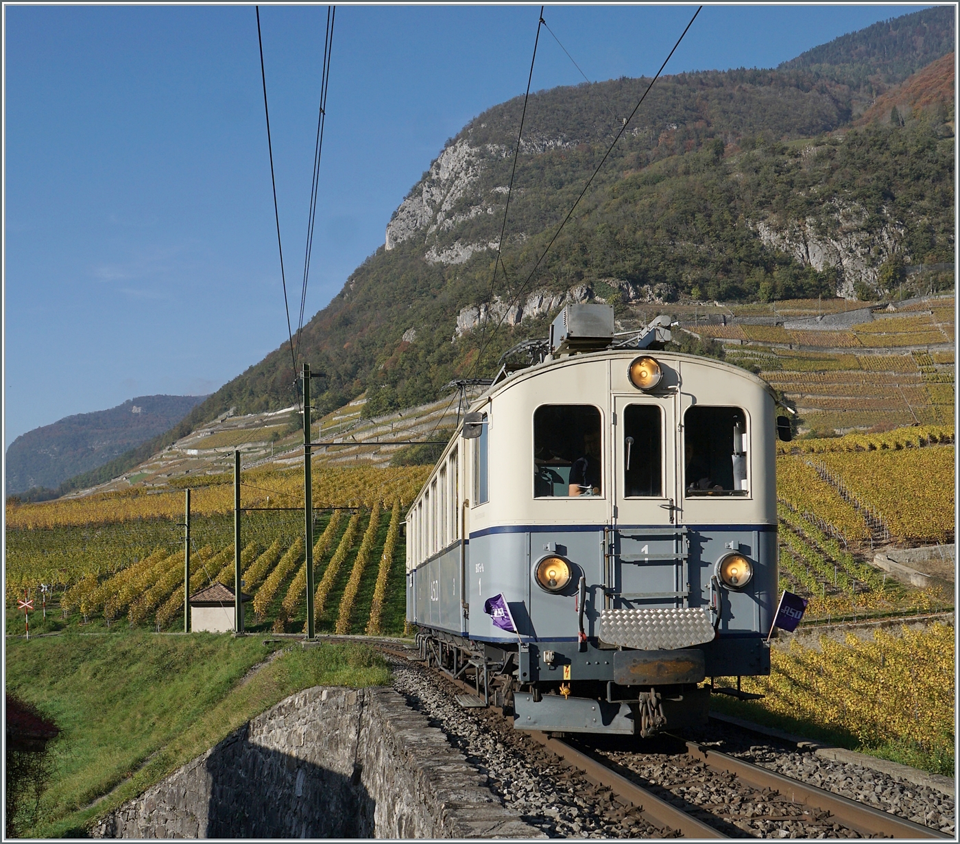 Es zeigte sich, dass es am Nachmittag gar nicht so einfach ist, eine lichtmässige gute Stelle zum fotografieren eines nach Les Diablerets fahrenden Zuges gibt. Und so wählte ich die erst vor gut eineinhalb Stunden vorher entdeckte Stelle für den Association ASD 1914 BCFe 4/4 N° 1 Extrazug, der dann keine Minute zu spät kam, denn hinter meinem Rücken rückte der Schatten der Berge drohen schnell heran. 
Der Association ASD 1914 BCFe 4/4 in den Rebbergen bei Aigle auf der Fahrt in Richtung Les Diablerets.  

2. Nov. 2024
