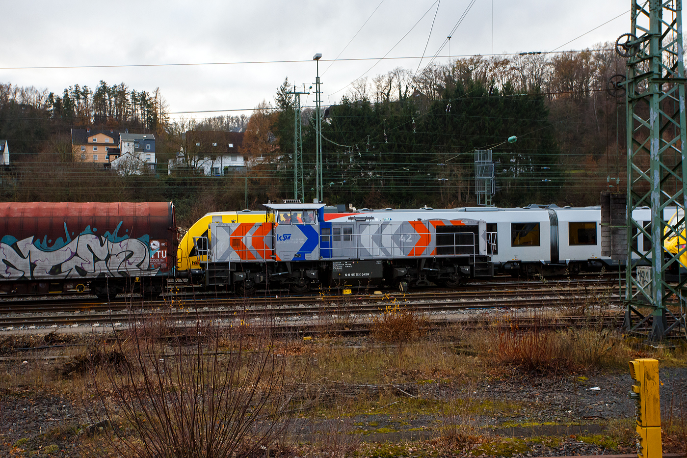 Geführt von der KSW 44 (92 80 1271 004-4 D-KSW), eine MaK G 1000 BB, fährt am 04 Dezember 2025 die KSW (Kreisbahn Siegen-Wittgenstein), im Sandwich mit einem sehr langen und schweren Coilzug, vom Rangierbahnhof Betzdorf/Sieg in Richtung Herdorf zum KSW-Rangierbahnhof (Betriebsstätte FGE - Freien Grunder Eisenbahn) nun los. Hinten hier im Bild nun die nachschiebende KSW 42 bzw. 277 902-3 (92 80 1277 902-3 D-KSW) eine Vossloh MaK G 1700 BB. 

Die Fuhre geht ja über die, nicht elektrifizierte, eingleisige KBS 462 „Hellertalbahn“, da nur eine Güterverkehrsfahrt zwischen den Personenverkehr der RB 96 passt, fährt die KSW lieber eine lange Fuhre im Sandwich. Für eine Lok wäre die Anhängelast eines solchen langen beladenen Coilzuges zu hoch. In Herdorf auf dem Rangierbahnhof der KSW, werden Züge in mehren Teile aufgeteilt und gehen dann über die KSW eigene Strecke NE 447 (ehem. Freien Grunder Eisenbahn nach Neunkirchen-Salchendorf (ehemals Pfannenberger Einigkeit) zu den Produktionshallen der EMW Stahl Service GmbH, ein Geschäftsbereich der SCHÄFER WERKE Gruppe. 

Schon heute werden so dorthin über 300.000 Tonnen Stahl pro Jahr über die Schiene angeliefert, zukünftig sind sogar 600.000 Tonnen geplant.