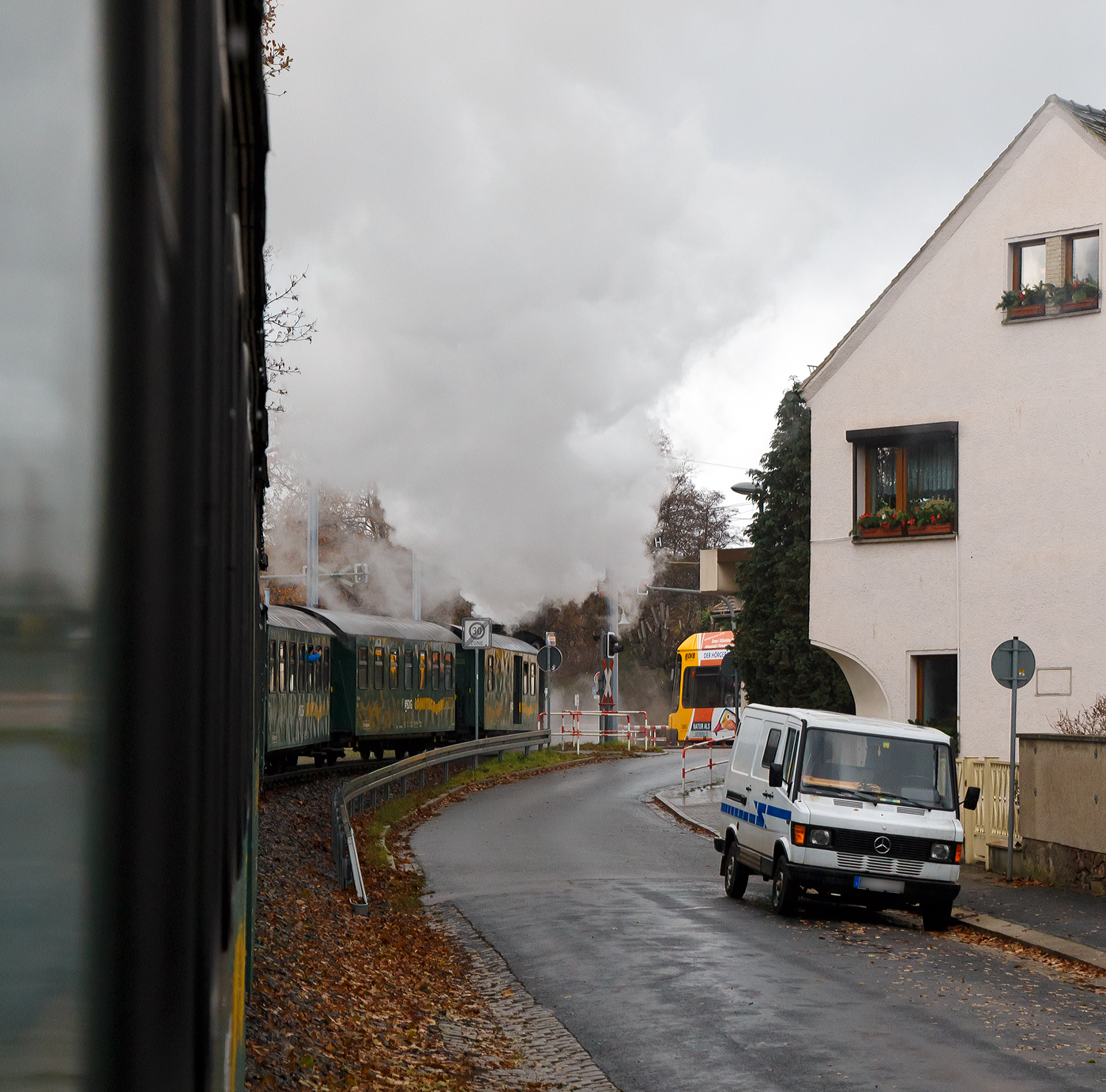 Gezogen von der s�chsischen VII K (Altbau) 99 1761-8 der „L��nitzdackel“  bzw. der Dampfzug der L��nitzgrundbahn am 07.12.2022 in Radebeul die Mei�ner Stra�e und somit bald den direkt dahinter liegenden Haltepunkt Wei�es Ro�. Die Schranken sind schon unten und so muss auch der NGT 6 DD Niederflur-Gelenktriebwagen der Dresdner Stra�enbahnlinie 4 halten