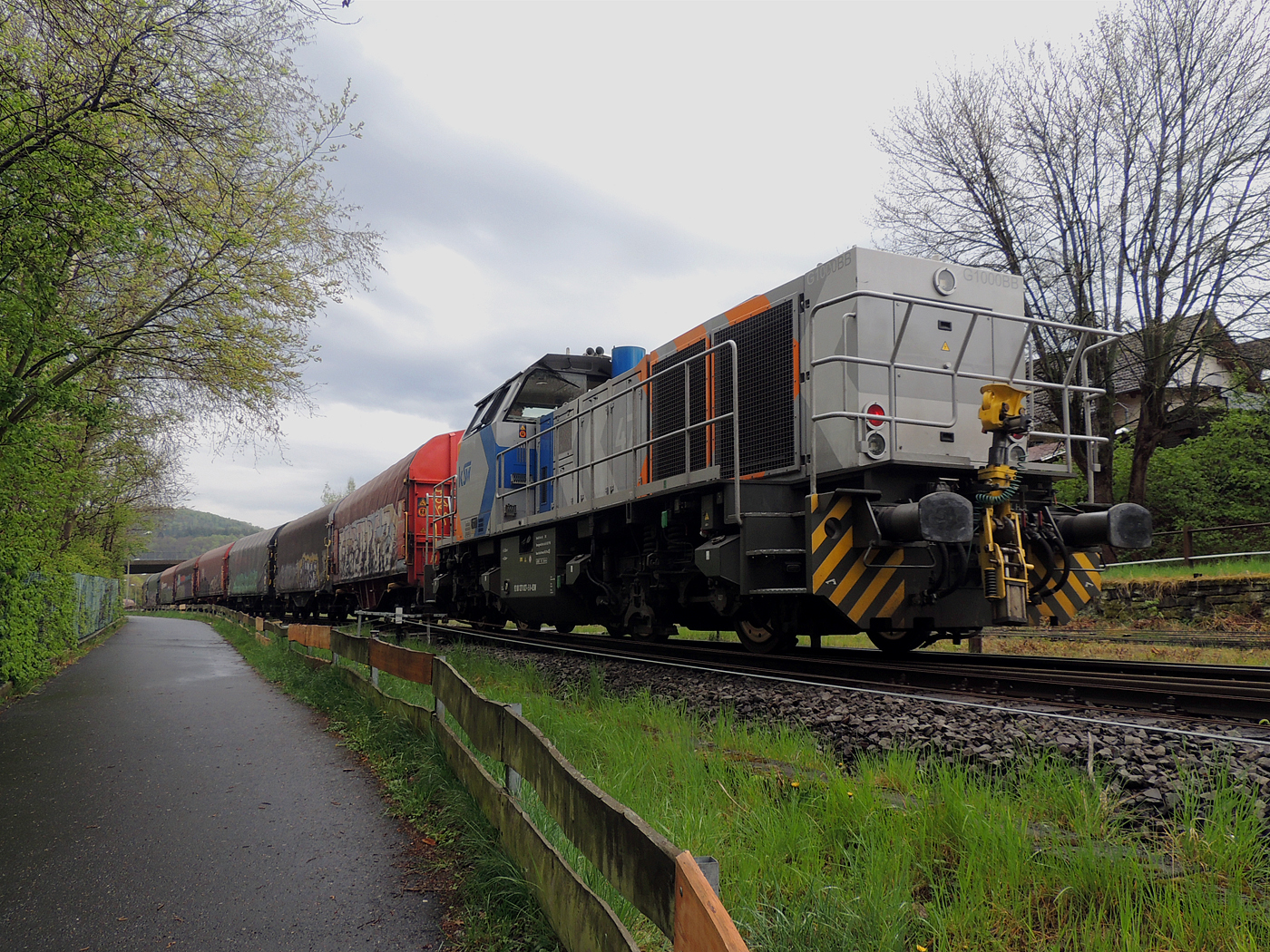 Hochbetrieb in Herdorf am 23 April 2025: 
Durch die vergangenen Osterfeiertage braucht es wohl wieder Nachschub. Die KSW (Kreisbahn Siegen-Wittgenstein) kommt im Sandwich mit einem sehr langen und somit schweren Coilzug, von via Betzdorf/Sieg kommend, und erreicht den KSW-Rangierbahnhof (Betriebsstätte FGE - Freien Grunder Eisenbahn).

Hier am Zugschluss die nachschiebende KSW 47 (92 80 1271 027-5 D-KSW), ex D 2 der HFM, eine Vossloh G 1000 BB, vorne als Zuglok die KSW 44 (92 80 1271 004-4 D-KSW) auch eine MaK G 1000 BB. Im Rbf wird der Zug geteilt, da er für die Weiterfahrt sonst zu lang wäre, und die KSW 44 zieht den ersten Teil weiter zu den Schäfer Werke KG am Pfannenberg in Neunkirchen-Salchendorf. 

Die KSW-Bahnstrecke Herdorf–Pfannenberg-(ehem. Unterwilden) ist eine rund 8 km lange Nebenbahn, bekannt ist sie auch als „Talbahn“. Die Strecke wurde von der 1904 gegründeten Freien Grunder Eisenbahn AG betrieben. Die gebliebenen Gleise und Anlagen sind seit 1970, als Betriebsstätte FGE - Freien Grunder Eisenbahn. Teil der heutigen Kreisbahn Siegen-Wittgenstein.

Später kam dann noch die KSW 43 (92 80 1273 018-2 D-KSW), die asymmetrische Vossloh G 2000 BB, mit einem langen Coilzug von Duisburg an.