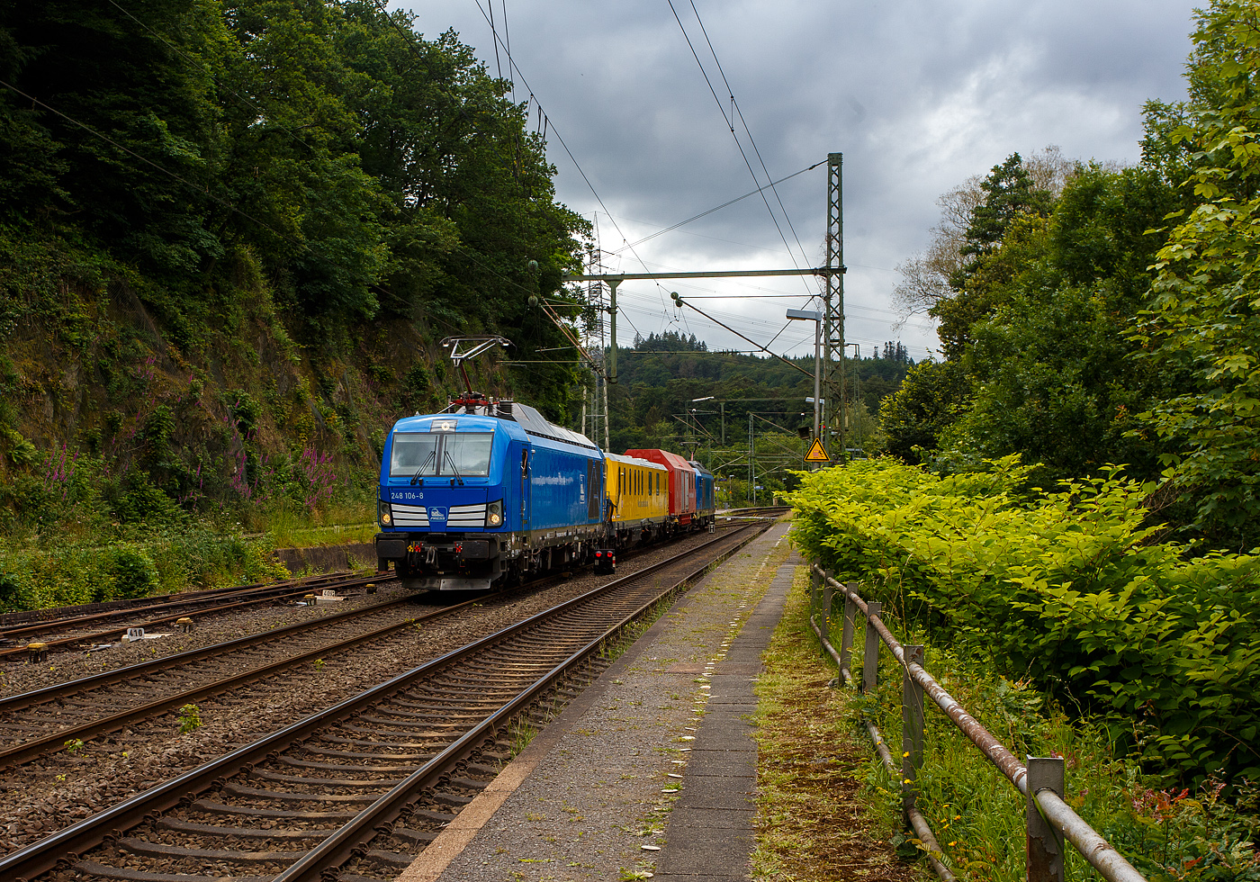 Im Sandwich zweier SIEMENS Vectron Dual Mode fährt ein Schienenprüfzug (SPZ 3), auf Prüffahrt (der Messwagen ist auf die Schiene absenkt) am 14 Juni 2024 durch Scheuerfeld/Sieg in Richtung Siegen.

Die vierteilige Komposition bestand aus:
• Der SIEMENS Vectron Dual Mode der 248 027-5 (90 80 2248 027-5 D-PRESS) alias 248 106-8 der PRESS (Eisenbahnbau- und Betriebsgesellschaft Pressnitztalbahn mbH, Jöhstadt).
• Dem Messwagen SPZ-STW (STW steht für Steuerwagen) 720 301(99 80 9360 006-7 D-DBMP) der DB InfraGO AG, ehemals DB Netz AG (NetzInstandhaltung/Fahrwegmessung).
• Einem Hilfszug-Wagen (Nummer unbekannt) der DB Netz AG (Notfalltechnik) bzw. DB InfraGO AG.
• Und der SIEMENS Vectron Dual Mode der 248 026-7 (90 80 2248 026-7 D-PRESS) alias 248 105-9 der PRESS (Eisenbahnbau- und Betriebsgesellschaft Pressnitztalbahn mbH, Jöhstadt).

Die Energieversorgung vom Messwagen und dem Hilfszug-Wagen erfolgte von den Loks (spartanisch) über außenverlegte Kabel.

Normalerweise ist der Schienenprüfzug ein zweiteiliger Messtriebwagen, bestehend aus Trieb- (ATW - 719 301) und einem Steuerwagen (STW - 720 301), siehe u.a. http://hellertal.startbilder.de/bild/Deutschland~Unternehmen~DB+Netz+AG/773623/der-plasser--theurer-schienenpruefzug-der.html Warum es nun diese Komposition ist, das ist mir nicht bekannt, vielleicht setzt man nun noch mehr auf E-antrieb.

Der Schienenprüfzug wurde 2015 von Plasser & Theurer in Linz (A) unter der Fabriknummer 6003 (SPZ-STW) gebaut. Um Schäden am Oberbau frühzeitig zu erkennen, setzt die Deutsche Bahn AG verschiedene Prüfzüge der Baureihen 719 und 720 ein. Mittels zweier zerstörungsfreier Prüfverfahren werden die Schienen auf Schädigungen untersucht. Bei der Ultraschallprüfung können Materialfehler durch Materialermüdung innerhalb der Schiene bis zum Schienenfuß erkannt werden. Mit der Wirbelstromprüfung wird der Schienenkopf geprüft.

Die beiden SIEMENS Vectron Dual Mode wurden 2022 von SIEMENS in München-Allach, unter den Fabriknummern 23168 und 23169, gebaut und an die PRESS - Eisenbahnbau- und Betriebsgesellschaft Pressnitztalbahn mbH in Jöhstadt geliefert. Die beiden Vectron DM haben die Zulassung in Deutschland für eine Höchstgeschwindigkeit 160 km/h.

Der Vectron Dual Mode vereint die Vorteile einer vollwertigen Diesellokomotive mit denen von elektrischen Lokomotiven. Dank des leistungsstarken Dieselantriebs sowie der Ausstattung für die Nutzung der Fahrleitung kann man jederzeit flexibel auf die Traktionsanforderungen reagieren. So bleibt man immer in Bewegung, egal ob mit oder ohne Fahrdraht. Wo ein Fahrdraht ist, sollte man ihn nutzen. Denn der Betrieb unter Oberleitung ist im Vergleich zum Dieselbetrieb deutlich kosteneffizienter und umweltfreundlicher. Doch weil es in Deutschland noch lange Zeit Strecken geben wird, die nicht vollständig elektrifiziert sind, fahren viele Diesellokomotiven unter Fahrdraht weiter. Das ist aber ökonomisch und ökologisch wenig sinnvoll. Dies ist hier ein Beispiel einer echten Alternative.