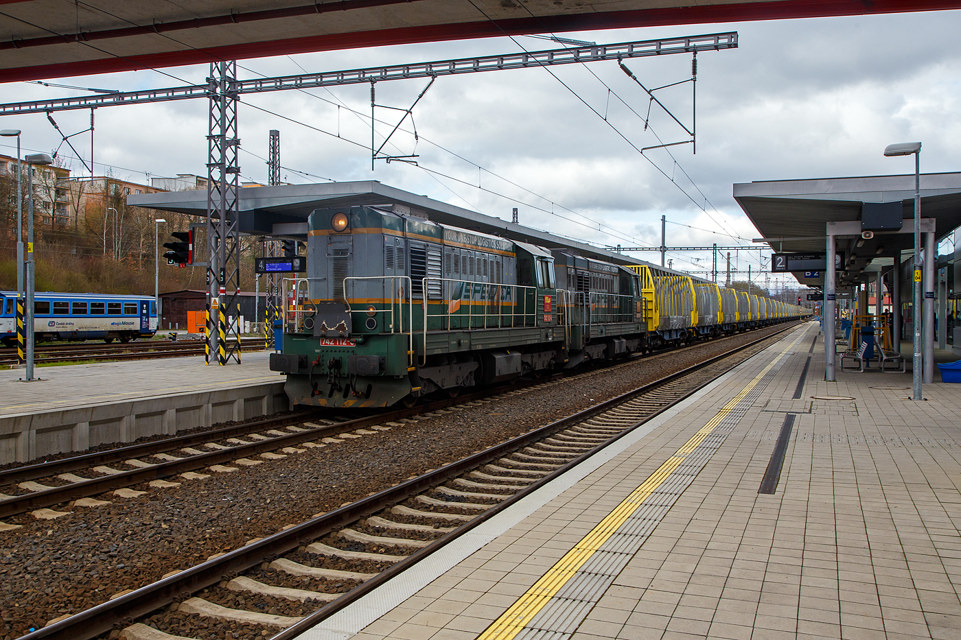 In Doppeltraktion fahren die beiden  Tranzisto  (Transistor), 742 112-6 und 742 205-8 der RM LINES a.s. (Sokolov), mit einem leeren sehr langen Holzzug (Wagen der Gattung Sggmrrs der �sterreichischen Innofreight Speditions GmbH, wobei eingestellt in Deutschland), am 17.04.2023 durch den Bahnhof Karlovy Vary (Karlsbad).

Der Eisenbahn-Verkehr des tschechischen Spedition und Logistik-Unternehmens SPEDICA s.r.o. mit Sitz in Sokolov wird vom dem Tochterunternehmen der RM LINES a.s. (RML) mit Sitz in Sokolov ausgef�hrt.

Die Diesellok  Kocour   oder  Tranzisto   (Kater, Transistor):
Die ČSD-Baureihe T 466.2, ab 1988 Baureihe 742 sind dieselelektrische G�terzug- und Rangierlokomotiven der ehemaligen Tschechoslowakischen Staatsbahn (ČSD). Die Entwicklung begann 1970 mit den beiden Prototypen der BR T 475.15 (744.5). 

Das Leistungswachstum in der Motortraktion sowie die Notwendigkeit von Fortschritten bei der Erneuerung der Dampftraktion und der k�nftigen Typenvereinheitlichung des Motorlokparks veranlassten das Verkehrsministerium, die Beauftragung der Entwicklung und anschlie�enden Produktion einer neuen Lokomotive zu pr�fen. Diese sollte f�r mittelschweren bis schweren Rangierdienst, leichteren Gleisdienst, aber auch im G�ter- und Personenverkehr, bestimmt sein.

Zwei Prototyp-Lokomotiven der Reihe T 475.15 (744.5) wurden 1970 von ČKD in Praha gebaut, wurden aber von der ČSD als ungen�gend abgelehnt. Dies lag haupts�chlich an ihrem F�hrerstand,  w�hrend die ČSD einen Turmf�hrerstand mit guter Sicht verlangte, hatten diese Lokomotiven einen F�hrerstand neben dem hinteren Ende der Lokomotive, sodass die Aussicht nicht sehr zufriedenstellend war. Die Maschinen der Baureihe T 475.15 wurden daher verworfen und stattdessen die neuen Lokomotiven der Baureihe T 466.0 (735) produziert. Die Produktion erfolgte ab 1972 im Turčiansk� stroj�rny in Martin. 1973 begann bei ČKD Prag die Produktion neuer Lokomotiven der Reihe T 448.05 (740.5), die f�r den Bedarf gro�er Industrieunternehmen und f�r den Export bestimmt waren. Die Produktion von Lokomotiven T 466.0 (735) bei TS Martin verz�gerte sich noch, die Entwicklung von Lokomotiven der Baureihe T 466.1 blieb erfolglos, au�erdem war geplant, die Produktion von Lokomotiven bei TS Martin einzustellen und das Werk auf die Waffenproduktion zu konzentrieren . Auch die bereits produzierten T 466.0 (735) Maschinen waren im Betrieb sehr unzuverl�ssig. Die Situation in der Flotte der ČSD-Motorlokomotiven ist daher unertr�glich geworden. Deshalb hat sich die ČSD eine Notl�sung einfallen lassen: 1976 bestellten sie bei der ČKD 60 neue Lokomotiven der Baureihe T 466.2 (742), die genau aus den Industriemaschinen der T 448.05 (740.5) entstehen sollten. Die Serie, die bereits seit drei Jahren in der Industrie im Einsatz war, mit zudem sehr guten Ergebnissen. Die Liste der erforderlichen Umbauten war recht lang: Gewichtsreduzierung, Umbau des Triebwerks, Einbau einer Zugsicherung, Umbauten im elektrischen Teil, Umbau der Bremsen.1977-78 wurden 60 Lokomotiven der 1. Serie gebaut geliefert und die neuen Maschinen wurden fast sofort auf CSD in Betrieb genommen. Die 2. Serie folgte sofort und eine weitere danach. Die Produktion der Lokomotiven T 466.2 (742) f�r die ČSD endete mit der 9. Serien im Jahr 1986; insgesamt erwarb ČSD 453 dieser Lokomotiven. W�hrend der langj�hrigen Produktion gab es mehrere partielle 

Modifikationen an der Konstruktion der Maschine – ab der 2. Serie mehrgliedrige Lenkung und Zugkraftw�hler, ab der 3. Serie eine Knickbr�cke seitlich am k�rzeren Vorbau, ab der 6. Serie wurden Jalousien auf dem Dach der Lokomotive installiert und ab der 7. Serie neue Fahrmotoren. 41 Lokomotiven wurden f�r den Bedarf der Industrie geliefert, Maschinen auf Basis der Baureihe T 466.0 ČSD wurden auch nach Vietnam und Bangladesch geliefert. Nach der Produktion von Lokomotiven T 466.2 (742) f�r ČSD erfolgte 1987-88 die Produktion von abgeleiteten Lokomotiven T 466.3 (743) f�r Adh�sionsbetrieb auf Steilstrecken.

TECHNISCHE DATEN der BR 742, ex T 466.2:
Hersteller: ČKD Praha
Baujahre: 1977 bis 1986
Hergestellt e Anzahl: 453 f�r die ČSD (in 9 Serien), 41 weiter f�r andere
Spurweite: 1.435 mm (Normalspur)
Achsfolge: Bo'Bo'
L�nge �ber Puffer: 13.580 mm ( am 4. Serie13.600 mm)
H�he: 4.472 mm
Breite: 3 130 mm
Drehzapfenabstand: 6.700 mm
Achsabstand im Drehgestell: 2.400 mm
Treibrad-�: 1.000 mm (neu) / 920 mm (abgenutzt) 
Dieselmotor: 6-Zylinder-Viertakt-Reihen- Dieselmotor mit Direkt-Einspritzung und Turbolader vom Typ ČKD  K 6 S 230 DR
Motorhubraum: 64,75 Liter (Zylinder-� 230 mm / Kolbenhub 260 mm)
Kompressionsverh�ltnis: 12,5 : 1
Nenndrehzahl: 1.250 U/min (Leerlaufdrehzahl 510 U/min)
Motorgewicht (ohne Generator): 7.700 kg
Achs�bersetzung: 1:4,8125
Dauermotorleistung: 883 kW (1.200 PS)
Leistung des Traktionsgenerators: 780 kVA
Leistungs�bertragung: dieselelektrisch
Fahrmotorentyp: TE 005 E / ab 7. Serie TE 015 C
Antriebsmotorleistung: 195 kVA
H�chstgeschwindigkeit: 90 km/h
Dienstgewicht: 64 t
Anfahrzugkraft: 192kN
Dauerzugkraft: 121 kN
Max. Tankinhalt: 4.000 l
Kleinster bef. Halbmesser: R 80 m

Quellen: SPEDICA s.r.o., Wikipedia, atlaslokomotiv.net