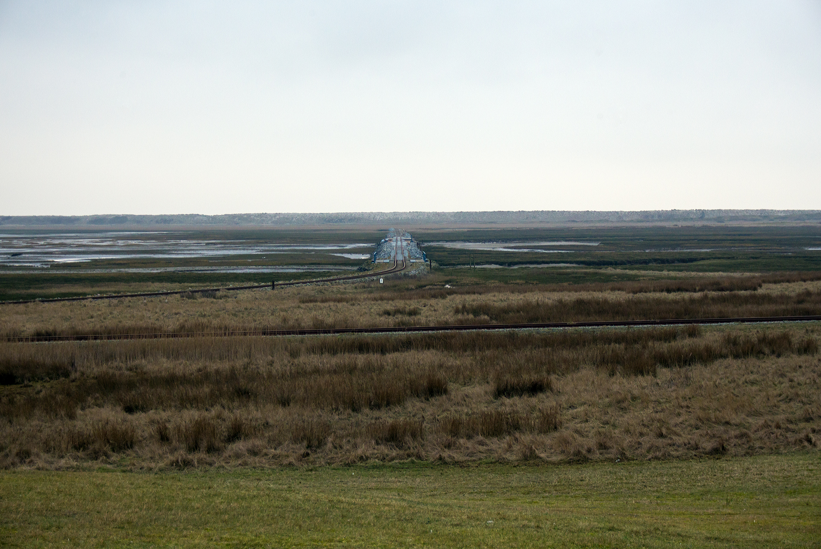 Inselbahn Wangerooge beim Abzweig Wangerooge Saline (vom Deich gesehen) am 12 März 2024. 

Geradeaus in der Bildmitte die Strecke auf dem Steindamm in den Salzwiesen zum Westanleger Wangerooge, mit einer Länge von rund vier Kilometern verbindet die Inselbahn den Ort Wangerooge mit dem Westanleger. Hier auf halber Strecke führt das Gleis über einen Priel. Mehrere Eisenbahnbrücken ermöglichen den Tidefluss (auf- und abfließen Gezeiten) im Priel zwischen der Salinenbucht und der Westlagune. 

Vorne (von links nach rechts) die Stichbahn/Strecke Wangerooge Saline zu Wangerooge Westen. 

Die Inselbahn Wangerooge ist die einzige von der Deutschen Bahn betriebene Schmalspurbahn und das wichtigste Verkehrsmittel auf der autofreien Insel. Sie ist auch eine der letzten Schmalspurbahnen Deutschlands mit Güterverkehr. Sie ist die einzige deutsche Inselbahn mit einer Zweigstrecke.
