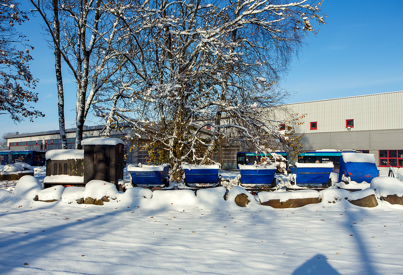 Kleiner 600mm Feldbahn-Kipplore-Zug „ganz groß“ als Denkmal beim Betriebshof der Westerwaldbahn (WEBA), hier am ersten Advent dem 03 Dezember 2023 auf der Bindweide bei Steinebach/Sieg.

Vorne eine 600mm DIEMA Feldbahnlok (Typ und Baujahr sind mir unbekannt), dahinter 5 Kipploren. 

Für den Laien ist alles, was auf der Feldbahn gezogen wird eine Lore. Tatsächlich bezieht sich dieser Ausdruck auf die wohl am weitesten verbreitete Wagenform - eine einfaches Rahmengestell mit zwei Achsen, Pilzkopfkupplungen und kippbarer Mulde. Die Mulden gab es in schmaler Bauform für den beengten Tiefbaubetrieb (Untertage-Bergbau), in breiter Bauform für die Tagebaue, Steinbrüche, Fabrikanlagen, usw.. In dieser Form war dieser Wagentyp in 100.000 und mehr Exemplaren weltweit im Einsatz. Von der Westerwälder Tongrube bis zum Bau der Autobahnen. In den Ausführungen zeigte sich eine kaum zu überblickende Vielfalt.

Diese Kipplore ist in der Bauart Eluco Record, in geschweißter Ausführung: Mulde aus Stahlblech, Abrollwiegen, Schlagleisten und Untergestell aus Profilstahl.
