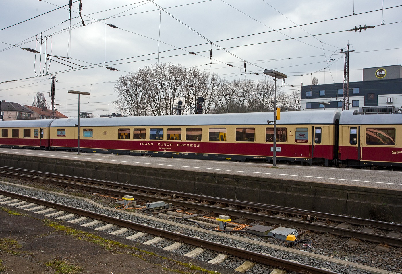 Klimatisierter 1. Klasse Halbspeisewagen der Gattung/Bauart ARmh 217, D-AKE 56 80 85-92 151-4, der AKE-Eisenbahntouristik – J�rg Petry e.K. (Gerolstein) am 10 M�rz 2024 im Hbf Osnabr�ck, eingereiht im Zugverband in den 1. Klasse-Sonderzug AKE RHEINGOLD (vom 10 bis 14 M�rz 2024) von Koblenz via Hamburg, Bremen, Husum und Westerland auf Sylt nach List auf Sylt. 

Der Wagen wurde 1969 von Waggonfabrik Wegmann & Co. in Kassel gebaut und als D-DB 51 80 84-80 251-2 AR�mh 217 an die Deutschen Bundesbahn geliefert. Im Jahr 2006 wurde er an Regentalbahn verkauft, wo er als 56 80 85-92 151-4 D-RBG BRmh gef�hrt wurde, 2013 ging er an die Pressnitztalbahn, neue Nummer 56 80 85-92 151-4 D-PRESS ARmh 217 und 2015 wurde er an die Vulkaneifel-Bahn wo er nun wieder die Bezeichnung 56 80 85-92 151-4 D-AKE ARmh 217 f�hrt.

Allgemeines zu den Halbspeisewagen:
Die Deutsche Bundesbahn f�hrte ab 1966 f�r die damaligen F-Z�ge Halbspeisewagen der Typen Armz 211, ARmh 217 und Armz 218 ein. Diese Wagen mit einer L�nge von 27,5 m bestehen aus einer K�che, dem Speiseraum und Sitzabteilen der 1. Klasse. Die Wagen waren zun�chst in innerdeutschen und internationalen F-, D- und TEE-Z�gen im Einsatz. Ab September 1971 kam auch der neu eingerichtete IC-Verkehr hinzu. Die Einstiege mit Drehfaltt�ren befinden sich an einem Wagenende. Dort sind auch die Toilette und eine Kofferablage installiert. Es folgt ein Gro�raum 1. Klasse mit 18 Pl�tzen, bestehend aus Einzelsitzen und zus�tzlichen Esstischen. Im anschlie�enden Speiseraum k�nnen Reisende an 30 Pl�tzen bedient werden. Somit verf�gt der Wagen insgesamt �ber 48 Sitzpl�tze. Der Wirtschaftsbereich besteht aus B�fett, K�che und Sp�lraum. Die Wagen wurden mit gasbeheizten Herden oder Elektroherden ausgestattet. Je eine Schiebet�r in den Seitenw�nden im Bereich der K�che dient zum Beladen des Fahrzeugs. Der ARmh 217 besitzt seit 1990 eine RIC-Zulassung f�r 200 km/h (f�r viele L�nder). Daher kommt der Wagen vornehmlich bei den Fahrten mit dem historischen TEE-Rheingold zum Einsatz. Die vorhandene Dampfheizung erm�glicht aber auch Eins�tze bei Dampfsonderfahrten.

TECHNISCHE DATEN:
L�nge �ber Puffer: 27.500 mm
Wagenkastenl�nge: 27.200 mm
Wagenkastenbreite: 2.805 mm
H�he �ber Schienenoberkante: 4.050 mm
Drehzapfenabstand: 19.500 mm
Achsstand im Drehgestell: 2.500 mm
Drehgestellbauart: Minden-Deutz 367
Leergewicht: 51 t
H�chstgeschwindigkeit: 200 km/h (bei Ablieferung 160 km/h bis 1990)
Sitzpl�tze: 18  im 1. Klasse Gro�raum / 30 im Speiseraum
Heizungsbauart: Klimae
Energieversorgung: Zentrale Energieversorgung aus der Zugsammelschiene

Die Geschichte von diesem TEE/IC-Halbspeisewagen ARmh 217  D-AKE 56 80 85-92 151-4 (Quelle AKE Rheingold):
Der Wagen wurde von der Waggonfabrik Wegmann & Co. in Kassel gebaut und am 17.04.1969 mit der Wagennummer 51 80 84-80 251-2 in Dienst gestellt. Er geh�rte zu einer Gruppe von 25 Wagen, die in vier Serien zwischen 1966 und 1970 geliefert wurden. Ihre zul�ssige H�chstgeschwindigkeit betrug damals160 km/h.

Diese Bauart wird als „Halbspeisewagen“ bezeichnet, weil sie im Gegensatz zu den „Vollspeisewagen“ einen verkleinerten Restaurant- und Wirtschaftsteil besitzt. Daf�r wurde in der vorderen Wagenh�lfte ein 1. Klasse-Gro�raum vorgesehen, der bei Bedarf als weiterer Speiseraum hergerichtet werden kann.

Alle Wagen hatten zu Beginn eine Lackierung in blau f�r die 1. Klasse bzw. rot f�r den Speisewagen-Bereich, was ihnen bald den Spitznamen „Kakadu“ einbrachte. W�hrend die meisten dieser Fahrzeuge ab 1971 in die TEE-Farben beige/rot umlackiert wurden, behielt dieser Wagen sein urspr�ngliches Farbkleid noch bis 1983.

Im Gegensatz zu den anderen vollelektrischen Speisewagen wird hier auf einem Gasherd gekocht, wegen des hohen Stromverbrauchs konnte auch keine elektrische Geschirrsp�lmaschine eingebaut werden. Daf�r kann der Wagen aufgrund seiner weitgehend autarken Energieversorgung in allen europ�ischen Bahnstromsystemen eingesetzt und auch problemlos von einer Dampflok bef�rdert werden.

Sein Einsatzgebiet war dadurch �u�erst vielf�ltig, zun�chst in Fernschnellz�gen, ab 1971 im neuen, damals noch erstklassigen IC-Netz. Hinzu kamen TEE-Z�ge, hochwertige nationale und internationale Schnellz�ge, Autoreisezug-Dienste, Sonderz�ge zur Hannover-Messe und bis 1989/90 einige Transitz�ge zwischen der Bundesrepublik und Berlin (West). Dieser  Wagen war u.a. in Amsterdam, Br�ssel, Paris, Strasbourg und Mailand anzutreffen, lief im legend�ren „Orient-Express“ nach Wien und f�hlte sich auch an der franz�sischen Atlantik- und Mittelmeerk�ste wohl.

1983 wurde er grundlegend aufgearbeitet und erhielt dabei u.a. neue Fenster, die mit besserer Abdichtung vor Korrosion sch�tzten, neue Sitzbez�ge, stabilere Tische im Gro�raum 1. Klasse und auch eine Lackierung in den TEE-Farben. 1991 erfolgte ein Anstrich in den neuen IC-Produktfarben orientrot mit pastellviolettem Absetzstreifen, dann erhielt er die verkehrsrote Farbgebung und auch das ICE-Farbkleid erlebte er 2002 noch.

Ab 1990 war der Wagen f�r eine H�chstgeschwindigkeit von 200 km/h zugelassen. 1999 wurde eine neue K�che eingebaut, die Sitze im Speise- und Gro�raum erhielten einen Polsterstoff in gediegenem Blau. Zuletzt lief er im EC „Wawel“ zwischen Hamburg und Breslau. Im Dezember 2005 wurde dieser Wagen bei der DB AG ausgemustert, erhielt anschlie�end seine „Kakadu“-Lackierung zur�ck und wurde fortan von der Regentalbahn AG in den bayerischen ALEX-Z�gen eingesetzt. Ab 2008 lief er bei der Pressnitztalbahn GmbH �berwiegend in Sonderz�gen, wurde aber von Dezember 2009 bis M�rz 2010 auch f�r den Eurobahn-Ersatzverkehr des RE 13 zwischen Hamm und
M�nchengladbach verwendet.

2012 wurde dieser Wagen von der Vulkan-Eifel-Bahn �bernommen, 2015 wieder in den TEE-Farben lackiert und ist seitdem in den Wagenpark des historischen „Rheingold“ der AKE-Eisenbahntouristik eingestellt.
