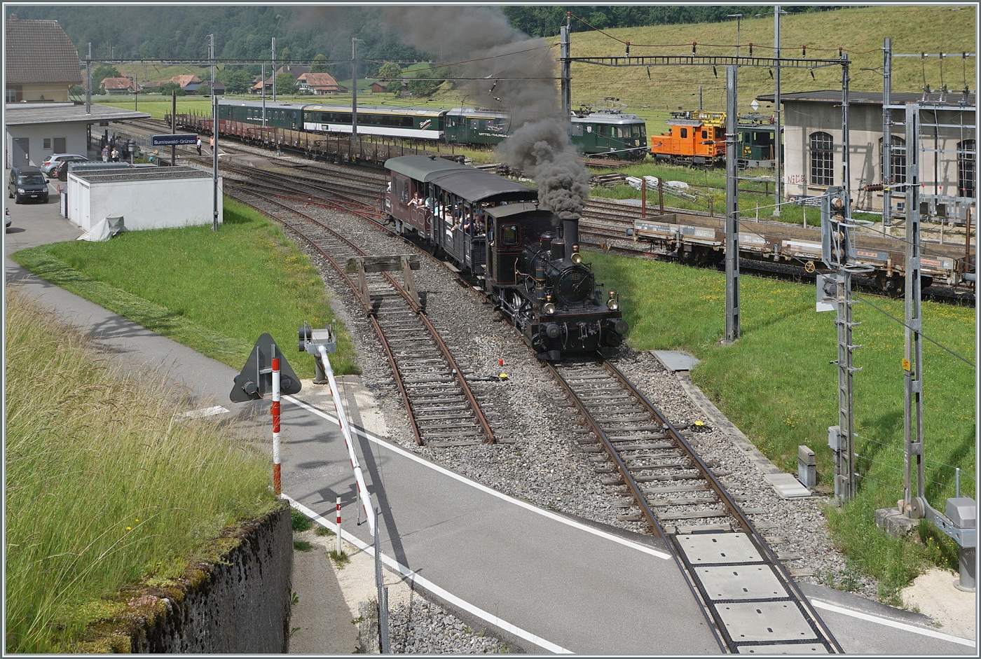 Mit einem Dampfzug der  Emmentalbahn  verlässt die E 3/3 853 (UIC 90 85 0008 573-3) den Bahnhof von Sumiswald-Grünen mit dem Ziel Wasen im Emmental. Im Hintergrund ist der VH-MThB ABe 4/4  N° 12 mit Bodan-Salon-Wagen und dem VH-MThB BDt zu sehen, der vor einer guten halben Stunde Sumiswald erreicht hat. 
Zudem wird in Kürze der OeBB Dampfzug aus Balsthal in Sumiswald eintreffen. 
Kurz zusammengefasst: heute findet der Gotthelf-Märit in Sumiswald statt. 

14. Juni 2025