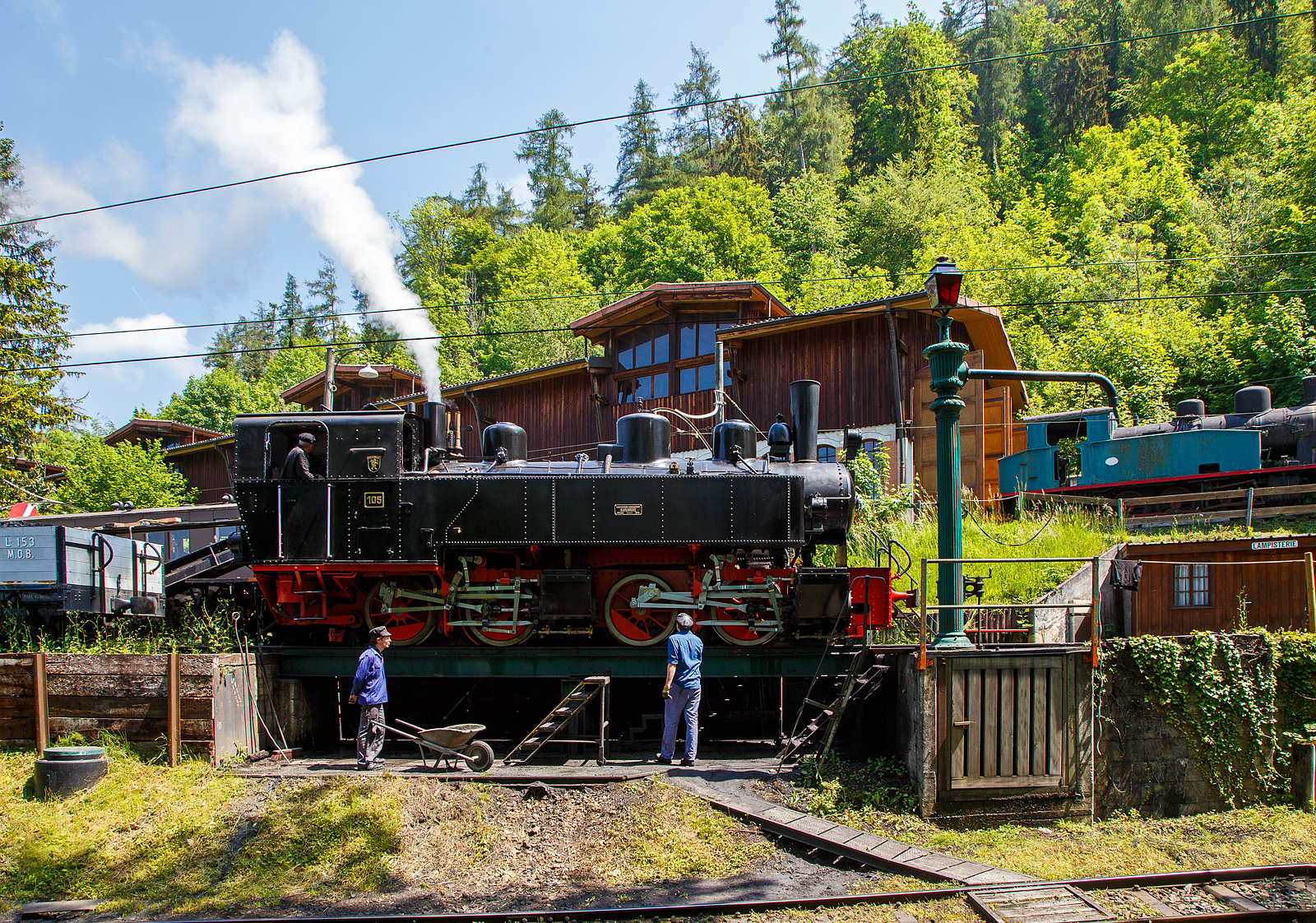 Museumsbahn-Romantik pur – Pfingsten 2023 (Samstag 27. bis Montag 29. Mai 2023) fand bei der Museumsbahn Blonay–Chamby das Schweizer Dampffestival 2023 / Festival suisse de la Vapeur 2023 statt.

Bei der Dampflok-Wartungsstelle der Museumsbahn Blonay–Chamby beim Museumsareal in Chaulin steht am 27. Mai 2023 die G 2x2/2 Mallet-Dampflok 105  Todtnau  der Museumsbahn Blonay–Chamby, ex SEG 105  Todtnau .  Links die Strecke hinab nach Blonay, rechts das Stichgleis zum Museum bzw. Depot.

Für den Einsatz auf den Meterspur-Strecken in Frankreich bestellten die Deutschen Heeresfeldbahnen bei der Maschinenbau-Gesellschaft Karlsruhe sieben Mallet-Dampflokomotiven. Aus Zeitgründen wurde keine zeitgemäße neue Serie entwickelt. Man nahm alte Konstruktionsunterlagen als Grundlage. Die Auslieferung erfolgte im August 1918. Bevor die Maschinen HK 94 bis HK 100 (HK = Heeresprüfkommission für Feldbahnen) ihren Einsatzort erreichten, war der I. Weltkrieg (Waffenstillstand von Compiegné am 11. November 1918) jedoch schon beendet. Da sie nicht mehr von den Heeresfeldbahnen benötigt und nicht zum Reparationsgut zugeordnet wurden, übernahm sie das Reichsverwaltungsamt. Dieses verkaufte in den Jahren 1919/1920 die Loks.

Die Lok wurde 1918 von der Maschinenbau-Gesellschaft Karlsruhe unter der Fabriknummer 2051gebaut und von der Heeresprüfkommission für Schmalspurbahnen abgenommen als Lok „HK 95“ abgenommen, wegen dem Kriegsende kam sie auf den Heeresfeldbahnen nicht mehr zum Einsatz. So wurde sie 1919 an die Kleinbahn Voerde-Haspe–Breckerfeld als HVB 28 verkauft. Die Kleinbahn Voerde-Haspe–Breckerfeld wurde elektrifiziert, und die  Nr. 28  wurde 1925 an die Zell-Todtnau-Eisenbahn (in der Nähe von Freiburg) der Süddeutsche Eisenbahn-Gesellschaft (SEG) abgegeben, wo sie die  Nummer 105  -  Todtnau  erhielt. Sie blieb bis zur Streckenstillegung der Linie im Jahre 1968 im Schwarzwald und ging gleich drauf an die Museumsbahn Blonay – Champy.
Es ist noch eine Schwesterlok erhalten geblieben, es ist die 99 5906 der HSB.

Konstruktion:
Das hintere Triebwerk mit den Hochdruckzylindern ist fest im Blechrahmen gelagert. Das vordere Triebwerk mit den Niederdruckzylindern ist mit einem Königszapfen mit dem hinteren Triebwerk verbunden, der genietete Kessel liegt mit Gleitplatten auf ihm auf. Seitliche Blattfedern halten das Triebwerk in einer mittigen Stellung. Beide Triebwerke haben einen Innenrahmen.

Der Dampf wird erst zu den hinteren Zylindern geleitet, von dort gelangt er über flexible Leitungen in die vorderen Zylinder. Alle Zylinder verfügen über Flachschieber und außenliegende Heusinger-Steuerung mit Hängeeisen. Die Loks verfügen über eine Wurfhebel-Handbremse und eine Dampfbremse als Zusatzbremse. Je nach Bahn wurden später Saugluft- oder Druckluftbremse als Zugbremse nachgerüstet. Auf dem Kessel sitzen zwei Sanddome, einer für jedes Triebwerk.

TECHNISCHE DATEN:
Hersteller Maschinenbau-Gesellschaft Karlsruhe (MBK)
Baujahr: 1918
Betriebsgattung: K 44.9
Kurzbezeichnung: B' B n4vt
Spurweite: 1.000 mm
Kurzbezeichnung: B' B n4vt
Länge über Puffer: 9.400 mm
Höhe über SO: 3.800 mm
Achsstand im Triebwerk: 1.400 mm
Treibraddurchmesser: 1.000 mm
Leergewicht: 28,5 t
Dienstgewicht: 34,4 t
Höchstgeschwindigkeit: 30 km/h
indizierte Leistung: 200 kW (270 PS)
Anfahrzugkraft: 47,76 kN
kleinster befahrbarer Gleisbogen: 50 m
Kesselüberdruck: 12 bar
Kohlevorrat : 1,1 t
Wasservorrat: 3,6 m³
Zylinderanzahl: 4
Zylinderdurchmesser: 280 mm (HD) / 425 mm (ND)
Kolbenhub: 500 mm
Bremse: Knorrbremse m. Z., Wurfhebel-Handbremse

Geschichte der Mallet-Lokomotiven:
Der zunehmende Verkehr auf schmalspurigen Eisenbahnen erschloss Mallet ein anderes Wirkungsfeld. Diese Bahnen benötigten stärkere und damit größere Maschinen, als es die engen Kurven der Schmalspurstrecken zuließen. Die einzige Lösung schienen hier Lokomotiven mit schwenkbaren Fahrwerken zu sein. Dazu waren bereits die Bauarten von Fairlie und Meyer verbreitet, die schwenkbare Maschineneinheiten verwendeten. Die einzelnen Einheiten wurden mit Dampf über flexible Verbindungen gespeist, die sich jedoch stets als Schwachpunkt der Maschinen erwiesen. Mallet entwickelte stattdessen eine Bauart mit zwei Fahrwerken, von denen nur das vordere, unter der Rauchkammer befindliche Fahrwerk schwenkbar gelagert war, während der Kessel fest auf dem anderen Fahrwerk ruhte. Damit reduzierte sich die Zahl der flexiblen Verbindungen um die Hälfte. Der wesentliche Unterschied der Konstruktion von Mallet im Vergleich zu den Bauarten Fairlie und Meyer war aber die perfekte Anwendung eines Verbundtriebwerkes. Der Frischdampf wird zunächst zu den Hochdruckzylindern des fest gelagerten Fahrwerks geleitet und nach dem Auslass in die Niederdruckzylinder des vorderen beweglichen Fahrwerks. Die dorthin führende bewegliche Dampfleitungsverbindung war wegen des geringeren Drucks besser beherrschbar als bei reiner Frischdampf-Versorgung. Diese Bauart ließ Mallet sich 1884 patentieren.

Dampflokomotiven haben im Allgemeinen zwei Arbeitszylinder, die Mallet-Loks besitzen diese Einrichtungen doppelt, also 4 Zylinder mit zugehörigen Triebwerksgruppen. Der Abdampf der ersten ist gleichzeitig der Arbeitsdampf der zweiten Zylindergruppe.

Schweizerische Bauartbezeichnung G2 x 2/2, Deutsche Reichsbahn Baureihe 99.590

Mallet-Lokomotive B'B n4vt
- B'B = Dampflokomotive mit 2 Triebwerken, das erste davon beweglich gelagert, zu je 2 Treibachsen
- n4 = Naßdampf und 4 Zylinder
- v = Verbundwirkung zwischen den Hoch- und Niederdruck-Zylindern
- t = Brennstoff und Wasservorräte werden auf der Lokomotive mitgeführt
- (in neuerer Schreibweise wird häufig das  t  weggelassen.
- Bei Angaben ohne  t  handelt es sich dann immer um eine Tenderlok, im Gegensatz dazu  T  = Schlepptenderlok).