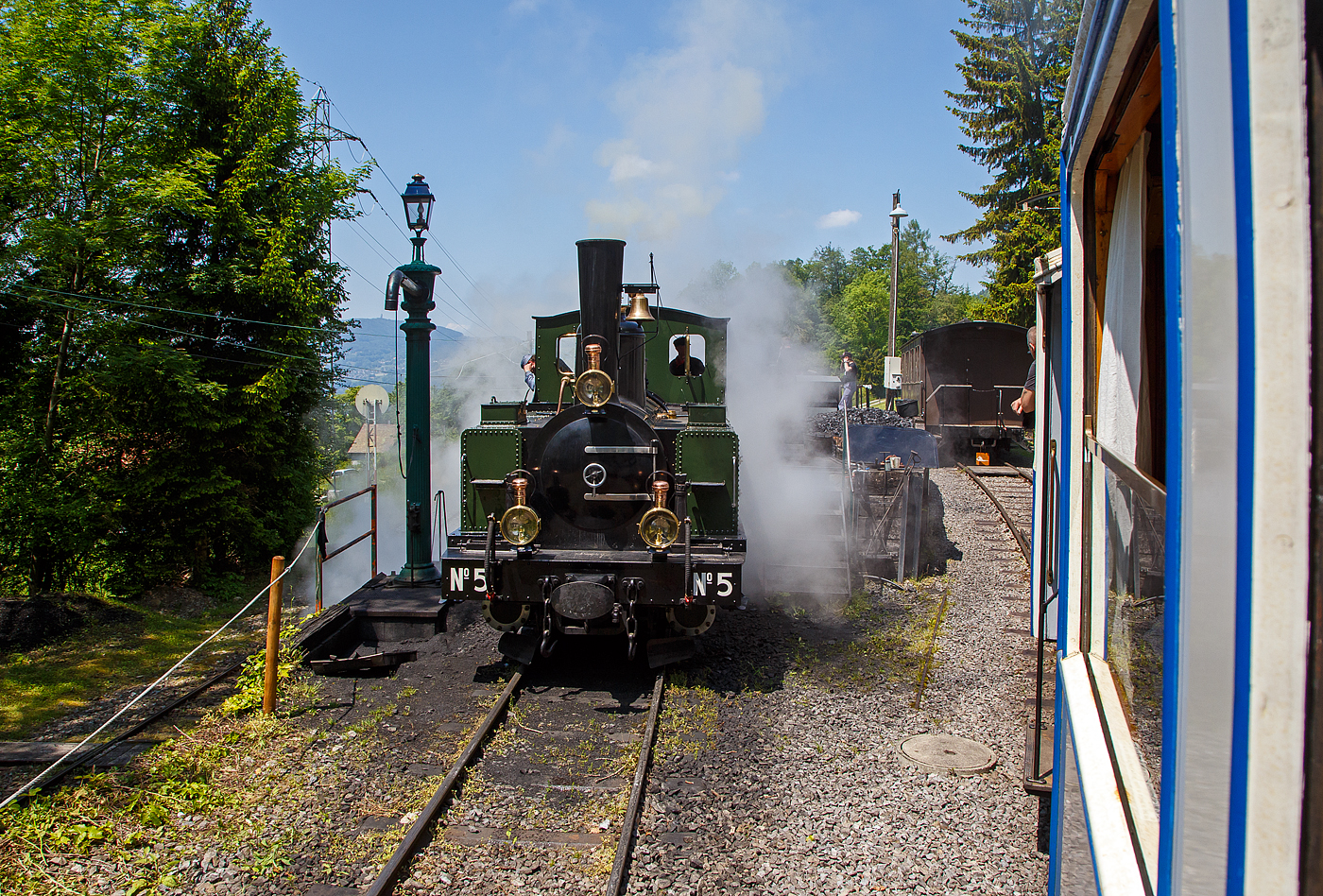 Museumsbahn-Romantik pur – Pfingsten 2023 (Samstag 27. bis Montag 29. Mai 2023) fand bei der Museumsbahn Blonay–Chamby das Schweizer Dampffestival 2023 / Festival suisse de la Vapeur 2023 statt.

Bei der Dampflok-Wartungsstelle der Museumsbahn Blonay–Chamby beim Museumsareal in Chaulin steht am 27.05. 2023 die G 3/3 LEB N° 5  Bercher  der Museumsbahn zum Kohlefassen. Links die Strecke 115 der MVR hinab nach Blonay, wir fahren mit dem ex MOB BCFe 4/4 11 rechts das Stichgleis zum Museum bzw. Depot hinauf.

Die ex LEB Nr. 5  Bercher  (Lausanne–Echallens–Bercher-Bahn) wurde 1890 von der Elsässische Maschinenbau-Gesellschaft Grafenstaden (später Société Alsacienne de Constructions Mécaniques) unter der Fabriknummer 4172 gebaut und an die Lausanne–Echallens–Bercher-Bahn geliefert. Die EMBG hatte auch zwei Jahre zuvor die baugleiche Nr. 2 geliefert. Die beiden dreiachsigen Tenderlokomotiven trugen die Hauptlast des Verkehrs, bis in den Jahren 1903 und 1905 zwei baugleichen Tenderlokomotiven, die G 3/3 6 „Gros-de-Vaud“ und G 3/3 7 „Talent „durch die Schweizerische Lokomotiv- und Maschinenfabrik (SLM) in Winterthur abgeliefert wurden. 

Von der YSteC konnte die LEB 1920/1921 die drei 1893 ebenfalls durch die EMBG gebauten Mallet-Lokomotiven G 2x2/2 Nr. 1 bis 3 gebraucht übernehmen. Nun waren die G 3/3 Nr. 2 und 5 nicht mehr gefragt. Während die G 3/3 2 „Échallens“ bereits 1929 verschrottet wurde (seit 1920 war sie bereits abgestellt), die G 3/3 Nr. 5  Bercher  hatte es da etwas besser, sie wurde 1934 an die Firma Energie de l’Ouest Suisse (EOS) für die Baustelle der Staumauer Grande-Dixence verkauf. Nach dem die Arbeiten 1935 erledigt sind geht sie bei der EOS außer Betrieb. Im Jahr 1939 verlässt die Schweiz und geht nach Vorarlberg in Österreich, zu einer Baufirma. Die Baufirma verschenkte 1967 die Lok und sie wurde, wie viele andere Dampflokomotiven zu dieser Zeit, auf einem Kinderspielplatz in der Stadt Feldkirch aufgestellt. Das Ausstellungsobjekt weckte die Aufmerksamkeit einiger Mitarbeiter der Museumsbahn Blonay–Chamby (BC), denen es gelang 1973 diese Lokomotive im Tausch gegen eine andere Lok zu erwerben.

Nach einer Aufarbeitung war die Lokomotive 1985 bis 2005 in Betrieb. Dann musste sie abgestellt werden. 2013/2014 wurde die Lokomotive ein zweites Mal durch die Museumseisenbahner aufgearbeitet. Seit dem Frühling 2015 ist die zweitälteste Schmalspur-Dampflokomotive der Schweiz, die älteste ist die G 3/4 1 „Rhätia  der Rhätischen Bahn (RhB), nach dem Abschluss der Revisionsarbeiten wieder in Betrieb.

TECHNISCHE DATEN der LEB G 3/3 N° 5  Bercher :
Baujahr: 1890
Spurweite: 1.000 mm
Achsformel: C
Länge über Puffer: 6.830 mm
Achsabstand: 1.800 mm (950mm / 850 mm)
Dienstgewicht: 20,4 t
Anzahl der Zylinder: 2
Zylindergröße: Ø 270 mm x 370 mm Kolbenhub
Treibraddurchmesser: 810 mm
Höchstgeschwindigkeit: 25 km/h
Stundenleistung: 150 PS
Kesselüberdruck: 12 bar
Kohlevorrat: 0,8 t
Wasservorrat: 2,2 m³

Die Lausanne–Echallens–Bercher-Bahn, abgekürzt LEB, französisch Chemin de fer Lausanne–Echallens–Bercher, ist eine meterspurige Privatbahn. Die knapp 24 Kilometer lange Strecke führt vom Stadtzentrum von Lausanne (Flon) durch die nördlichen Vororte und weiter nach Echallens und Bercher im Gros de Vaud, dem Waadtländer Hinterland. Die LEB ist eine moderne Vorortbahn, die in Lausanne teilweise unterirdisch verkehrt. Die Züge fahren alle 30 Minuten (zwischen Echallens und Bercher gibt es einige wenige Taktlücken am Vormittag). Werktags wird ein Viertelstundentakt bis Cheseaux angeboten. Von Montag bis Freitag verkehren in Lastrichtung einige beschleunigte Hauptverkehrszüge.
