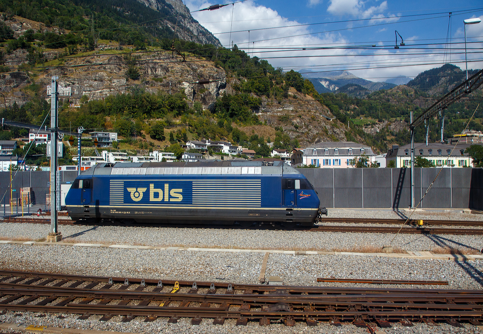 Noch im alten originalen Dunkelblau und somit noch nicht modernisiert, die BLS 465 002-4 „Görnergrat“ (91 85 4465 002-4 CH-BLS) seht am 08 September 2021 in Birg, aufgenommen aus einem IC.

Die BLS Re 465 stellen eine Weiterentwicklung der SBB Re 460 dar. Wie diese hat sie GTO-Thyristoren als Ventile im Stromrichter und Drehstrom-Asynchronmotoren. Der Unterschied liegt in der Umrichteranlage. Im Fall der Re 460 der SBB besteht ein Traktionsstromrichter (zwei je Lok, ein Gerät pro Drehgestell) aus zwei Vierquadrantenstellern die den Zwischenkreis parallel versorgen und einem Motor-Wechselrichter der zwei Motoren parallel speist. Die Stromrichter der BLS Re 465 gruppieren sich zu drei Vierquadrantenstellern parallel an einem Zwischenkreis mit zwei Wechselrichtern, je einen Motor im Drehgestell speisend. Somit lässt sich eine schleudernde Achse schneller und effektiver wieder in einen normalen Lauf bringen. Wurde bei der Entwicklung der Re 460 auf Dreipunkt-Stromrichter gesetzt, wurde im Gegensatz dazu die Re 465 mit Zweipunkt-Technik ausgestattet. Die Zwischenkreisspannung senkte man entsprechend von 3,5 kV (Re 460) auf 2,8 kV (Re 465). Zudem besitzt die Re 465 sechspolige Asynchron-Fahrmotoren, die Re 460 hingegen nur vierpolige Asynchronmotoren. Daraus resultiert eine gegenüber der Re 460 erhöhte Dauerleistung von 6.400 kW (Stundenleistung von 7000 kW). Die Radsätze im Drehgestell stellen sich radial zum Gleisbogen ein.

Zudem ist die Re 465 im Unterschied zur Re 460 mit der Vielfachsteuerung des Systems IIId und (mit Übergangskabel) BLS/BBC ausgerüstet. Dies erlaubt die Vielfachsteuerung zum Beispiel mit Re 4/4II, Re 4/4III, Re 6/6, Re 425 oder Ae 415.

In den Jahren 2019 bis 2022 wurden die Lokomotiven einem Refit unterzogen. Darin enthalten waren unter anderem der Einbau der Vielfachsteuerung ZMS für den Güterverkehr mit Traxx- und Vectron-Lokomotiven und ETB (Ethernet Train Backbone) für den Autoverlad am Lötschberg. Die Kästen wurden saniert und neu in hellem BLS-Lindengrün mit blauem Logo lackiert. Die Arbeiten wurden in der eigenen Werkstätte der BLS in Bönigen ausgeführt, die Kosten beliefen sich auf 20 Millionen Franken.