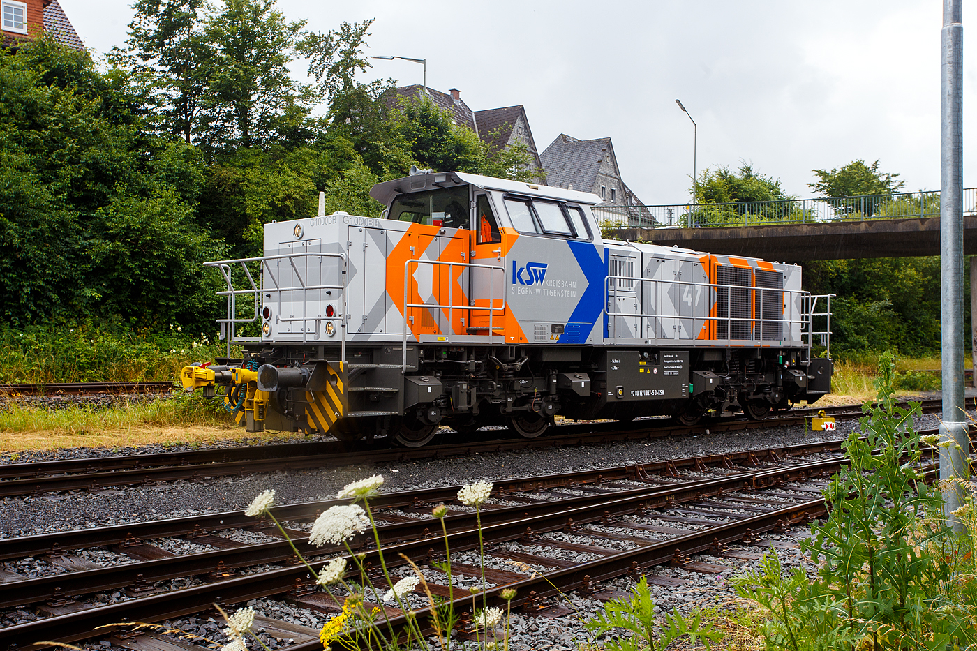 Nun auch im neuen Look/Outfit (Lackierung) die 
Die KSW 47 (92 80 1271 027-5 D-KSW), ex D 2 der HFM, eine Vossloh G 1000 BB der KSW (Kreisbahn Siegen-Wittgenstein), wartet am 03 Juli 2024 auf dem KSW-Rangierbahnhof in Herdorf der Betriebsstätte FGE -Freien Grunder Eisenbahn (KSW NE447 / DB-Nr. 9275). Die Lok ist hier mit Rangierkupplungen vom Typ RK 900 ausgestattet. 

Die Lok wurde 2008 unter der Fabriknummer 5001673 bei Vossloh in Kiel gebaut, 2009 ging sie zur kundenspezifische Anpassung zum Service-Zentrum Moers und erst am 16.07.2010 erfolgte die Auslieferung an HFM Managementgesellschaft für Hafen und Markt mbH in Frankfurt (Main)  D 2  (92 80 1271 027-5 D-HFM). Am 31.10.2016 ging sie dann an die Kreisbahn Siegen-Wittgenstein (KSW).

Die G 1000 ist eine vierachsige dieselhydraulische Lokomotive
für den schweren Rangier- und leichten Streckendienst. Die zuverlässige Vielzwecklokomotive ist mit modernster Technik ausgestattet und erfüllt daher die neuesten Vorschriften des Unfallschutzes. Die Anwendungsbreite der Lokomotive reicht vom leichten Rangierdienst in Einzeltraktion über den Einsatz als Streckenlokomotive in Mehrfachtraktion bis hin zum schweren Rangierdienst. 

Mit der MaK G 1000 BB wird seit dem Jahr 2002 eine Lok für den Leistungsbereich unterhalb der G 1206 angeboten. Sie basiert auf der G 800 BB, von der außer dem kompletten Fahrwerk und Rahmen auch das Führerhaus und der hintere Vorbau übernommen wurden. Deutlich anders ist dagegen der vordere Vorbau, in dem Platz für den größeren Dieselmotor geschaffen wurde.

TECHNISCHE DATEN:
Spurweite: 1435 mm (Normalspur)
Achsfolge: B´B´
Länge über Puffer: 14.130 mm
Drehzapfenabstand: 6.700 mm
Radsatzabstand im Drehgestell:  2.400 mm
Treibraddurchmesser: 1.000 mm (neu) / 920 mm (abgenutzt)
größte Breite:  3.080 mm
größte Höhe über Schienenoberkante:  4.225 mm
kleinster befahrbarer Gleisbogen:  60 m
Dienstgewicht: 80 t
Motorart: V8-Zylinder-Viertakt-Dieselmotor mit Common-Rail-Einspritzung, sowie mit Abgasturboaufladung und Ladeluftkühler
Motortyp: MTU 8V 4000 R41L
Leistung: 1.100 kW (1.475 PS)
Nenndrehzahl: 1.860 U/min
Motorabmessung (LxBxH): 1.915 x 1.380 x 1.800 mm
Motorgewicht (trocken): 4.700 kg
Bohrung x Hub / Motorhubraum: 165mm x 190 mm / 32,5 Liter
Strömungsgetriebe: Voith L4r4
Anfahrzugkraft: 259 kN
Höchstgeschwindigkeit:  100 km/h
Bremse: Radscheibenbremse (Knorr), auf alle Räder wirkend, hydrodynamische Bremse
Bremsgewichte G/P: 65 t/96 t
Kraftstoffvorrat:  3000 l
    
Seit 2002 wurden 103 G 1000 BB gebaut (Stand 01.01.2015).