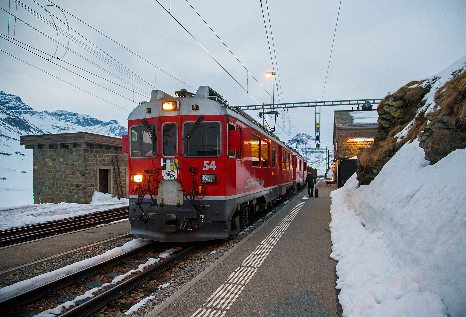 Nun haben die beiden RhB ABe 4/4 III Triebwagen 54  Hakone  und  51  Poschiavo  am 21.03.2023 als PmG (Personenzug mit G�terbef�rderung) nach Poschiavo, fahren nun vom h�chsten Punkt der Berninabahn, den Bahnhof Ospizio Bernina weiter nach Poschiavo.

Ab hier sind nun eher die Bremsen gefordert, denn nun geht es bis nach Poschiavo fast nur bergab. Von Pontresina nach Ospizio Bernina geht es nur bergauf, und wir merkten wie die Triebwagen arbeiten mussten.
