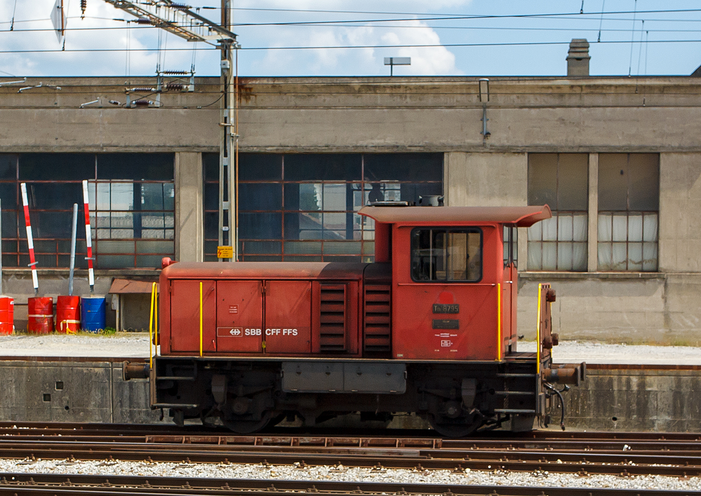 SBB Tm IV Diesellok (Rangiertraktor mit Dieselantrieb) Tm 8795 ist am 28.05.2012 in Bulle abgestellt. Der Index IV steht f�r die Leistungsklasse IV (�ber 350 PS). Das Bild entstand aus einem Zug heraus.

Die Lok wurde 1976 von der SLM (Schweizerische Lokomotiv- und Maschinenfabrik) in Winterthur unter der Fabriknummer 5074 gebaut und als Tm 8795 an die SBB - Schweizerische Bundesbahnen geliefert. Heute sieht der Rangiertraktor nicht mehr so aus, denn 2013 erfolgte im Industriewerk Biel der SBB ein Umbau, Einbau einer Funksteuerung und Remotorisierung, danach wurde sie ab November 2013 als SBB Tmf 232 306-1 (98 85 5 232 306-1 CH-SBBC) der SBB Cargo AG gef�hrt.

Die Fahrzeuge wurden als fahrdrahtunabh�ngiges Fahrzeug f�r den Rangier- und Baudienst beschafft. Erstmals bei einer gro�en SBB-Fahrzeugserie, kam bei diesen Fahrzeugen die hydraulische Kraft�bertragung zum Einsatz. Da das Turbowendegetriebe eine Ausr�stung f�r beide Fahrtrichtungen hatte, konnte auf das st�rungsanf�llige mechanische Wendegetriebe verzichtet werden. Um die ung�nstige Wirkungsgradcharakteristik abzuschw�chen, wurde ein nur im Stillstand schaltbares Stufengetriebe eingebaut, das die Wahl zwischen einer H�chstgeschwindigkeit von 30 oder 60 km/h, oder die Wahl zwischen gr��erer Zugkraft oder gr��erer Geschwindigkeit erm�glichte.
