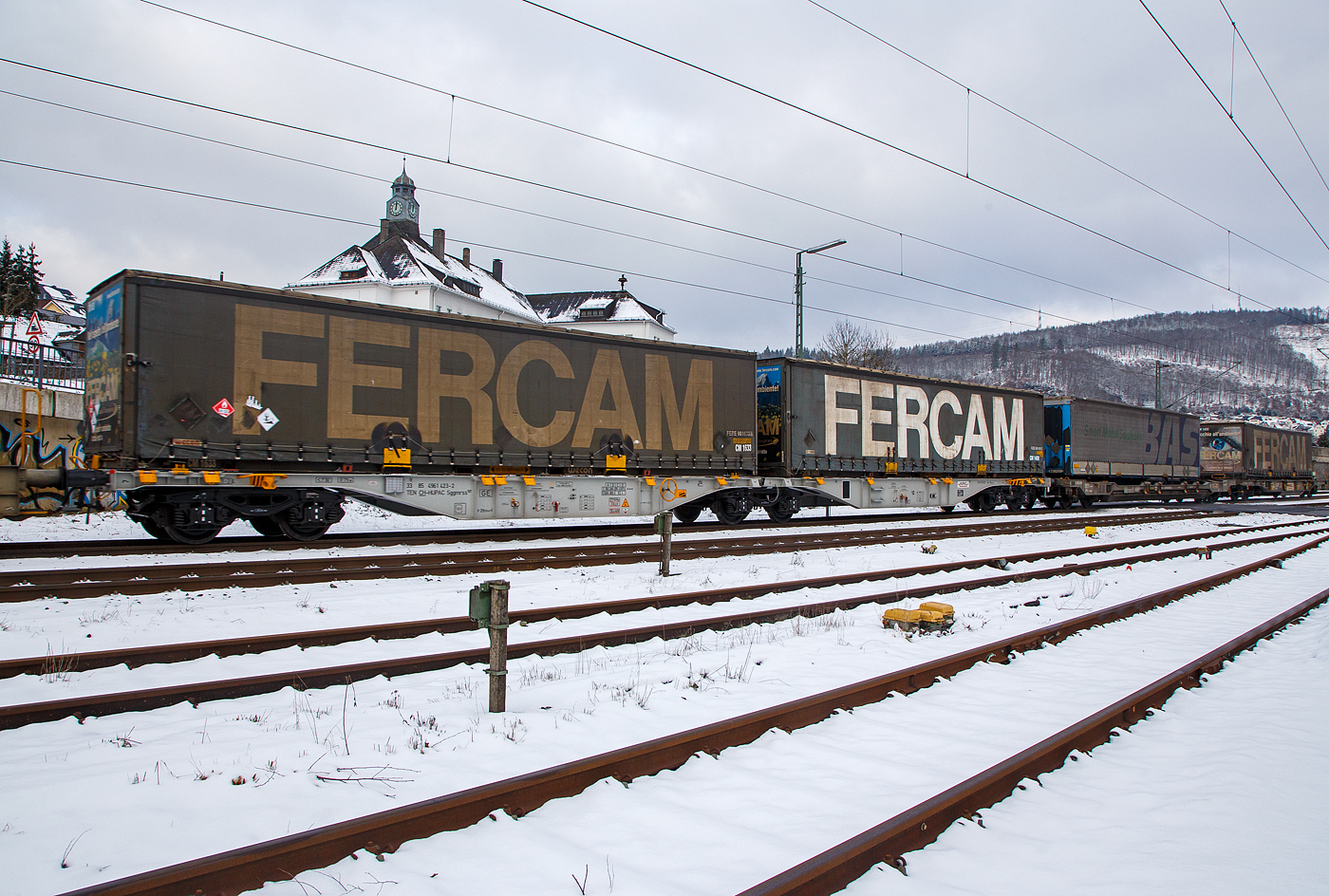Sechsachsige Drehgestell-Gelenk-Containertragwagen-Einheit 33 85 4961 423-2 CH-HUPAC, der Gattung Sggmrss 90', der HUPAC Intermodal SA, im Zugverband am 21.01.2023 bei der Zugdurchfahrt in Niederschelden (Sieg), hier beladen mit zwei Sattelauflieger-Wechselbrücken.

TECHNISCHE DATEN:
Spurweite: 1.435 mm
Anzahl der Achsen: 6 in drei Drehgestellen
Länge über Puffer: 29.590 mm
Drehzapfenabstand: 2 x 12.025 mm
Achsabstand im Drehgestell: 1.800mm
Laufraddurchmesser: 920 mm (neu)
Ladelänge : 2 x 13 820mm  (90 ft)
Höhe der Ladeebene über SOK: 1.155 mm
Höchstgeschwindigkeit: 100 km/h Lastgrenze S / 120 km/h bei Lastgrenze SS und leer)
Max. Zuladung bei Lastgrenze S: 107,5 t (ab Streckenklasse D)
Max. Zuladung bei Lastgrenze SS: 92,5 t (ab Streckenklasse C)
Eigengewicht: 27.500 kg
Kleinster bef. Gleisbogenradius: R 75 m
Intern. Verwendungsfähigkeit: TEN-GE

Gattungs-Kennbuchstaben bedeuten:
S -   Drehgestell-Flachwagen in Sonderbauart
gg -  für den Transport von Containern mit einer Gesamtladelänge über 60 Fuß eingerichtet
m - mit sechs o. mehr Radsätzen Ladelänge 18 m bis unter 22 m
r - Gelenkwagen
ss -  Höchstgeschwindigkeit 120 km/h (beladen)